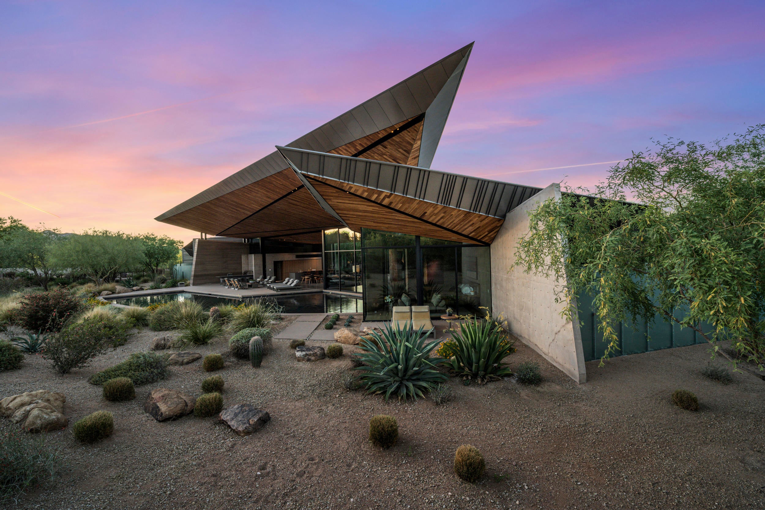 From what began as an appeal and vision to create the most alluring home in Arizona's highly sought-after Paradise Valley, Dancing Light came into being, a triumph in contemporary residential architecture that truly reflects the spirit of its natural surroundings. A sprawling 2.8 acres contains two stunning residences, with the main house and guest house consisting of 3 bedrooms and 3 ½ baths, and 1 bedroom and 1 bath, respectively. Prepare for moments of awe in this Kendle Design, Architect/Desert Star Construction/David Michael Miller, Interiors-designed 6,198 square-foot masterpiece replete with artfully functional details that extends naturally to the outdoors. Camelback Mountain is silently poised nearby, as if offering its blessing to a desert compound made up of the area's natural substances and the highest quality building materials. Enter through doors of frosted glass and be at once greeted by a sophisticated ambiance -  a desert courtyard surrounded by a comfortable, open living environment with views of the outdoors from almost any vantage point. Floor-to-ceiling sliding glass walls open up the great room into the exterior patio, eventually interrupted by soft wood panels and grey adobe-textured walls that frame the living spaces such as the ultra-modern kitchen, dining area, and wide hallways. Light streams in from well-placed windows, either at the floor, near the ceiling, or as accent walls, creating various nuanced shades in the spaces decorated by muted greys and light browns, with the occasional pops of color. The strategic placement of the pool affords cool breezes to the inside, and the roof appears as if it's rising up to meet the mountains. State-of-the-art features like Gaggenau appliances, Vola kitchen and bath fixtures, and custom woodwork fill the rooms, adding to the home's understated modern elegance. Powered by Savant technology, the entire estate can easily be controlled on-site or from a distance, whether it's maintaining the Gbtwo-meticulously designed landscape or engaging the home's security and energy systems. A stunning portrayal of domestic art, it is no wonder that the compound has caught the attention and acclaim of experts in architecture and design worldwide, being showcased in over 100 online design websites, mentioned in industry magazines and published books, and winning multiple home-building and design awards. With equally stunning views of the landscape, this home plus guest house is the perfect setting in entertainment or retreat for the most discerning of tastes.