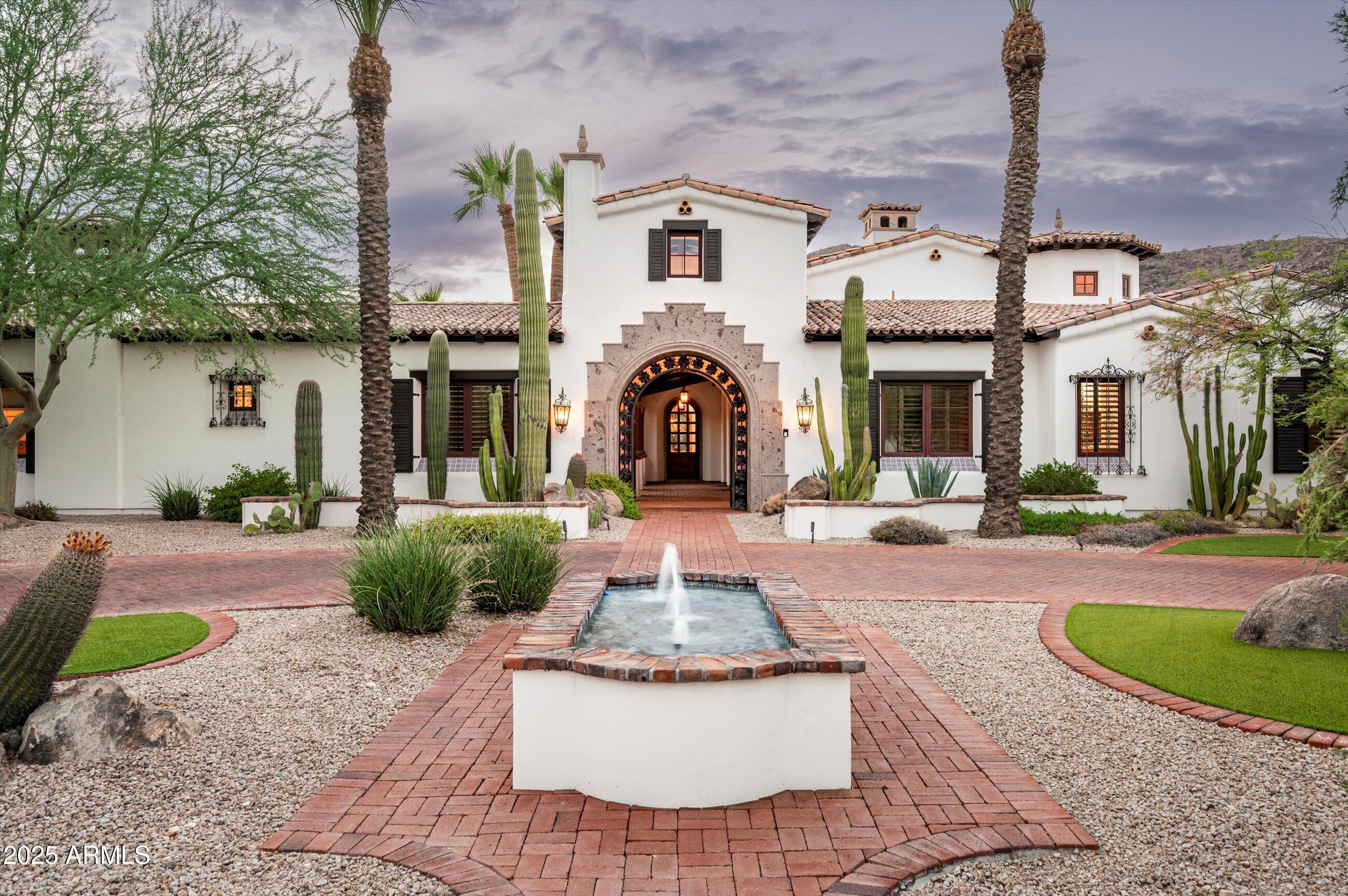 Framed by the dramatic silhouettes of Mummy and Camelback Mountain, this Paradise Valley estate blends artisan craftsmanship with a seamless indoor-outdoor lifestyle. Built by La Casona in 2013 on just over an acre, the home is introduced by a gated courtyard leading you to light-filled living spaces. A formal dining room with hand-painted dome, an elegant living room with barrel ceiling, and a media room with seating- create inviting places to gather. The kitchen pairs dual islands in butcher block and Carrera marble with a walk-in pantry and separate butler's pantry for effortless entertaining. In the great room, a stone fireplace and exposed beams open to the central courtyard. The primary suite offers its own fireplace, dual baths, and two walk-in closets, with three... additional en-suite bedrooms and guest casita add to the versatility.   A 4-car garage and room for a sport court complete this exceptional property.  Lush resort style living is complete with heated pool and spa accented by a cascading-water feature -perfect for year round relaxation and entertaining.  Expansive covered patios, native landscaping, complete with outdoor kitchen and seating areas with picturesque Camelback views. This is truly a one-of-a-kind estate where every detail reflects sophisticated craftsmanship.