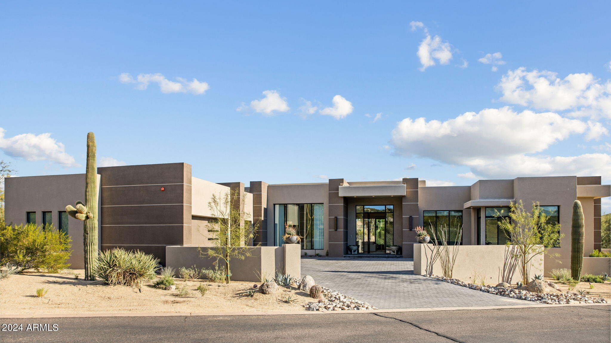 This dramatic desert modern home completed in November of 2023, nestled just within the Desert Mountain community's guard-gated entrance. Crafted with a seamless fusion of indoor and outdoor spaces, its design boasts multiple sliding glass doors, inviting the surrounding environment to become an integral part of daily life and entertaining. Collaborating with Jamie Rose Interiors, they have furnished the residence with an aura of sophistication and refinement, evident in its high-quality finishes and elegant touches throughout. This home is being sold fully furnished. The open floor plan encompasses expansive living areas, with a Chef's kitchen serving as the heart of the home. Equipped with top-of-the-line Wolf/Subzero appliances, including an icemaker and built-in Meile coffeemaker, it caters to culinary enthusiasts. Moreover, several beverage refrigerators strategically placed throughout the home ensure refreshments are always at hand. For wine connoisseurs, a custom wine cellar, along with additional storage in the pantry with its own dedicated cooling system, provides ample space for their collections.
The integration of a Crestron home automation system enhances the home's functionality, offering effortless control over audio, TV's, security, pool/spa, and surveillance cameras. Notable upgrades include automated window treatments in the Primary Suite, tinted windows for protection against sun damage, bar backlighting, and the installation of solar panels for sustainable energy.
Accommodating guests is effortless with three generously sized guest suites, including a separate casita with its own living space, ensuring both privacy and comfort. Outdoor living spaces beckon with a sparkling pool and spa, complemented by a full outdoor kitchen boasting a refrigerator, sink, and Wolf BBQ. Surrounded by inviting seating areas, they provide an idyllic setting for relaxation and appreciation of the breathtaking desert scenery.
For panoramic vistas, a roof-top view deck offers unparalleled views of the 17th hole of the Renegade golf course, captivating desert sunsets, and majestic mountain vistas, completing the epitome of desert luxury living.
