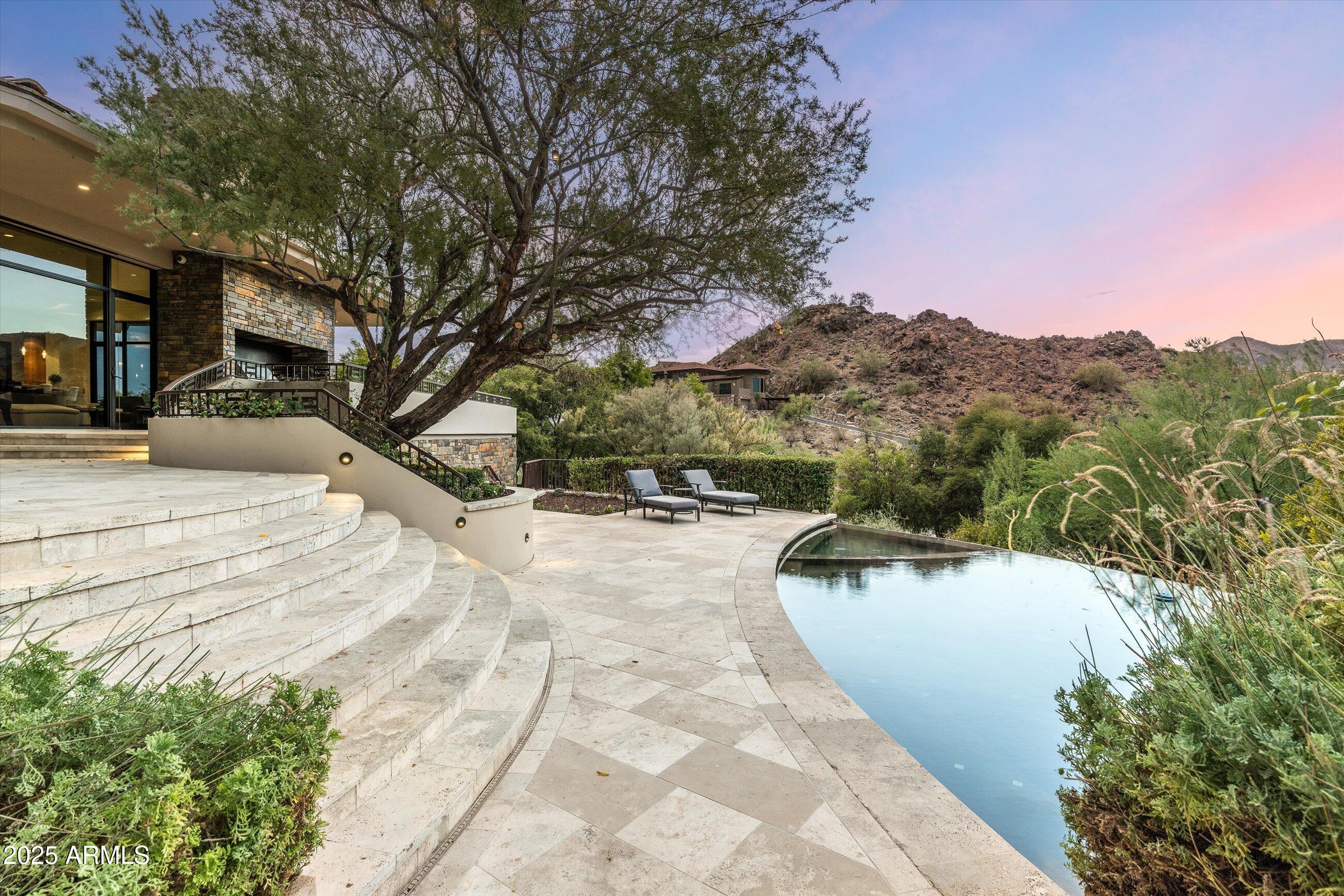 At the summit of Paradise Valley living, Altura rises above the ordinary. This architectural estate spans two residences offering a spacious main house and a fully-appointed guest house - complete with separate address. Perched on a hillside, it is positioned on a premium lot with panoramic mountain views, lush desert landscaping, and striking privacy. Grand interior volumes are balanced with warm materials: natural stone, wood-paneled walls, and expansive glass showcasing wraparound views. The main living room opens seamlessly to a sweeping travertine terrace with an infinity-edge pool below. Inside, you'll find multiple gathering spaces including a home theater, a sleek chef's kitchen open to the great room, walk-in wine storage and your own personal aquarium. With 6 bedrooms between the main home and guest house, this estate invites effortless entertaining, multigenerational living, or simply the luxury of space. And, nearby you can enjoy golf, hiking, curated shopping, and award-winning restaurants. Altura is a true retreat - discreet, architectural, and completely in tune with its surroundings.