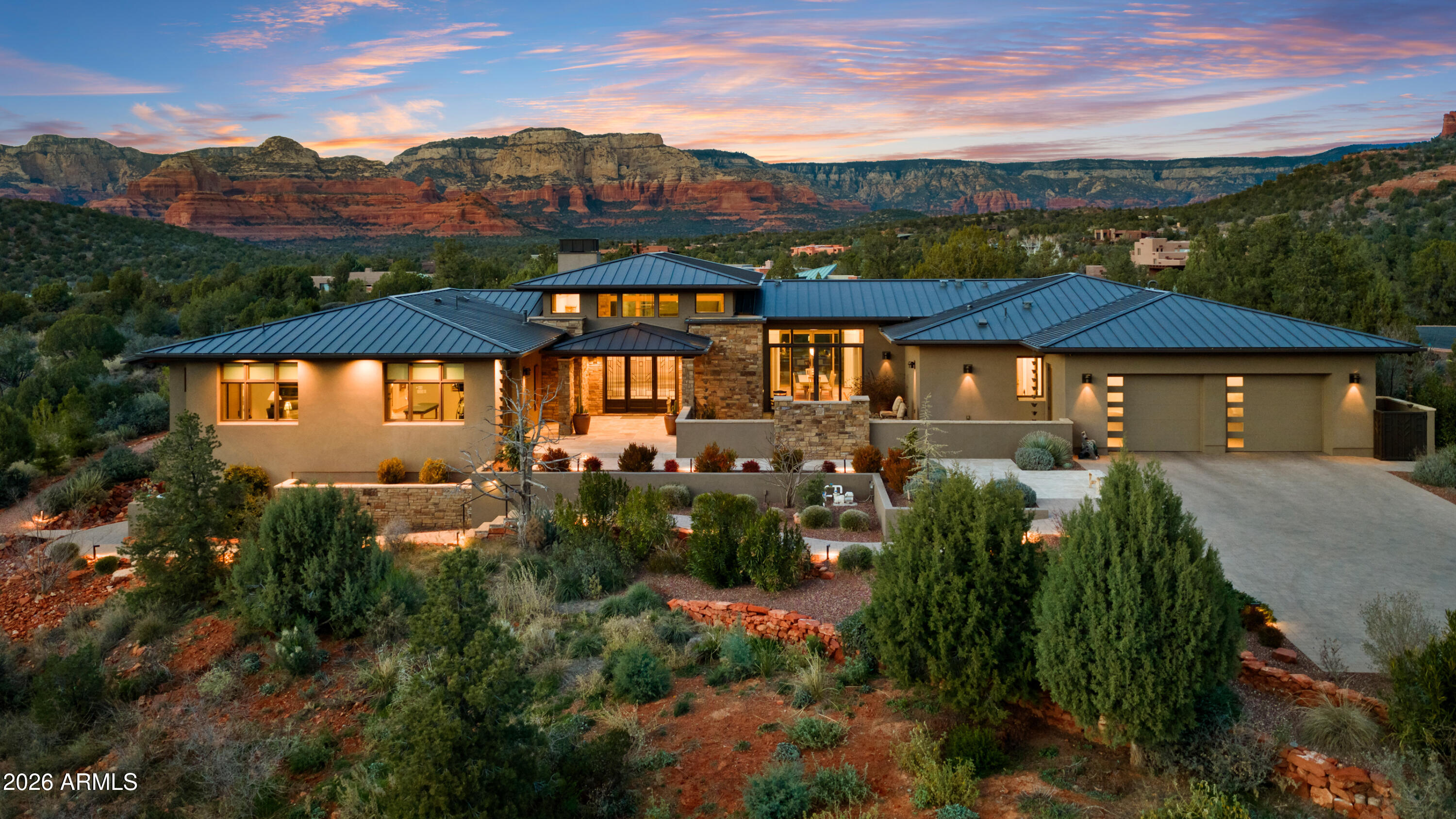 Tucked within the prestigious gated North Slopes community, this exceptional modern mission-style residence sits on more than two acres of natural forest, offering an extraordinary blend of privacy, views, and refined design. Completed in 2023, this single-level luxury home showcases thoughtful construction, high-end finishes, and extensive landscaping that together represent a tremendous investment of vision, craftsmanship, and detail.

From the moment you step through the grand entry, the home immediately reveals its sense of space and light. Expansive windows frame sweeping views while clerestory windows fill the interior with beautiful north-facing natural light. The great room welcomes you with warmth and sophistication, centered around a hand-cut cream travertine and natural stone fireplace, with large sliding glass doors that seamlessly connect indoor living with the serene front courtyard or the immaculate backyard designed for entertaining and relaxation.

The open layout flows effortlessly into the heart of the home -- a stunning kitchen featuring Taj Mahal quartz countertops and backsplash, a large island ideal for gathering, and a generous walk-in pantry. Home is also fitted with Hunter Douglas shades throughout that are all controlled via digital remote for clean and easy use. The design balances elegance and functionality, making everyday living as enjoyable as hosting guests.

The home's split floor plan creates both privacy and versatility. A dedicated office offers a quiet and inspiring environment for work, study, or creative pursuits. The primary suite feels like a private retreat of its own, with ample living space, corner windows capturing canyon views, and a spa-inspired bathroom designed for comfort and relaxation. A custom walk-in closet completes this luxurious sanctuary.

The guest wing is thoughtfully designed to provide comfort and independence for visiting family and friends. Two spacious bedrooms share a well-appointed bathroom and are complemented by a convenient coffee bar with sink and refrigerator, creating a welcoming suite that guests will truly appreciate.

Adding even more flexibility, an additional oversized bedroom is currently configured as an office or fitness space. This bright and airy room enjoys incredible views, abundant natural light, private patio access, and its own full bathroom, making it perfect for a variety of uses.

As if the main residence weren't impressive enough, the property also features a private lower-level apartment with its own entrance. Complete with a full kitchen, bathroom, and laundry, this space offers endless possibilities for extended family, guests, or a private retreat.

Outdoor living is equally remarkable. The front courtyard is beautifully finished with travertine tile and a tranquil fountain, offering views toward Jerome Mountain, while the fully enclosed backyard provides a peaceful setting surrounded by nature. Mature landscaping and careful design create outdoor spaces that feel both luxurious and serene. (Don't forget to ask for the photo album of the backyard in full bloom!)

Altogether, the home offers five potential bedrooms and four bathrooms, including the private apartment and flexible living spaces. Nearly new construction, single-level living, panoramic views, and extensive completed landscaping make this property a rare opportunity in one of Sedona's most sought-after communities.

This is more than a home--it is a thoughtfully crafted retreat where privacy, beauty, and modern luxury come together in perfect harmony.