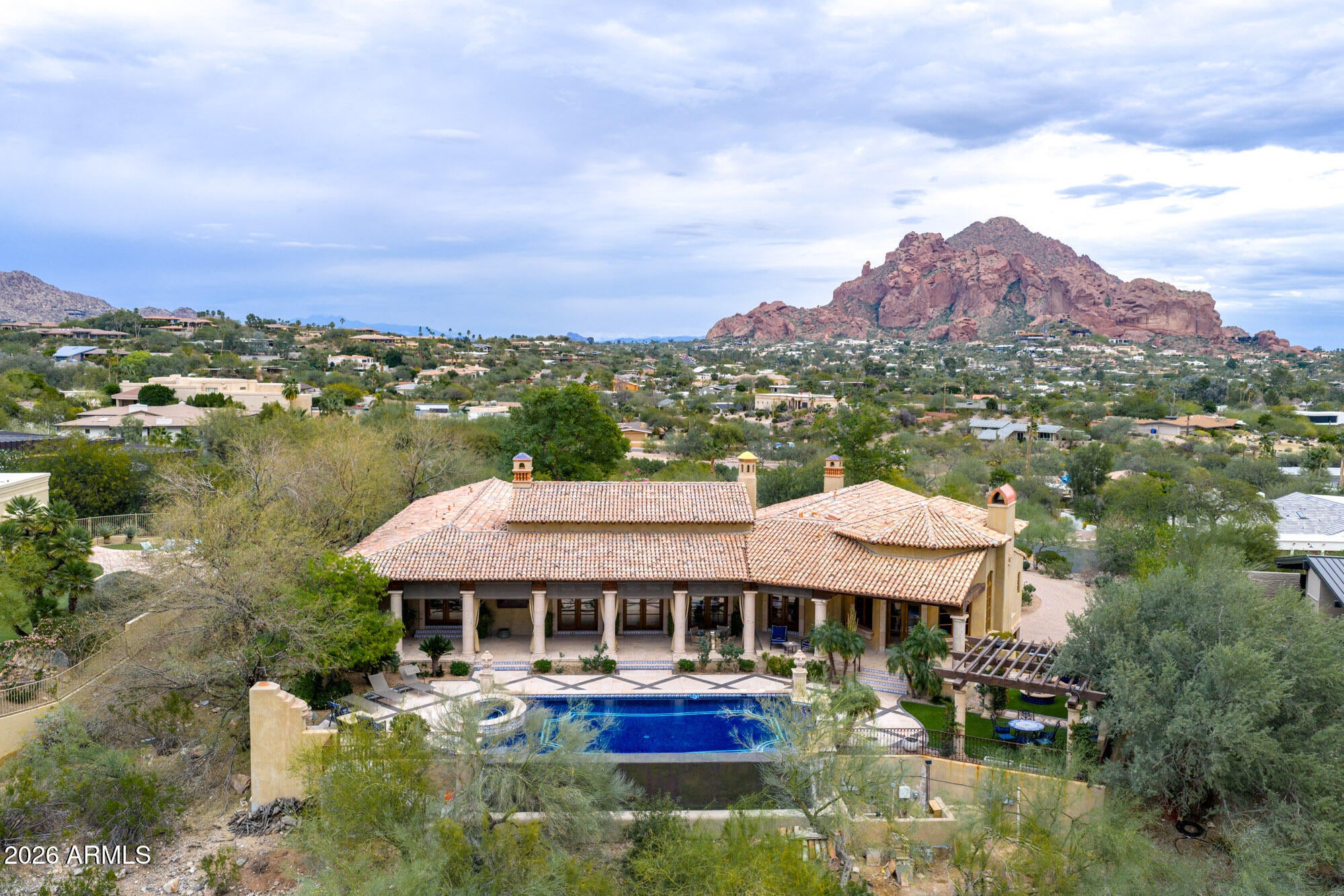 Gated Paradise Valley estate crafted by Nance Construction, offering exceptional architectural integrity, elevated finishes, and sweeping 350-degree mountain views. Privately positioned behind gates and framed by mature desert landscaping, this remarkable residence makes an immediate impression with dramatic arched entryways, soaring ceilings, exposed wood beams, paneled brick ceiling details, and hand-finished plaster walls. French doors and expansive windows flood the home with natural light, while timeless chandeliers, designer sconces, and multiple concrete gas fireplaces create warmth and sophistication throughout. The open-concept floor plan seamlessly connects the formal living room with wet bar, formal dining, and chef's kitchen—designed for effortless entertaining. The kitchen features high-end appliances, an oversized island, and its own fireplace, blending function with ambiance. Each space offers seamless indoor-outdoor living with direct backyard access and stunning mountain views. The primary suite is a serene retreat, showcasing breathtaking vistas, a private patio, fireplace, and a spa-inspired bath complete with dual vanities, a soaking tub, separate shower, enclosed water closet, and custom walk-in closet. The resort-style backyard embodies elevated Arizona living with covered patios, multiple outdoor fireplaces and fountains, and a ramada with built-in BBQ ideal for entertaining. The custom pool and spa feature ornate cement water elements and an expanded deck, all set against panoramic mountain backdrops. Additional highlights include three guest ensuite bedrooms, a nearly 1,300 sq ft finished basement with wine storage, and a three-car garage. A rare opportunity to own a timeless Paradise Valley estate where craftsmanship, privacy, and breathtaking scenery define the lifestyle.