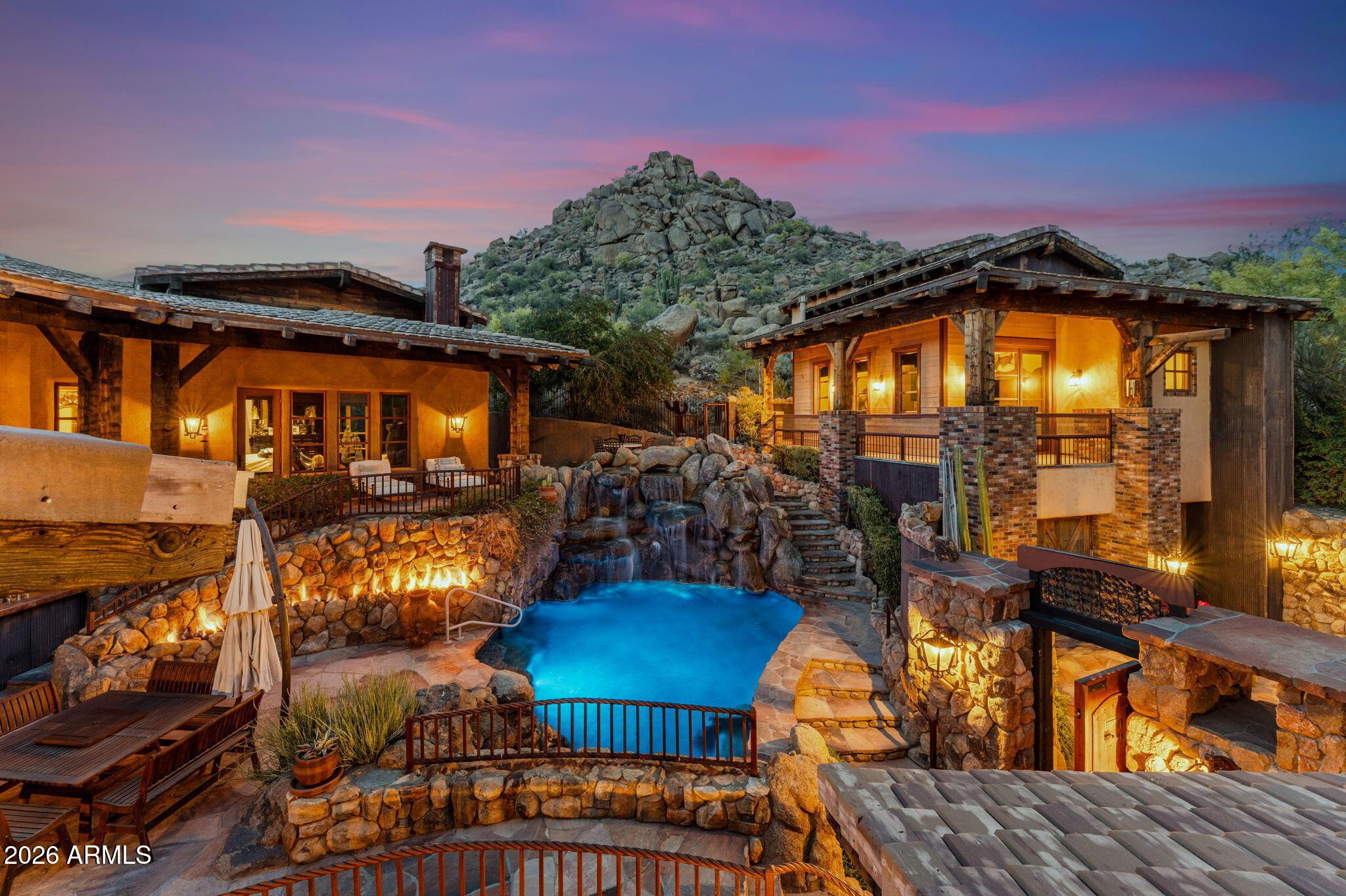 RARE ARCHITECTURE, PINNACLE PEAK VIEWS, DETACHED GUEST HOUSE, & UNMATCHED PRIVACY!

Positioned on an elevated mountainside within Estancia, this architecturally distinct residence captures unobstructed Pinnacle Peak views while delivering a level of craftsmanship that is nearly impossible to replicate.

Designed with an elegant-rustic lodge aesthetic, the home was constructed using a curated palette of imported and reclaimed materials including 150-year-old barn beams, 100-year-old pine flooring, reclaimed wood siding, rusted corrugated metal, and hand-laid stone masonry. Every element was intentionally selected to create depth, character, and a true sense of permanence. The split floor plan offers dual primary suites, an additional guest suite with private entrance, dedicated office, and an enclosed den/media room. A detached guest house provides its own living area, ensuite bedroom, and loft, positioned along a private walking path with elevated community and mountain views.

At the center of the home, a fully enclosed courtyard becomes the focal point - featuring cascading waterfalls, stacked boulders, a bridge over a pebble-lined pool and grotto, Sedona flagstone, and expansive rock fire features. The result is a controlled, immersive indoor-outdoor environment designed for both privacy and experience.

Direct access to nearby hiking trails enhances everyday livability, while recent updates including 2020 HVAC systems, newer roof, and updated appliances provide modern reliability. Four garage spaces complete the offering.

This is not a home you recreate. It's one you acquire.