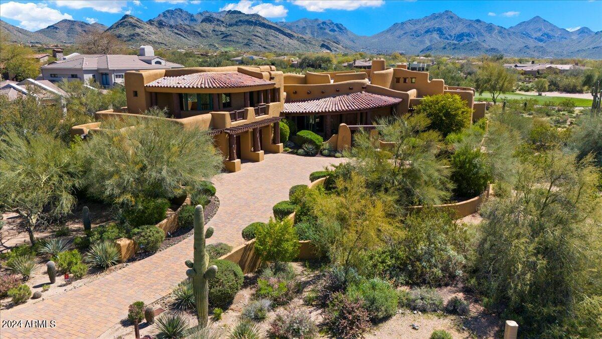 Situated on nearly an acre lot within the DC Ranch Country Club neighborhood and backing to the 6th hole, this Organic Pueblo-style custom home sits in harmony with its natural surroundings. The earth-colored palette and flowing lines of the curved parapet walls blend seamlessly with the desert landscape and backdrop of the McDowell Mountains. Warm and welcoming, the interior of the home is a treasure trove of natural materials. Hand hewn vigas, natural boulders, stone, clay and wood floors, knotty alder cabinetry and doors, carved wood and copper accents all lend to the rustic sophistication of this residence while Mexican tile accents and hand painted kiva fireplaces lend to the southwest charm.  

A paver stone driveway extends past the wooden garage doors with copper inserts to the front entry courtyard where a double wooden gate welcomes visitors. Enclosed by low walls and sheltered by a clay tile roof, the courtyard offers a beautiful space to relax and enjoy its beautiful desert garden.  

A distressed alder front door opens to the circular entry foyer with a custom radius pattern tiled floor and capped by a domed ceiling inlaid with tumbled stone.

Picture windows frame the stunning "saddle" of the McDowell Mountains and draw you into the circular great room. A hand-painted Kiva fireplace nestled against a large natural boulder anchors the corner of the room.  Hickory wood floors, 24" hand-selected viga posts, and a barreled ceiling with 12" vigas that stretch like sunrays from the faux stained glass skylight are among the many thoughtfully curated details of this room. Bordered by carved columns, the built-in buffet is both a functional space and a visual delight with seeded glass and saguaro rib cabinetry inserts, a long granite countertop and a slate and mosaic tile backsplash with copper accents.

Adjacent to the great room and separated by a low wall is the kitchen, where an irregular-shaped island with a natural boulder imbedded into one corner provides a perfect spot for prepping meals. Granite counters, a gas cooktop with a slate tile backsplash, a walk in pantry with a custom arched door, double wall ovens and a warming drawer ensure that the chef is well equipped. The Subzero fridge has custom decorative panels that provide a playful pop of color. The kitchen is open to both the nook, a relaxing space to gather for an informal meal, and the hearth room, a cozy sitting area with a kiva fireplace with hand-painted detailing.

Off of the great room, a curved gallery hallway leads to the primary retreat with hickory wood flooring and an adobe fireplace flanked on either side by irregular shaped niches, carved wood bookshelves and media area. Enjoy the mountain views through the large windows that fill the room with natural light, or step outside to the private covered patio framed by heavy wood vigas. The ensuite bathroom offers a travertine snail shower, claw foot tub, granite slab vanities, and a walk-in closet.

Two additional ensuite bedrooms are available on the main floor as well as an office that overlooks the front courtyard and contains a built-in credenza and bookcase, a custom built-in workspace, and reclaimed oak floors.  

This home is full of pleasant surprises, and as you continue down the hallway from the office, there is a beautiful wide staircase to be discovered - a work of art in itself with colorful Mexican tile risers, wide hickory steps and a hand-hewn railing.  Halfway up the stairs is a wide landing, adorned with a viga and latilla ceiling, that overlooks the kitchen, nook and hearth room. The staircase leads to two upstairs guest bedrooms with walk in closets and a jack and jill bath. Clay tile and maple wood floors infuse the upper level with warmth. In addition, a large balcony is accessible from the second level hallway, with captivating views that overlook the city to the south, west and north to Pinnacle Peak.

At the rear of the home and extending off the main living areas, a deep covered patio offers an abundance of space for dining and lounging.  A cozy outdoor sitting area with a kiva fireplace and outdoor TV is the perfect place to relax and retreat at the end of the day.  

The backyard is the perfect setting for enjoying the outdoor Arizona lifestyle. A water feature - a 25 ft stream of natural boulders - flows into the giant 900 sf saltwater pool with 2 race lanes. A spacious ramada provides the perfect sheltered area for the outdoor kitchen, complete with a built in barbeque, sink, fridge and stainless steel cabinetry for grilling supplies and dining accessories. Gather around the large firepit with bench seating on winter evenings, or unwind in the heated raised spa that spills into the pool. A generous grassy play area of low maintenance artificial turf, and a pool bath with a walk-in shower, hand-painted ceramic sink and coordinating glazed Mexican tile ensure that no detail has been overlooked in this outdoor paradise.  

Tucked away, but certainly not to be missed, a winding saltillo and Mexican tile staircase leads to a rooftop deck with both covered and uncovered patio areas and stunning 180 degree views overlooking the golf course and McDowell Mountains to the east, and the city to the south and west. This balcony has an additional outdoor kitchen, adobe fireplace and ample space to entertain guests while watching the glow on the mountains at sunset and twinkling city lights at night.

With its prime location within the DC Ranch neighborhood, this classic residence offers a lifestyle of upscale amenities and convenience. The community offers 33 miles of manicured paths and trails, 47 community pocket parks, 2 community centers, and is located adjacent to the McDowell Sonoran Preserve and just 5 minutes north of the 101 Freeway in North Scottsdale. The property is also conveniently located within walking distance of Market Street's retail shops and restaurants. Membership to the Country Club at DC Ranch is available by separate application, approval, and membership fee.