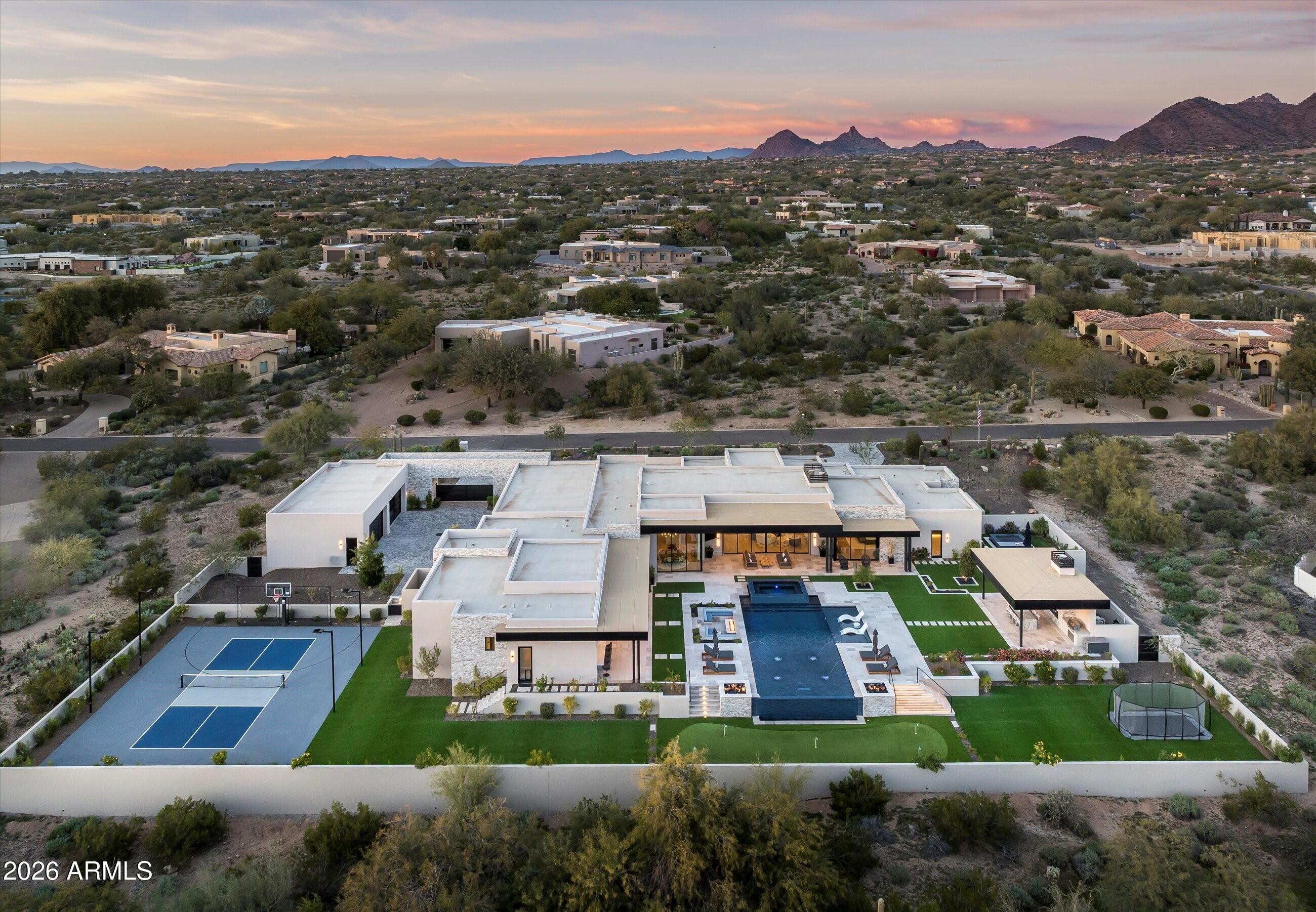 An estate defined by intention, scale, and warmth. Arrival is nothing short of dramatic. A circular driveway guides you either to the private 8-car auto court or toward the main entrance, where floating steps glide over water, leading to twin fountains, centered between them, a striking floating fire feature sets an unforgettable tone before you even step inside.
The entry is marked by a double-height pivot door of frosted glass, framed by matching windows. As the door opens, you are immediately feel transported into a true estate, introduced by soaring 20-foot ceilings and a perfectly aligned sightline straight through to the backyard, revealed through a full wall of pocketing glass doors.
The great room is nothing short of grand, designed to be experienced from every angle. A dramatic tray ceiling is crowned by an elegant statement light fixture, while a floor-to-ceiling stone fireplace with decorative built-ins with backlighting anchors the space. The wall of glass dissolves completely into the wall, allowing the indoors to flow seamlessly outdoors and filling the room with natural light.
Transitioning toward the kitchen, a fully equipped wet bar connects the spaces effortlessly, featuring an ice maker, beverage refrigerator, and custom cabinetry that blends perfectly with the kitchen, this space is ideal for both everyday living and entertaining at scale.
The open kitchen itself is warm, luxurious, and meticulously designed. Dual islands are topped with a waterfall marble that continues seamlessly upward as a full-height backsplash, its veining both dramatic and bewitching. Above, the light fixtures hover, casting a soft glow that enhances the richness of the two-toned cabinetry. The space is fully appointed with double Wolf ranges, a custom vent hood covered in marble, a built-in espresso machine, and an extra-wide, panel-faced refrigerator, all integrated effortlessly.
Tucked discreetly (invisible by design) is the butler's pantry and back kitchen. Fully outfitted with an additional Wolf range, vent hood, refrigerator, sink, and dishwasher, this space is as beautiful as it is functional. Rich, warm-toned cabinetry, abundant storage, and carefully selected hardware elevate it beyond utility into a true design moment. From here, a pocket door leads into the formal dining room, continuing the home's refined elegance. The space is anchored by a temperature-controlled, full-height glass wine wall, both a functional feature and a stunning visual statement.
Just off the kitchen, the breakfast nook offers an inviting place to gather, centered beneath a striking statement light fixture. Two walls of pocketing glass doors frame the space, opening directly to the backyard and allowing natural light to pour in throughout the day. From here, a thoughtfully designed hallway leads you toward the home's entertainment wing. Gallery-style art lighting and bespoke sconces line the corridor, setting the tone as you approach the theater room. Double sliding barn doors serve as both a functional feature and a bold design moment, opening into a space designed for both comfort and connection. The theater is equipped with full surround sound and opens once again to the backyard through a wall of pocketing glass doors. There is a show-stopping wet back with back-lit shelves that enhances the experience, featuring a sink, ice maker, and beverage refrigerator. The fully pocketing pass-through window connects the bar directly to the outdoor living area and pool area, effortlessly transforming it into an indoor-outdoor serving space. A nearby bathroom with exterior access adds both convenience and flexibility for guests enjoying the outdoor amenities.
This wing of the home also includes a well-appointed laundry room and three additional ensuite bedrooms, each offering a private bathroom and walk-in closet. One of these rooms has been thoughtfully transformed into a dedicated fitness studio, complete with padded flooring, a mirrored wall, and a ballet barre.
Opposite the theater, a private attached casita offers exceptional versatility. Ideal as a guest retreat or multi-generational living space, it features a full bathroom with dual vanities, a well-appointed kitchenette with a beverage refrigerator, sink, storage, and direct access to the front patio, where a firepit creates a welcoming outdoor extension of the suite.
The east wing introduces a warm and stylish powder room, thoughtfully designed with character and unexpected detail. 
The primary suite is a retreat that is both expansive and indulgent. The bedroom itself is generously scaled and anchored by a dramatic floor-to-ceiling marble gas fireplace, creating an atmosphere that feels refined and inviting. A beautifully appointed private wet bar adds another layer of luxury, featuring a sink, beverage refrigerator, and built-in espresso machine, perfect for mornings or quiet evenings in. The suite continues to impress with the exceptional walk-in closet, which is sure to impress in both size and design, complete with a custom storage island, and so much tailored cabinetry, and the added convenience of an in-suite washer and dryer.
The ensuite bath is designed as a spa experience. Separate vanities provide individual space, while a private water closet enhances comfort. The expansive steam shower with full-height glass front is outfitted with a rain shower head, dual wall-mounted shower heads, dual handheld wands, and wall-to-wall integrated stone bench that offers both function and a seamless, intentional design. Across from the shower, a freestanding soaking tub invites relaxation, while a full Red Light & Infrared sauna brings a true wellness element into the suite. Outdoor access further elevates the experience. One exit leads directly to the backyard and pool, while a second opens to a fully private courtyard featuring a jacuzzi spa and serene mountain views, creating a secluded retreat that feels worlds away.
Stepping outside, the experience continues with the same sense of calm intention that defines the home. The backyard is thoughtfully composed to feel both expansive and serene, with each element placed to enhance the overall flow rather than compete for attention. Covered patio spaces provide inviting areas for outdoor dining and relaxed seating, creating a natural extension of the interior living spaces. A dedicated gazebo serves as a true outdoor gathering point, featuring a built-in barbecue and smoker, centered by a fireplace that anchors the space. Integrated retractable roll-down shades allow the area to transition effortlessly from day to evening.
The pool is designed as a visual and experiential centerpiece. An infinity-edge spa leads down to the pool, while a Baja shelf offers a place to lounge to the opposite side, a sunken seating area with a fire pit creates a quiet place to gather. As the pool extends outward, its infinity edge is framed by symmetrical fire features, producing a cascading effect that unfolds to the, a five-hole putting green that is subtly integrated into the landscape, blending recreation into the natural setting. To one side, an in-ground trampoline, to the other an open green space, provide room to play or unwind, leading naturally to the sports court. Designed for versatility, the sport court accommodates both full-size basketball and pickleball, completing the outdoor experience with balance and flow.
Beyond the sport court, the property loops seamlessly back toward the front auto court through a gated entry that fully pockets into the wall, disappearing entirely from view, a detail that speaks to the home's thoughtful engineering as much as its design. Here, two climate-controlled four-car garages face one another, offering accommodation for up to eight vehicles. One garage has been designed with the flexibility to convert into a detached casita. The second is outfitted with expansive walk-in storage and an integrated tool wall. Within one of these spaces, an immersive IMAX simulator adds another layer of experience. Far beyond traditional golf simulation, it supports a range of interactive sports, shooting, and many more activities, powered by advanced multi-camera detection technology for an incredibly dynamic experience.
The estate is fully integrated with a Control4 smart home system, providing seamless control of lighting, climate, audio, and automated in-wall shades throughout the residence. A built-in speaker system extends across the home and into the outdoor living spaces, including the covered patios and gazebo, ensuring a consistent experience indoors and out.
All of this is set within Pima Estates, one of the area's most coveted enclaves, known for its privacy, space, and timeless appeal. It's a setting that perfectly complements a home designed with intention, serenity, and lasting presence.