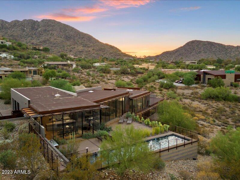 Designed by award-winning FAIA architect Eddie Jones of Jones Studio and fabricated by premier builder The Construction Zone, the artful fusion of modern materials, integrated into the pristine Sonoran desert is an inspired vision brought to life. Unwind with expanded mountain views and city lights to rejuvenate your soul every day throughout the years!  The unmistakable inspiration of Frank Lloyd Wright and the Modernism of Jones Studio are perfectly expressed in this fine residence positioned hillside above Tatum Blvd.  Facing sweeping vistas on the eastern horizon, floor to ceiling glass captures superlative views of the McDowell Mountains!  The many details of the home are reminiscent of the fit and finish of a luxury yacht and yearn to be experienced for full appreciation. Surrounded by views, the home is set on 1.76 acres for privacy and has been substantially upgraded since 2019.  Superbly crafted with a unique blend of masonry, steel, wood and glass: the quality of the build is evident throughout.  Your epicurean kitchen is equipped with a full array of the finest Miele appliances and caters to the foodie and connoisseur alike.  Top-of-the-line major systems of the home include: recently upgraded and customizable Crestron security system for complete convenience, automated window shades, variable-speed HVAC, highly upgraded EV charging over-sized 3 car air-conditioned garage, recently installed premium whole house water system, recirculating tank-less gas fired water heaters, added floor level heated vents in primary bath, lighted vanity mirrors, organizational electric plug drawers, luxurious towel warmer, elegant control systems, built in shower trays for flow and continuity.  LED lighting through-out, pre-wired for sound, recent new pool system equipment installed, conversation area warming fire and so much more. 
 
A list of designer furniture will be sold with the home.

The primary bedroom has been transformed with deluxe closet cabinetry, dressers, side tables, designer pulls and low-profile ambience lighting and a customized complete king bed system beyond compare.  Luxury extras you expect in a fine property have also been added to the primary bath. There is a music/reading room also on the main floor.  

Completely redesigned, the laundry/pantry area is now an upscale, highly-functional favorite workspace. 

The lower level has 3 en-suite bedrooms with beautiful views, a fitness/yoga room and a media lounge space with patio access.  The largest en-suite bedroom also has a separate patio entrance and could be a second primary.

Panoramic mountain vistas with hanging clouds, picturesque skies and the most gorgeous sunrises, this is truly an inspirational property to be experienced.
