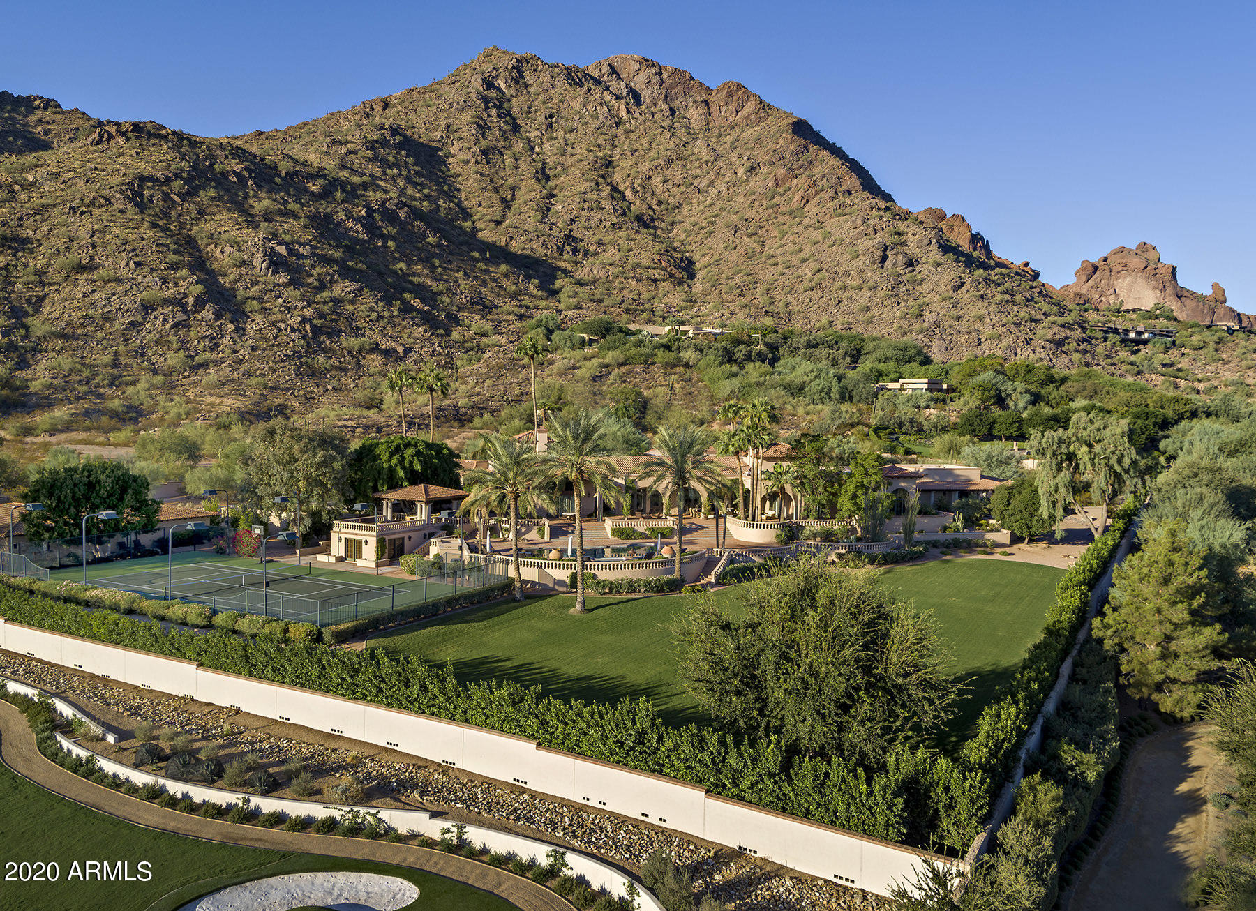 This idyllic Spanish Colonial Revival Estate sits on one of the best view lots in Cameldale. From northern mountain ranges to Four Peaks and beyond, an evening on the patio will take your breath away! Casually elegant and fastidiously maintained, this easy and generous floor plan offers a grand entry into an attractive living room with striking 16' ceiling detailed with rich beams and flowing into one of the most charming dining rooms ever to entertain your guests. All of the high 14-16' ceilings throughout reveal eye-catching designs, each different and impressive. A wood paneled library sits just off the foyer enriched with beautifully crafted millwork and high arching windows to take in the view of Camelback Mountain. The inviting family room is warmed with fireplace and bar service... from an antique bar created in France. The kitchen is open to a cozy smaller family room and casual dining area with fireplace. Fabulous patios and a large open terrace create the best outdoor experience with seating around the firepit and overlooking pool and spa as you gaze at the brilliant views. The Master retreat has an intimate seating area and high ceilings, spacious Master bathroom and large walk-in closet. Additional bedrooms are very roomy and classically appointed with their own TV/family room and patios. The Guest House is complete with 2 bedrooms, living room, kitchen, laundry room and garage, and there is a sport/gym house at the tennis court level. Gated with circular entry driveway, you will know you have arrived at this resplendent Estate.