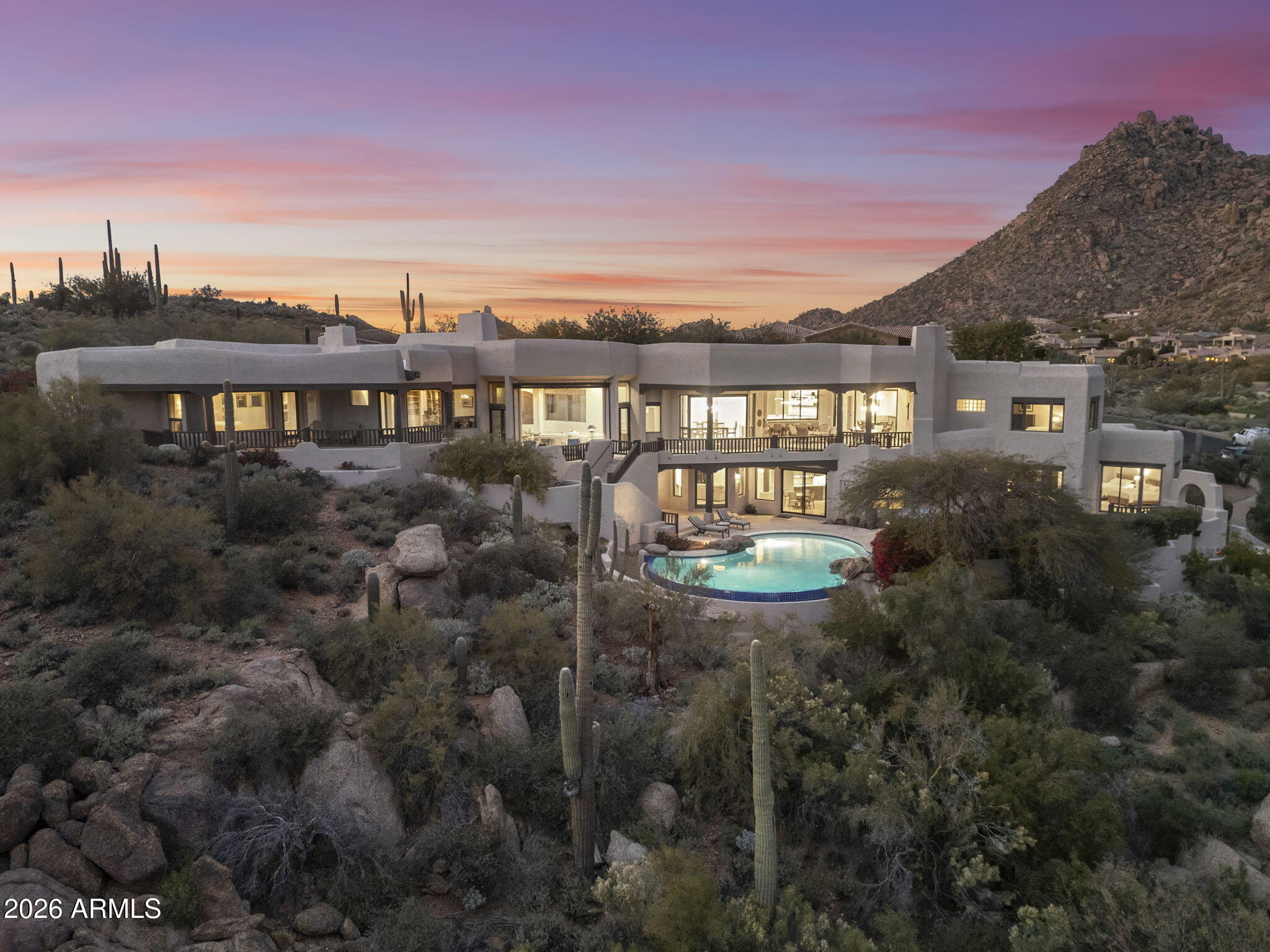 Commanding an extraordinary setting in the guard gated community of Glenn Moor in Troon Village, this estate is a rare convergence of architectural artistry, panoramic desert beauty, and refined luxury living. Perfectly positioned against the McDowell Mountain preserve and overlooking the Par 3 signature hole of Troon Country Club, the residence captures sweeping mountain silhouettes and golf course vistas that unfold from sunrise to sunset, creating a truly elevated living experience. Thoughtfully enhanced with significant updates, the home honors its Southwest-territorial roots while introducing a modern, sophisticated aesthetic. Recent improvements include a beautifully updated kitchen, a reimagined great room designed for grand yet comfortable entertaining, refreshed flooring throughout, exterior paint and wood sealing, and a fully remodeled lower-level with 2 bedrooms, a kitchenette and secondary family room for guests or multi-generational living. Architectural details define the home's character. Exposed wood beams, custom stone and plaster fireplaces, expansive walls of glass, and curated finishes create a warm, elevated atmosphere that blends seamlessly with the surrounding desert landscape. Generous living and entertaining spaces flow effortlessly, complemented by a striking wine display and thoughtfully designed gathering areas that invite both intimate evenings and large-scale entertaining. Designed to celebrate Arizona's coveted indoor-outdoor lifestyle, multiple covered patios, balconies, and view decks extend the living spaces into the natural surroundings. A resort-style pool terrace is perfectly positioned to enjoy serene privacy, dramatic mountain backdrops, and unforgettable sunsets, offering an ideal setting for entertaining or quiet relaxation. Every outdoor space has been oriented to maximize views, privacy, and connection to the landscape. Set within one of North Scottsdale's most sought after luxury enclaves, the property offers a rare sense of seclusion while remaining moments from golf, world-class hiking and biking trails, upscale dining, and shopping. This location balances luxury, recreation, and tranquility in equal measure.