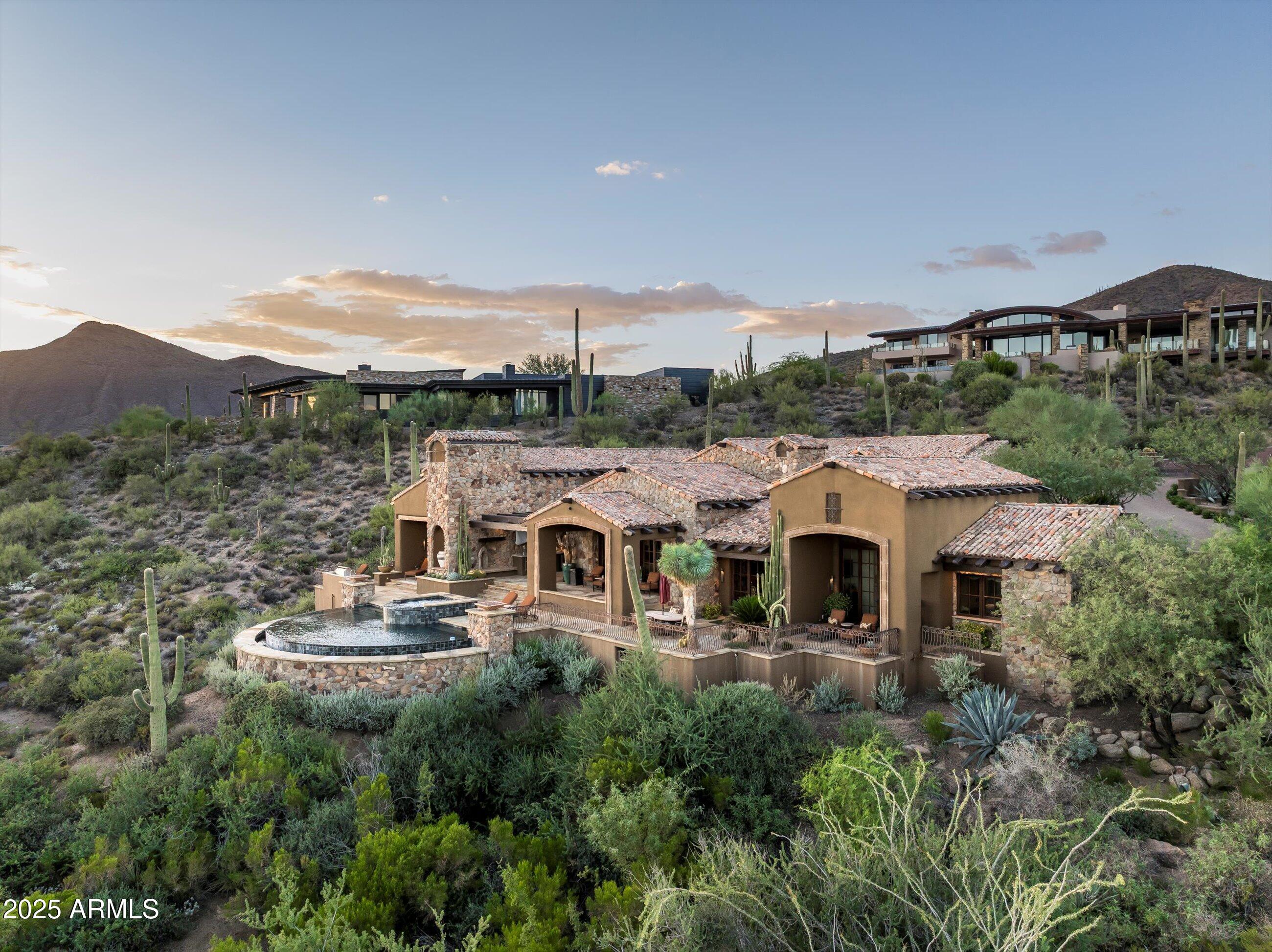Desert Mountain GOLF MEMBERSHIP available. Welcome to this Exceptional Private Desert Mountain Estate - A Masterpiece of Luxury Living Nestled in one of Desert Mountain's most coveted enclaves, this exceptional estate is a true testament to uncompromising quality, artisan craftsmanship, and refined design. Every inch of this home exudes sophistication, offering an unparalleled lifestyle. As you enter the gated entry, you're greeted by lush desert landscaping, mature trees, and indigenous plants that provide both beauty and privacy. This home commands attention without shouting—offering an oasis that is both serene and awe-inspiring. Step through the grand entryway into a world of elegance. The expansive open-plan living area features soaring ceilings, where light pours in through he doors perfectly framing panoramic views of the surrounding mountains and desert. The home's craftsmanship and attention to detail are immediately evident in every corner: custom beam work, soft Venetian plaster, warm hardwood floors, natural stone and brick accents all seamlessly flow throughout the space. Neutral tones create a serene atmosphere that invites both calm and sophistication, making every room feel like a sanctuary.
The dining and living area are entertainer's dream, with well appointed wet bar and the striking fireplace that serves as a focal point, creating a warm and inviting atmosphere. The wine room offers ample space for storing your finest collection.
The heart of this estate is undoubtedly the gourmet kitchen, a chef's dream featuring top-tier appliances, a generous center island, and custom cabinetry. Whether preparing a quiet dinner or hosting an elegant gathering, this kitchen is designed to rise to any occasion. The kitchen flows effortlessly into the adjacent open-plan living area, where a fireplace provides warmth on cooler evenings. Sliding doors retract to reveal the outdoor sanctuary, blending the indoors with Arizona's natural beauty.
The private library, an inviting space for both work and leisure. With custom-built bookshelves and ample natural light, this tranquil room includes dual desks and double doors to patio with expansive views.
The owner's suite is a private haven designed for relaxation and rejuvenation. Featuring large fireplace, a spa-like bathroom, walk-in closet, and thoughtful finishes, this sanctuary also boasts breathtaking views of the mountains and valley. The dual-owner's suite, complete with its own fireplace, sumptuous bath, and private patio, offers your guest the ultimate in luxury living and privacy.
Additional guest en-suite are equally spacious and well-appointed with private balconies perfect for family, guests, or for transforming into a creative space. Every inch of this estate has been designed with both comfort and style in mind, ensuring every family member and guest feels like royalty.
This homes resort-style backyard truly sets it apart, from the sparkling pool and spa to outdoor kitchen with top tier BBQ and refrigerator, fire pit patio to the cozy dining patio with smoker and
fireplace every detail has been designed to enhance your lifestyle and to create an entertainer's paradise. Surrounded by lush desert landscaping offering breathtaking views of the Sonoran Desert, golf course, mountains and valley below this space offers the perfect blend of privacy and is the perfect setting for al fresco dining, intimate gatherings, or simply unwinding in nature.
Saguaro Forest 165 was designed by Terry Kilbane, built by Madison Couturier, and is made for a life well-lived. This estate is more than just a home; it's a story...one that you'll love living every day.
For those who appreciate both functionality and luxury, the three-car garage provides ample space for your vehicles, tons of storage to meet all your needs, air station and also features an air-conditioned exercise room, perfect for a home gym, yoga studio, or personal fitness space.
Crestron system allows you to control home both while in residence or away from home.
A Golf Membership to the Desert Mountain Club is available for purchase upon approval from the Desert Mountain Club