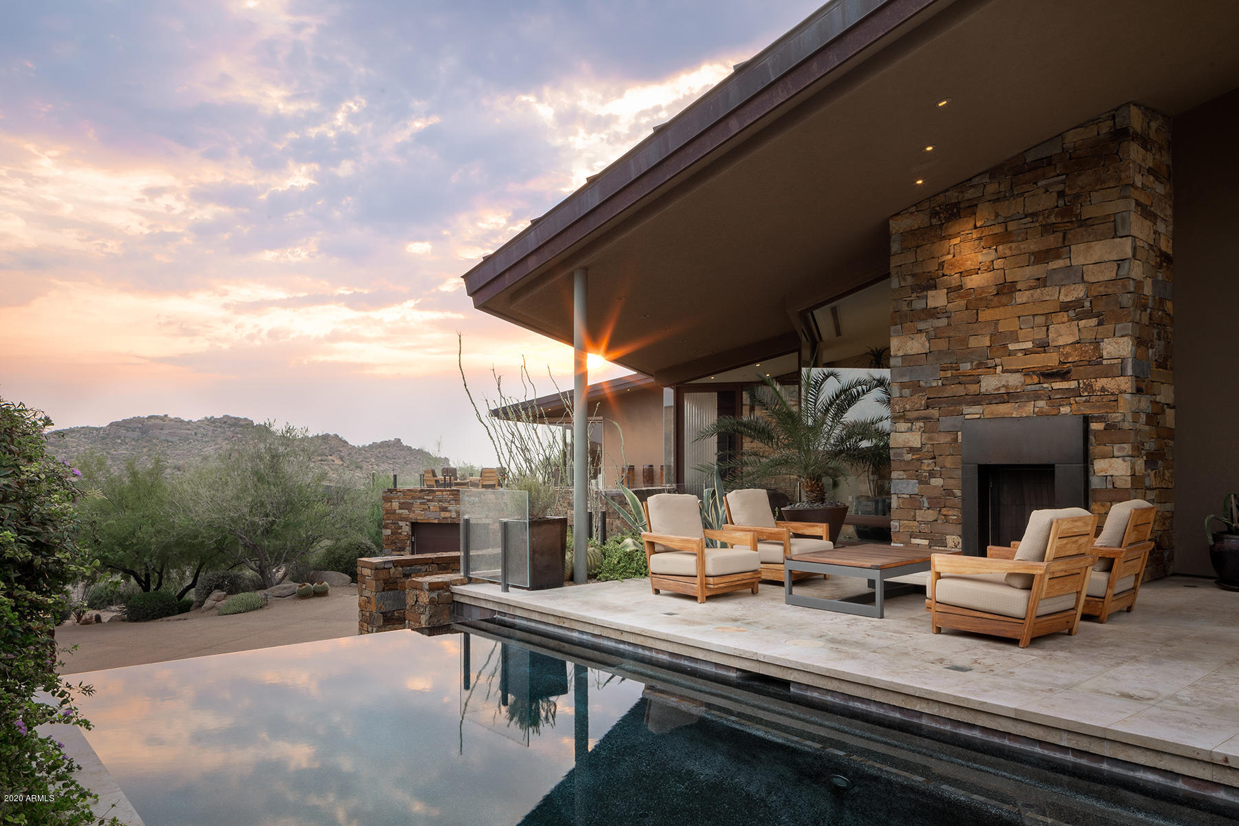 Located in renowned guard-gated Estancia, in Scottsdale, this modern desert residence illustrates the grand result when combining an exquisite view lot, a highly esteemed contractor/builder and a top-rated design team. Sited on a gentle-sloping hillside parcel, with breathtaking Pinnacle Peak and city light views, Glen Ernst/Peak Ventures has constructed a contemporary jewel box, showcasing the beauty of combining nature's elements with man's work. Renowned designer David Michael Miller has created an interior that is at once wondrously luxurious and sublime, instilling a sense of serenity. German Polished Limestone Floors, natural light wood finishes, glass walls that disappear to bring the outdoors in, solid block construction, 80 solar panels and a two-hundred-year Copper Roof are just some of the features to be found. The floor plan is open and relaxed, with a state-of-the-art kitchen that flows seamlessly to both casual and formal dining and a great room that is perfect for any entertaining. Natural daylight abounds, augmenting a light and bright home. Spacious dual home office, expansive master bedroom retreat, a peaceful and gracious library/reading
room and one of the finest media rooms ever to behold. Guests are offered one of three private suites, two are detached from the main residence. One guest house could readily convert to a home workout gym. Additional features include a temperature-controlled wine cellar and professional home elevator. Beautiful
southwest-facing private pool and spa are designed and located to be a seamless and integral part of the of this amazing residence.