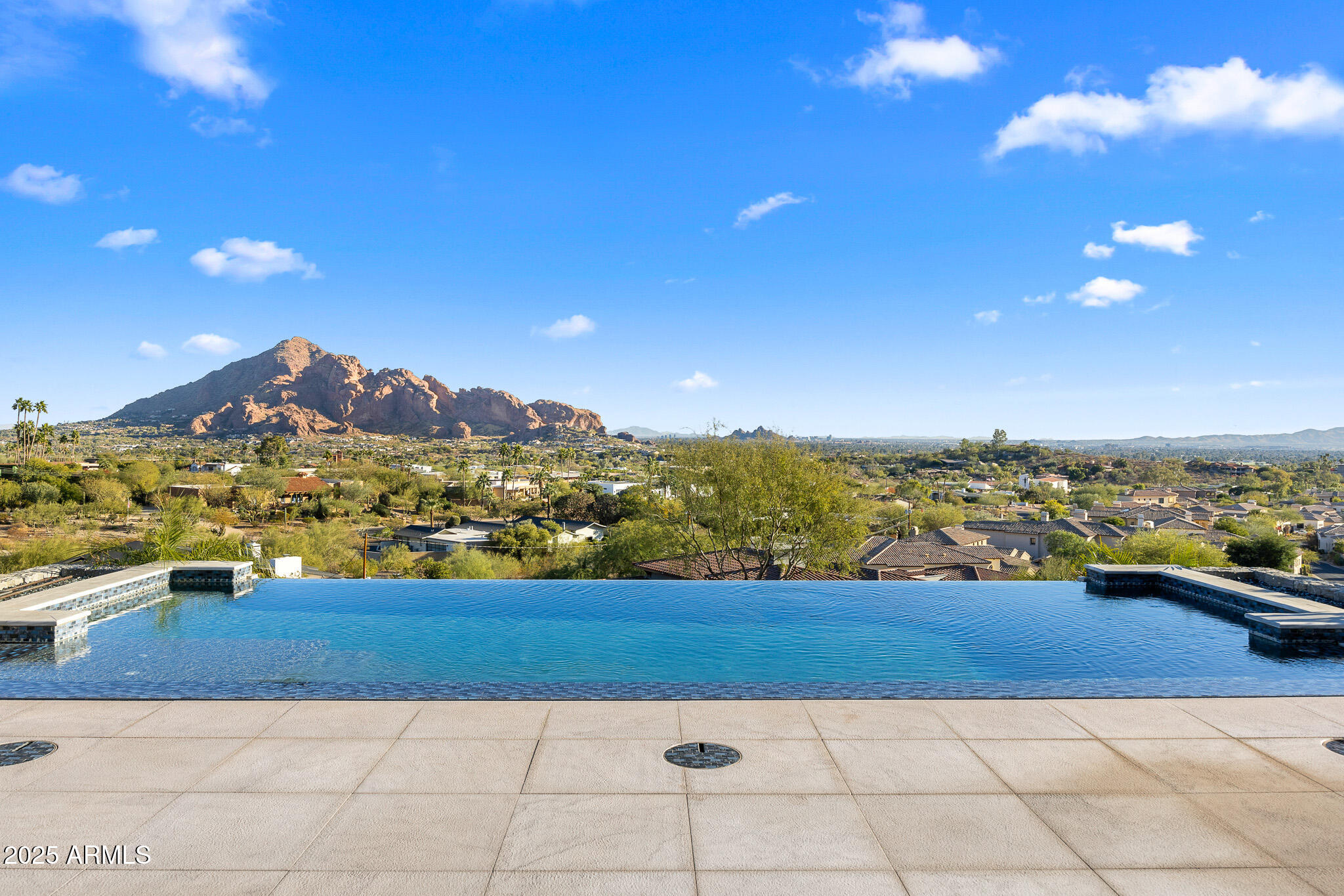 Set on 2.17 hillside acres, this extraordinary contemporary estate is perfectly designed to complement its stunning hillside location. With sweeping views of the valley, city lights, and Camelback Mountain, this home offers a rare combination of beauty and seclusion. Surrounded by native hillside and lush landscaping, the residence exudes masterful craftsmanship, from the intricate tilework to the hand-laid natural stone waterfall that cascades gracefully down the hillside. Designed for seamless indoor-outdoor living, the home maximizes its views from nearly every room. The great room, with its soaring 25-foot ceilings, is made for entertaining, featuring a striking Himalayan fossil stone fireplace and a sophisticated custom glass bar with under-lit accents.... ...The chef's kitchen is a dream, with a sprawling quartz waterfall island and top-tier appliances from Wolf, Sub-Zero, and Miele, including a 60" range with double ovens and a built-in Miele coffee/espresso machine. Expansive walls of glass doors open directly to the outdoor living areas, offering the best views of Camelback Mountain and the city. The outdoor spaces are perfect for entertaining, with shaded dining and living terraces equipped with heaters and a misting system, an infinity-edge pool, heated spa, sundeck, and a fire pit lounge.

The luxurious master suite offers a spa-inspired bath with iceberg grey marble countertops, double vanities, and a TV in the mirror. The custom-designed his-and-hers closets are truly exceptional, featuring 11 electric clothes cabinets and built-in safes for each. Her closet includes a glamorous vanity with a Kallista makeup sink, a TV in the custom-lit mirror, and surrounding display cases.

The three additional en-suite guest rooms each feature private balconies with beautiful valley views. The home also boasts a modern theater, a fully equipped gym, a putting green, a built-in BBQ, and a Celtic custom 3-floor elevator. The Crestron Automation System allows for easy control of A/V, lighting, shades, and the pool, while commercial-grade roller shutters ensure security when you're away. With two garages providing space for up to six cars, this estate is the perfect haven for both luxury living and privacy.

Located within a guard-gated community, this exceptional home is just minutes from world-class shopping, dining, golf, and cultural attractions, offering the perfect blend of elegance, modern luxury, and serene seclusion.