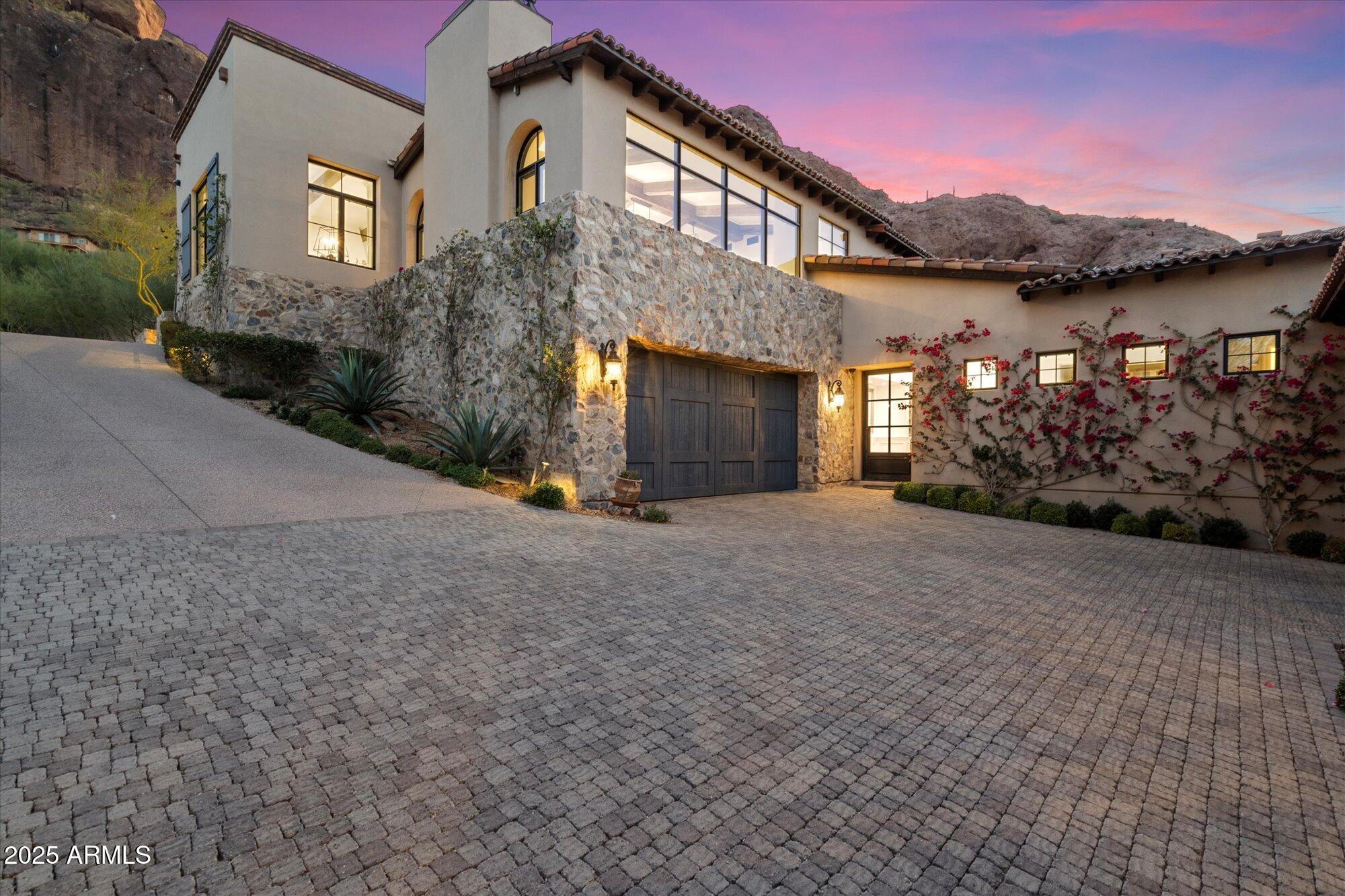 Perched at the base of Camelback Mountain, this extraordinary luxury estate offers breathtaking views and an unbeatable location. The main residence spans two levels, featuring a sophisticated living room and a gourmet kitchen designed for both functionality and style. The lower level boasts four spacious bedrooms, including a stunning primary suite, plus a private theater room for ultimate relaxation. A serene courtyard with a sparkling pool provides a picturesque retreat framed by mountain vistas. An additional building offers a refined entertaining space with a caterer's kitchen and a private guest suite. With its dramatic stone facade and exceptional design, this home is a true statement of luxury.