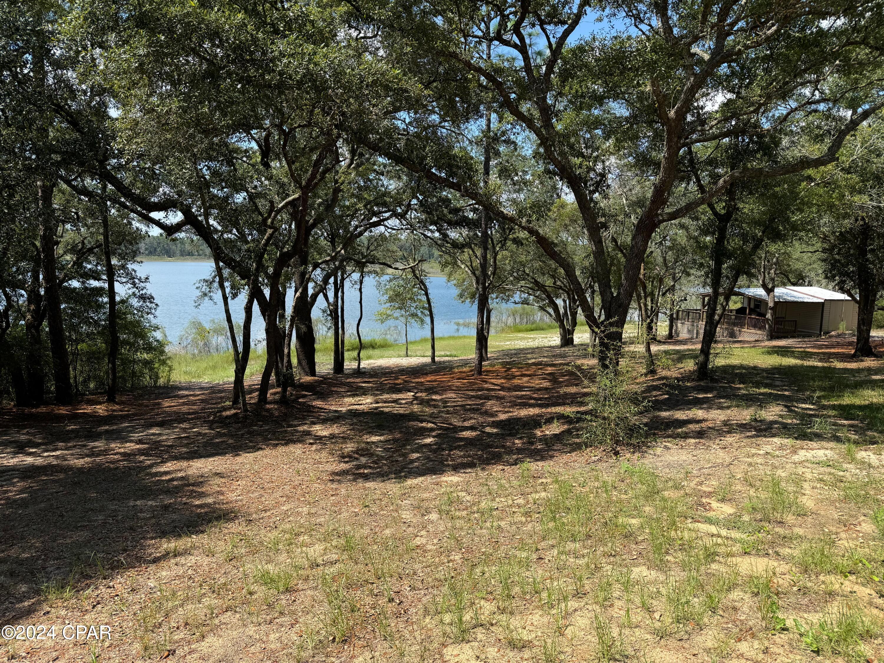 STUNNING WATERFRONT LOT on Spring Lake in Southern Washington County, FL, featuring 150 feet of pristine, sandy beach. The upper area is beautifully shaded by large oak trees, perfect for enjoying warm sunny days. 
This vacation homesite includes a 24 ft by 48 ft RV port built in 2021, which currently houses a lightly used 48 ft Jayco fifth wheel camper with four slideouts (please note: while the camper is included with the property, it is not part of the sale price). Additionally, there is a storage building located midway to the lakeshore which offers extra seating and dining spaces with lovely views of the water. Don't miss this little slice of paradise!!!