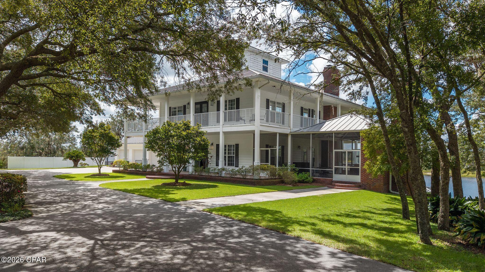 There are properties, and then there are places that quietly reorder your sense of what home can mean. Positioned at the crown of its own private peninsula on freshwater River Pond, this extraordinary Southern estate commands 360 degrees of unobstructed lake views across 82 ACRES of unspoiled Florida landscape and waves, just twenty minutes north of Panama City, yet worlds away from the ordinary. Five acres within carry highway frontage and commercial zoning, making the possibilities here as expansive as the horizon itself.

The arrival alone sets the tone. A canopied road lined with century-old live oaks, their branches heavy with Spanish moss, draws you toward a 7,200-square-foot residence that feels less like a house and more like an inheritance. Built like a fortress with poured concrete construction and dressed in classic white with red brick accents, the home is as enduring as the landscape that frames it.

Three levels of refined living unfold with a rare sense of intention. Wrap-around porches grace every floor, each one an invitation to pause, whether you're watching the morning mist lift off the water or following a sunset as it dissolves into the lake. Ten-foot ceilings run throughout all three levels, and a full-size elevator ensures every space in the home is effortlessly accessible.

On the main level, the expansive kitchen anchors the heart of the home with quartz countertops, an adjacent bar, and a generous walk-in pantry. The living room centers on a fireplace and opens through French doors to the covered porches and their sweeping waterfront panorama. A screened summer kitchen extends the entertaining possibilities seamlessly outdoors, while a formal dining room and a cozy sitting room-equally suited as a private study, speak to the home's thoughtful floor plan. A powder room on the main level is also easily accessible for guests. 

The upper floor is devoted to rest and retreat. The primary suite offers a soaking tub, walk-in shower, double vanities, and a custom walk-in closet of considerable proportion. Two additional bedrooms, two full baths, a dedicated laundry room, and direct porch access overlooking the oak-lined grounds complete the upper level.

The lower level challenges every assumption the word ''basement'' carries. With 2,000 square feet, ten-foot ceilings, a full second kitchen with an oversized island, a living room anchored by its own fireplace, a dedicated home theater, and two additional bedrooms and two baths, this floor functions as a fully self-contained retreat, ideal for multigenerational living or a home in itself for guests. French doors open directly to the covered porch to an open lawn. This area would be perfectly suited for a lakefront pool and also offers a convenient half bath under the covered porch. The lower level of this home would be an incredible entertaining space for family gatherings, pool parties and more! An additional heated/cooled 1,090 square feet of storage is also accessible from the lower level.

To speak of this property only in terms of the home would be to miss its greater gift. The freshwater lake invites fishing, water skiing, and long, unhurried afternoons on the water. The acreage beyond the home accommodates ATVs, side-by-sides, and the full breadth of an outdoor life. A detached three-car garage and circular motor court provide practical elegance at the entry. Impeccably maintained by its original owner since construction, every detail of this estate, from its remarkable landscaping to its poured concrete bones, reflects a standard of stewardship rarely encountered.

To own an entire peninsula is to own something genuinely irreplaceable. Estates of this scale, this setting, and this integrity are rare and to own this kind of paradise will stay in families for generations to come.