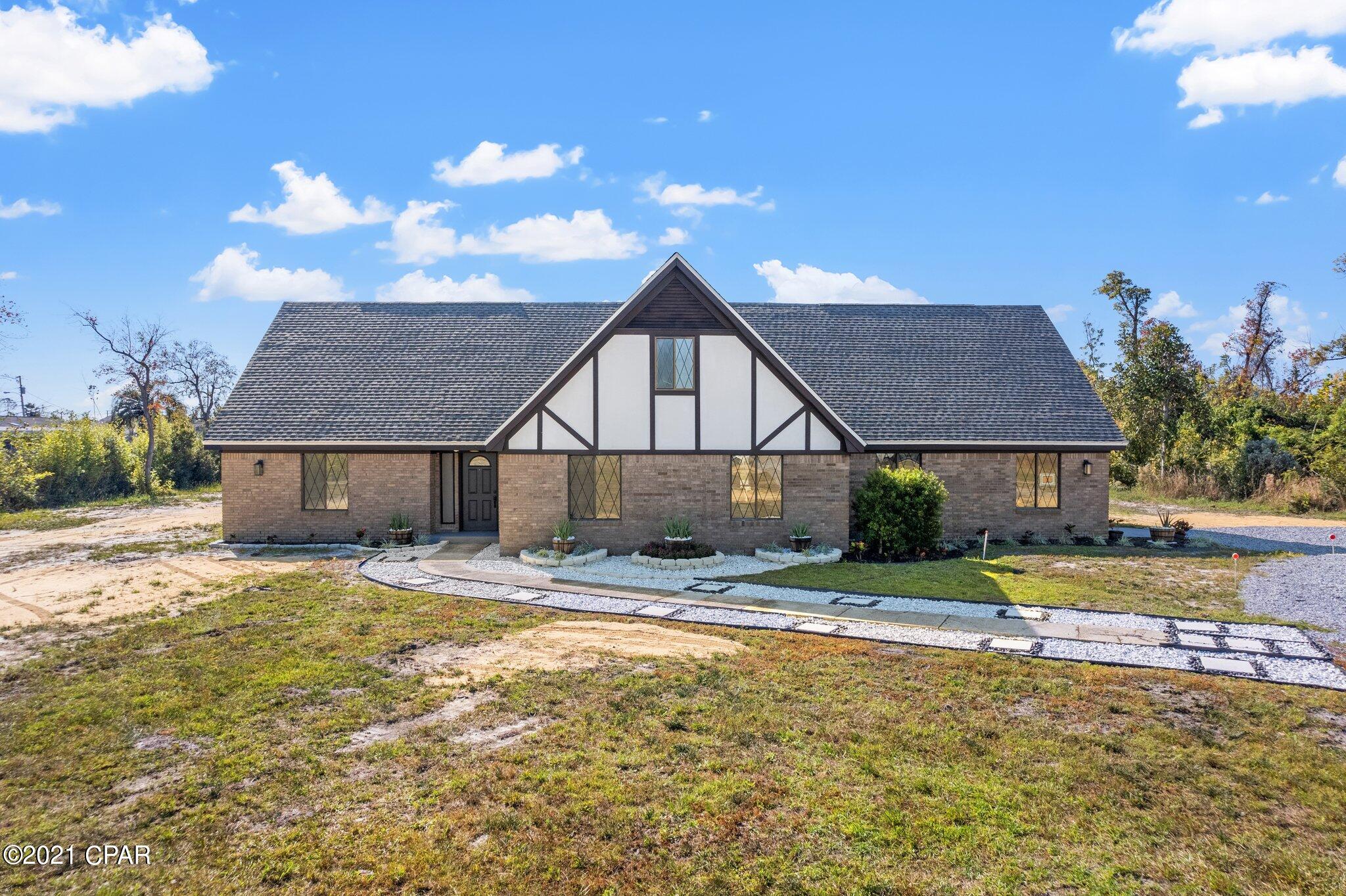 Welcome home! Your new home is sitting on over 2 acres of freshly cleared land and gravel driveway. This newly renovated home is across the street from the Callaway Bayou and just a short drive to the Tyndall Air Force Base, retail and dining options, Downtown Panama City, and U.S. HWY 98. Walking through the front door you will be greeted with an impressive hand painted tile floor and white wood paneling in the foyer. Throughout the remainder of the home  there is new luxurious water resistant vinyl flooring. This home features custom Tudor style windows. The open floor plan showcases an impressive stone fireplace, vaulted ceilings, and a first floor Owner's Suite.  Recent updates include a new garage door and opener, water heater, stove, and a new beautifully landscaped exterior. Moving into the kitchen you will be met with a surplus of natural light, highlighting the beautifully refinished cabinets and granite countertops. Tudor style sliding glass doors will lead you to a large enclosed porch overlooking the backyard. The Owner's Suite is located on the first floor with an ensuite bathroom, opening up with a Barn door, including a large soaking tub and walk-in shower. Proceeding upstairs, brings you to the additional bedrooms and bathroom. This home offers an attached, oversized  one car garage with a half bath and extended driveway. In the back of the property there is a refortified massive detached garage/workshop with room for a boat. This is a must see property, and we are expecting multiple offers. Schedule a showing today before this gem is gone!