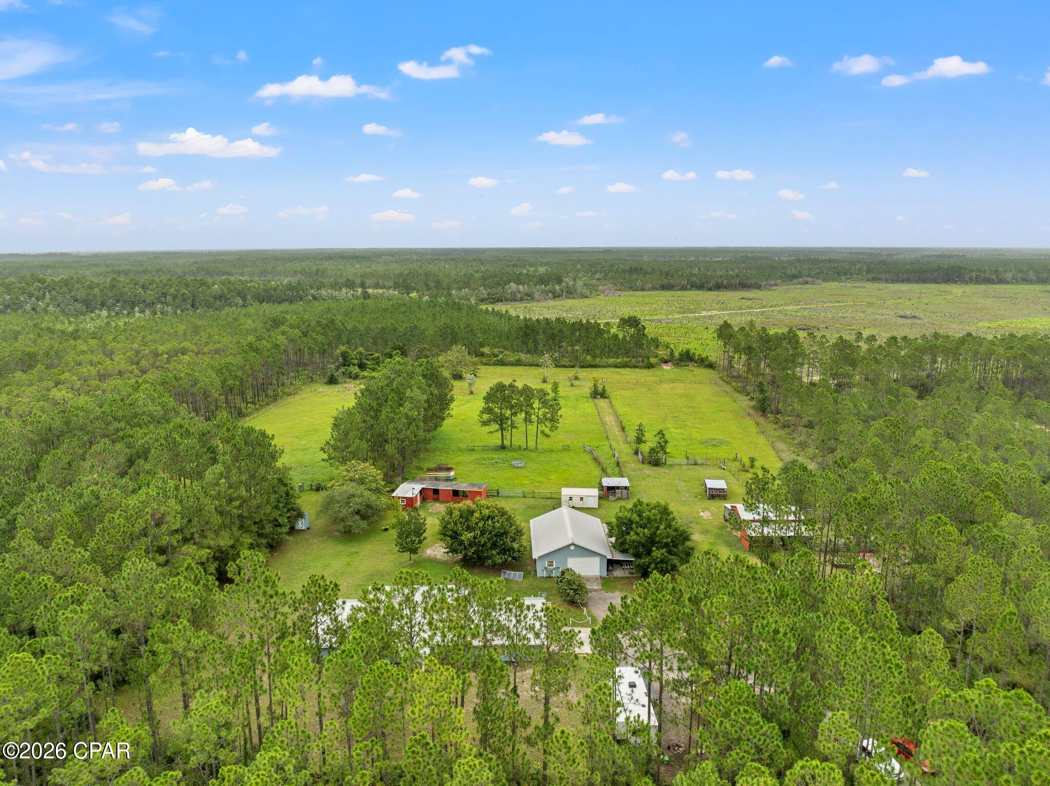 9140 Steel Field Road: Where 11+ acres of privacy meet the convenience of coastal living. Located less than 10 miles from the sugar-white sands of Panama City Beach and just a short drive to Scenic 30A, Margaritaville, and ECP International Airport, this unique property offers the best of both worlds.

The 3-bedroom, 2-bath home features over 2,100 square feet of heated and cooled living space with a functional split floor plan, spacious kitchen, great room, family room, garage, and additional climate-controlled storage room. Tile and plank flooring run throughout the home, complemented by a metal roof, covered back porch, and full-size laundry room with utility sink.

Ideal for farming, livestock, or equestrian use, the property includes two barns, stables, fenced pastures, corrals, a partially cooled workshop/butcher shop, storage shed, detached solar-powered garage, and an underground storm shelter.

With Conservation Habitation zoning, potential to be subdivided into two parcels, and future land use designated as Village Center allowing certain commercial uses, this property offers exceptional flexibility for homeowners, farmers, and investors alike.

Rarely does a property combine acreage, privacy, development potential, and proximity to the beach like 9140 Steel Field Road.

All measurements are approximate. Buyer to verify.