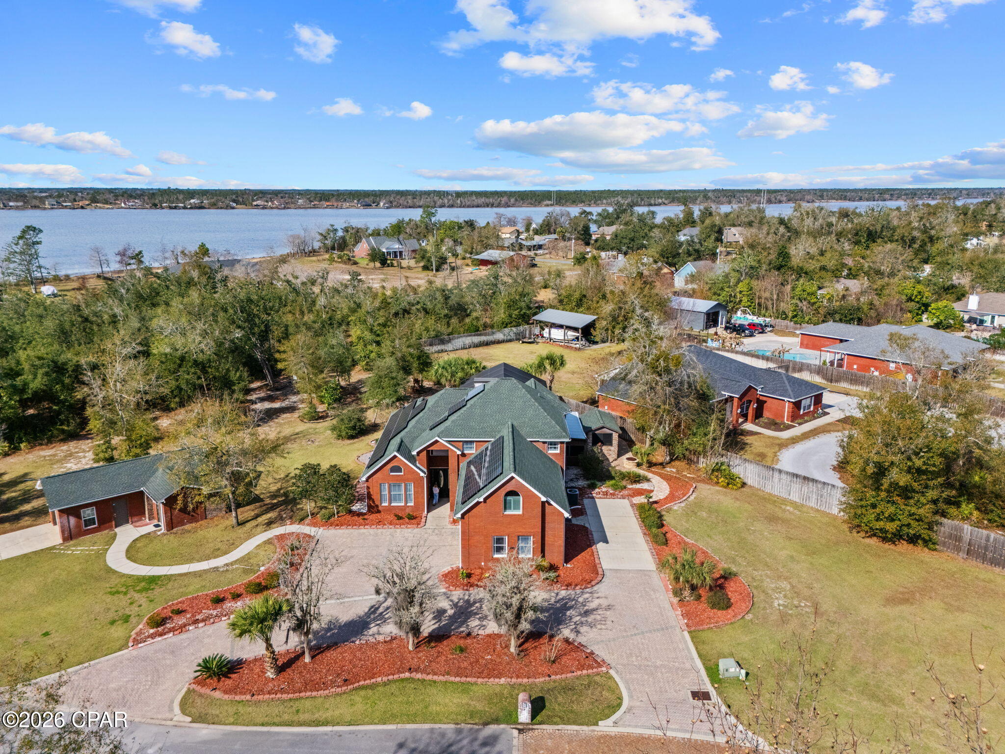 Discover an exceptional privately gated estate on Deer Point Cove Lane, set within a small, private setting and crafted with impressive detail, functionality, and quality throughout. This red-brick residence is introduced by an elongated half-circle driveway, expansive RV parking, and a 2+ car garage wired for electric charging. A detached third garage adds even more versatility and includes a climate-controlled 2,000-bottle wine cellar with Vintage View and Sorbus racking, plus a fully equipped 11×6 secure storage and firearms room.
Also available for sale is a separate half-acre, fully buildable lot (estimated $125K value) already improved with power, offering opportunities for future use or added privacy. Additional exterior features include 58 solar panels with two Tesla Powerwalls, a sprinkler system, private Econfina well, septic, security cameras, Ring doorbell, hardwired pathway lighting, Nest thermostats, and two HVAC systems.
Inside, the main level features ceramic tile flooring, a newly remodeled kitchen, and an extra-large island topped with an exotic marble-granite hybrid that extends into a full-height backsplash. The GE Café Signature Series appliance suite and Italian copper ductless range hood create a striking focal point. The grand living room showcases 20-foot ceilings and overlooks the saltwater pool and hot tub, supported by pool pumps, filtration system, and gas heater that are less than five years old.

Outdoor living includes two dedicated entertainment areas. The first is a fully outfitted pool house kitchen with a fireplace, bar area, refrigerators, microwave, and sound system. Across the patio, the second outdoor kitchen includes a grill, stovetop, wine fridge, refrigerator (plumbed for an icemaker), prep sink, ceiling fan, and its own A/C unit.

The main-level owner's suite features coffered ceilings, a sitting area, and double French doors leading to the pool area. The remodeled bath includes live-edge granite counters, vessel sinks, a soaking tub, extensive storage, and a remarkable 12-foot shower with five showerheads.

Upstairs, a beautifully updated full bath showcases live-edge granite, oval vessel sinks, a glass-enclosed tub/shower, and frosted glass barn doors. Four additional bedrooms offer generous closet space, including one en suite with a balcony overlooking the pool. The oversized bedroom above the garage provides excellent potential for a media room or other flexible use.

This estate offers extensive upgrades, thoughtfully designed spaces, and modern systems, creating a standout opportunity near Deer Point Lake.