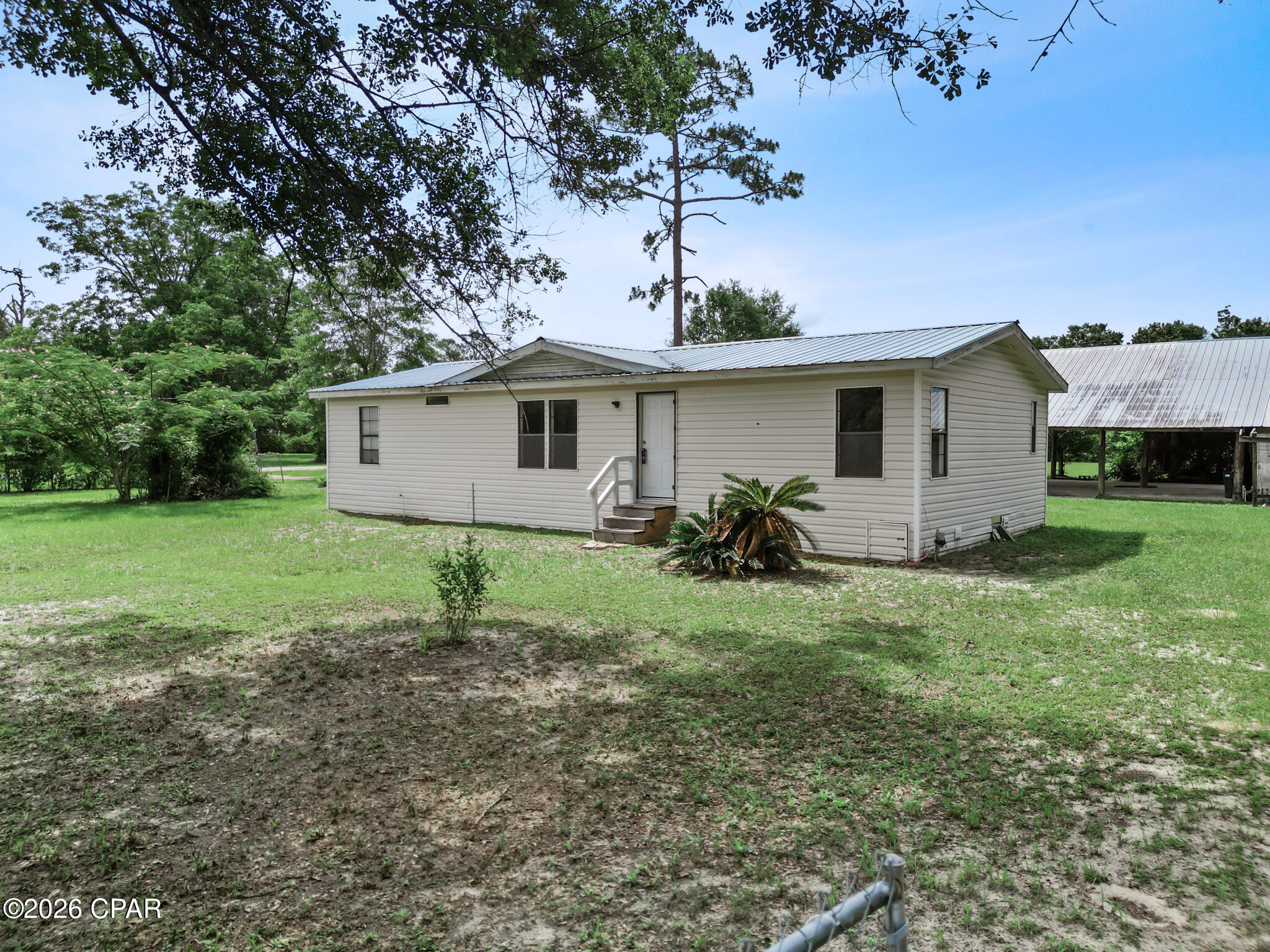 10461 NW 1st Street in Bristol, Florida offers the space, flexibility, and North Florida lifestyle you've been searching for. Situated on approximately 1.29 partially fenced acres, this 3-bedroom, 2-bath home provides room to spread out, enjoy the outdoors, and make the property your own.

This 1,152-square-foot home features a metal roof, vinyl siding, vinyl plank flooring and carpet throughout, and a comfortable layout designed for everyday living. The kitchen includes a bar area, electric stove / oven, refrigerator, and opens to the dining area, making it easy to stay connected while preparing meals or entertaining guests.

The living room provides a welcoming gathering space and features a fireplace that is currently capped off. The spacious primary suite includes two vanities, a soaking tub, and a separate stand-up shower, creating a private space to unwind after a long day. Two additional bedrooms and a guest bathroom with a tub/shower combination provide flexibility for a variety of needs.
Step outside and enjoy the back porch overlooking the property. A concrete pole barn with electricity offers excellent space for projects, equipment storage, hobbies, or outdoor work, while the attached utility shed provides even more storage options.

With approximately 1.29 acres, this property offers room to enjoy today and potential opportunities for future use. Buyers should verify with the appropriate county and regulatory agencies any plans for additional structures, homesites, or property improvements.

Location adds even more value to this property. You'll be approximately one hour from both Tallahassee and the white-sand beaches of Mexico Beach, about 15 minutes from the Apalachicola National Forest, and only minutes from the Bristol Boat Landing. Whether you enjoy fishing, boating, hiking, exploring nature trails, or taking day trips to the Gulf Coast, you'll appreciate having outdoor recreation and local conveniences within easy reach while still enjoying the relaxed pace of North Florida living.

If you've been searching for an affordable property with acreage, outbuildings, and room to enjoy the outdoors, this could be the opportunity you've been waiting for. Schedule your private showing today and see everything this Bristol property has to offer.