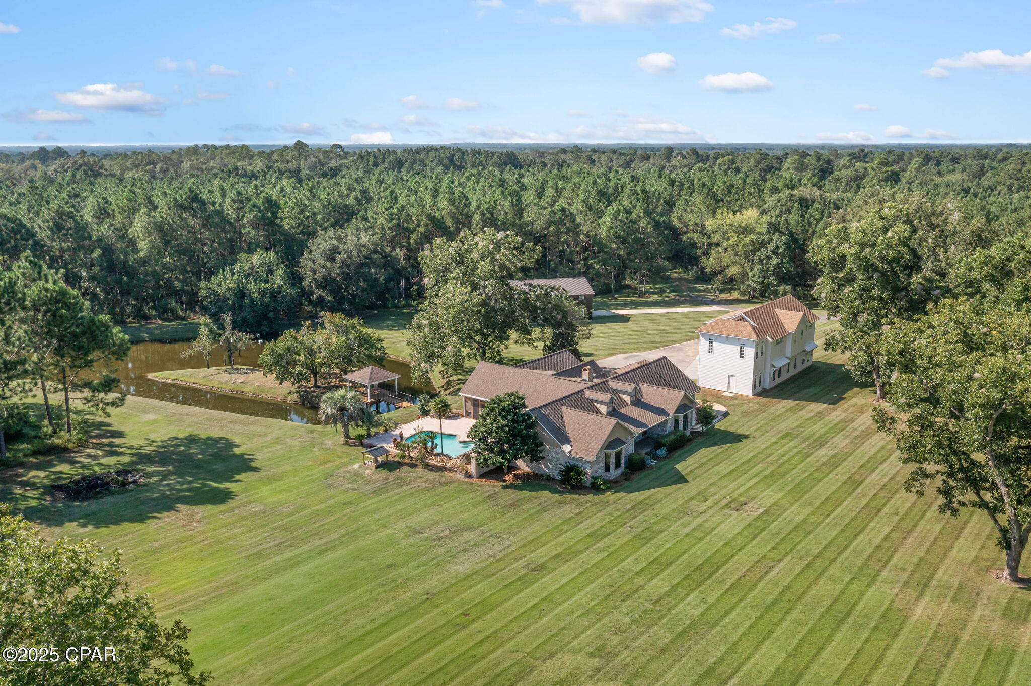 Welcome home, where attention to design and detail create a residence that is both elegant and inviting. This 3-bedroom, 2 ½-bath estate home rests on over 31 acres of beautifully maintained grounds featuring mature trees, multiple ponds, and lush landscaping. A private gate and long paved driveway set the tone for the peaceful retreat that awaits within your very own private oasis. Outdoors, you'll find numerous spaces to relax and entertain, including a screened lanai with TV setup, a covered pavilion overlooking the pond, and an inground pool with a custom stone slide—perfect for gatherings with family and friends. Inside the main home, an oversized living room welcomes you with soaring 14-foot cathedral ceilings accented by custom wood beams, built-in cabinetry, and a cozy gas fireplace. Additional highlights include a Florida room with panoramic views of the pool and pond, a formal dining room, office nook, and a spacious eat-in kitchen with island seating. The primary suite is a true retreat with custom cabinetry, dual sinks, granite countertops, a walk-in shower with rain head and stone floors, a jetted tub overlooking the pool, a massive walk-in closet with built-ins, and direct access to the pool and patio area. Adding to the estate's appeal is a newly constructed luxury carriage house, designed with comfort and style in mind. Offering 1,668 sq. ft. of heated and cooled living space with  2 bedrooms (including a master and a bunk room), 1 1/2 bath, a gorgeous custom kitchen with island, durable vinyl plank flooring and an attached 4 car garage. Perfect as a private guest retreat or multi-generational living space, this carriage house provides both independence and sophistication for visitors. For those seeking even more options, the property also includes a 60x36 black metal barn with the framework ready to be transformed into additional living quarters or a dream workshop. With endless opportunities for equestrian pursuits, cattle, or simply enjoying the outdoors, this estate offers both luxury and versatility just west of Chipley off Hwy 90.
