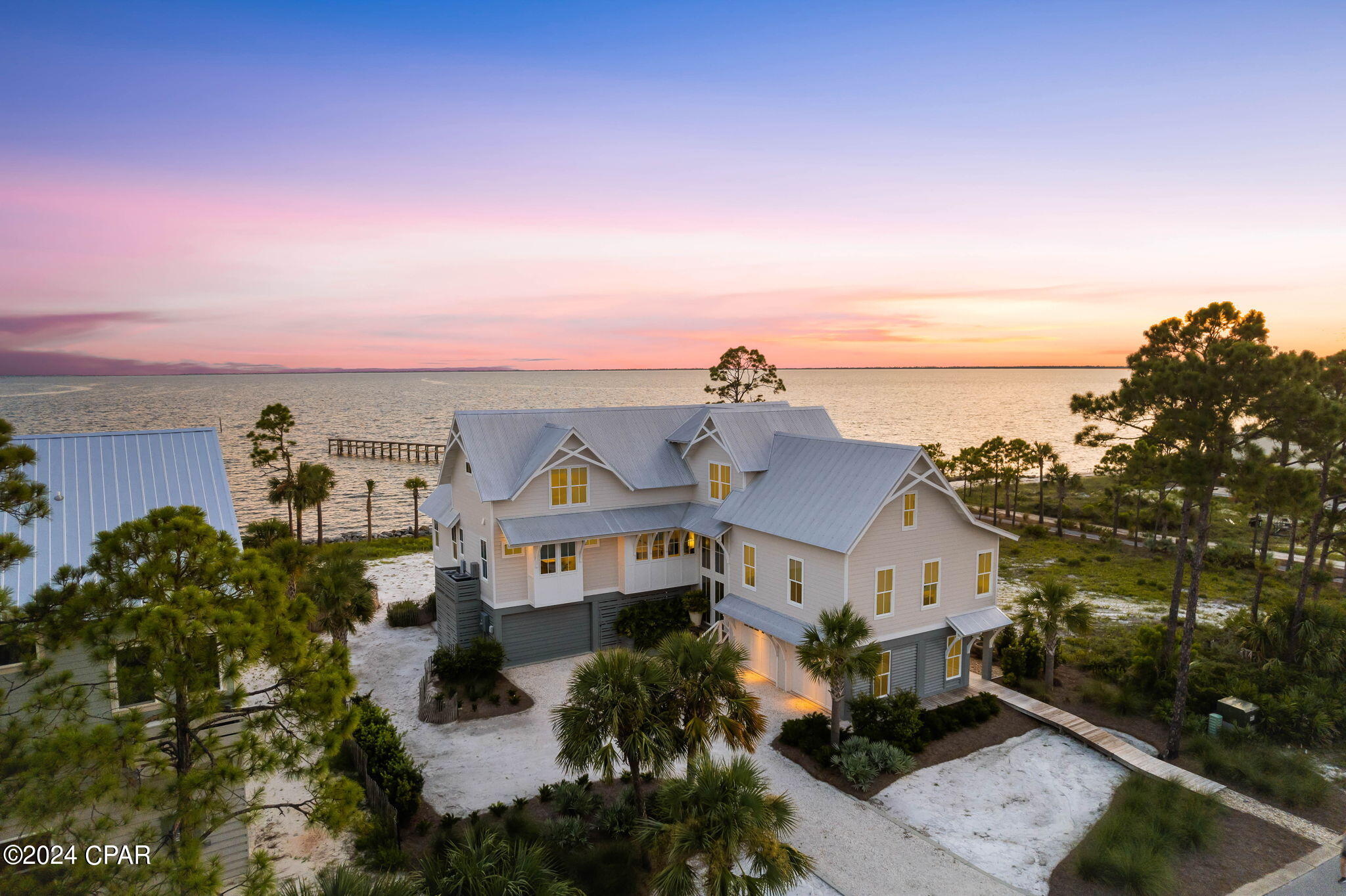 This custom-built beach house offers bright, spacious interiors and breathtaking views of St. Joseph Bay. With top-tier fixtures and finishes, it's the ideal home for those seeking a waterfront lifestyle, complete with a private sandy beach in the backyard. The first floor features a generous entertainment area, complemented by a fully-equipped outdoor kitchen and covered deck, perfect for relaxing, entertaining, or grilling up the catch of the day. A bar area invites socializing over icy drinks, while a hammock and surround sound system enhance relaxation both inside and out. The three-car garage and ample storage space ensure all your water toys are easily accessible, maximizing the enjoyment of your private waterfront haven. An elevator smoothly transports you to the beautifully furnished second-floor living space, where large windows frame stunning views of the white sandy beach, swaying palm trees, and the tranquil waters of St. Joseph Bay. The light, open living area features timber beams and wood cabinetry, reflecting the natural surroundings. The family-sized kitchen is equipped with a full suite of gourmet appliances, including an oversized gas range, double oven, and wine refrigerator, while a sleek quartzite-topped island offers casual dining space. The formal dining area is perfect for larger gatherings and celebrations. The second-floor sitting area, warmed by a built-in gas fireplace, offers spectacular views, with French doors opening onto a spacious deck furnished with deep cushioned sofas, perfect for enjoying the gentle breeze. A well-designed office space allows you to balance work and leisure. Each generously sized bedroom comes with its own private bathroom, ensuring privacy and convenience, even when hosting guests. You can fish from the community dock or take a quick ride in the golf cart to the community pool.