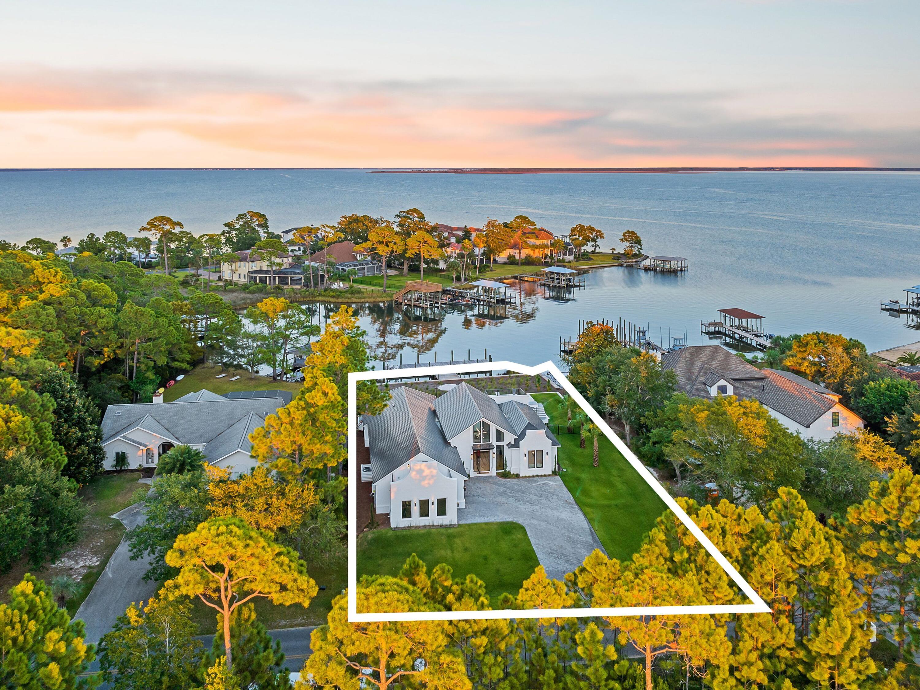 Boaters and entertainers will want to check out this stunning new bayfront home with its own private pool and carriage house. It goes beyond the norm with a deep-water dock, one of the last in Driftwood. The 60-ft. dock can easily accommodate a larger boat and offers direct gulf access via Destin Harbor. This contemporary home has a refreshingly modern facade with clean minimalist lines throughout, making good use of frameless custom glass windows and doors. The design boasts generous indoor and outdoor areas for entertaining, including 2,300 square feet of shell stone on the rear patio. The 30x12 pool provides a focal point for gatherings and has a rear balcony for elevated views across the sheltered waters of Choctawhatchee Bay. The open floor plan flows from the attached three-car garage through a series of living and dining areas to the covered porch and stunning waterfront. This house has a full outdoor covered kitchen with a built-in grill, flat-top griddle and refrigerator. The carriage house serves as the fifth bedroom and has its own private balcony for guests to enjoy outdoor living as well as a small kitchen area with sink, refrigerator and counter space for small appliances. The home has many exceptional design features including metal framing for the airy cathedral ceiling and a stunning 10x6 pivot front door. Mortar-smeared brick adds character along with custom-built cabinetry throughout the whole house. The chef's kitchen makes a dramatic statement with its chocolate and white cabinets, walk-in pantry, special order Italian oven, oversized island and a host of high-end stainless appliances including an ice maker for those days out on the boat. There's an eye-catching linear fireplace that extends 10 feet in the floor-to-ceiling 22-ft. wall of tile in the lofty sitting room and a dedicated glass wine room for your reds and a 30-bottle glass-front wine refrigerator to keep your whites chilled until the cork is popped. Five bedrooms include a vast master suite with a boutique-worthy walk-in closet and spa-like garden tub and master shower that will make you feel that you've arrived at your favorite spa. Bathrooms all boast frameless showers and tankless floating toilets to maintain the minimalist effect. This one-of-a-kind home is sold partially furnished and combines serene bayfront living and views of incredible wildlife with visits from dolphins and friends. This home is so new it still has many months of builder warranty. All this and Sandestin's noteworthy shopping, dining and golf, only minutes from 30A and those beautiful white sandy beaches.