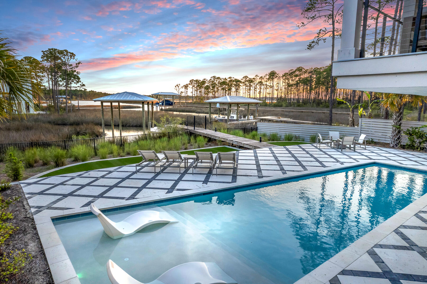 Take a slow drive down this quiet street just minutes from 30A's bustle and beaches but worlds away. Perfectly positioned along the water's edge and sitting high above a captivating bayou, you'll find this architecturally significant, modern coastal masterpiece. Every element is visionary yet functional, including fabulous furnishings (most remain).

Built in 2022 and improved by the current owner, this home is timeless in detail and rich in amenities. Over ½ acre of outdoor space includes a full-sized pool with tanning ledge, highlighted by grass-lined pavers, and surrounded by native landscaping with a clever AstroTurf lined play yard. A private wooden path leads to your private boat slip over deep water and all voyages lead through wispy reeds and romantic marshes to the bay and beyond.  

A drive-under garage for two cars plus all your toys includes a pre-engineered elevator shaft, ready for your addition of an elevator should you so choose and a recently added 350 sq ft climate controlled storage! A brand new washer and dryer are conveniently located to easily launder wet towels!  The expansive main floor, cable-railed balcony with outdoor kitchen perfectly captures rose-hued skies, bounteous bayou wildlife, and meandering waterways. 

A stunning two-story entry way, incorporates the home's signature cable-railed staircase and an edgy light fixture, hinting at the detail in what's to come. Leading to the open concept living area, you'll pass a newly equipped pantry with custom cabinetry and ice maker, a stylish powder room, and a recently redesigned wine bar with wine cooler and faux brick detail.

From the vast living/dining/kitchen under 14' wood-paneled ceilings, all eyes lead through tall glass-sliders to breathtaking water vistas. Pause, but don't miss the custom kitchen with stylish painted cabinetry, edgy hardware, quartz counters, KitchenAid appliances (including a 5-burner gas stove and double refrigerator drawers), and stylish lighting. The oversized island with seating for 8, invites people to stay awhile. The 8-person dining area occupies its own waterfront perch. The relaxed living area begs for curling up with a good book on a rainy afternoon.

Four bedrooms on the main floor include two guest rooms with their own unique charm, as well as a junior suite with bayou views and an ensuite bath. The main bedroom suite is a retreat unto itself with calming water views under clear blue skies. With coffered ceilings, barn doors, and oversized closet plus a full-sized laundry with washer/dryer/folding, you won't want to leave its comfort. The main bedroom bath is equally impressive with dual floating vanities, marble finishes, dual shower heads, and a deep soaking tub. 

On the third floor, it's a party! Time to shoot pool and jam to some tunes, all paths lead upstairs. Equipped with its own wet bar and serviced by a powder room with floating cabinet, it's a celebration room and hideaway all in one. 

No HOA adds to the appeal of this unique property. Please verify all information. And please, call for a private showing!