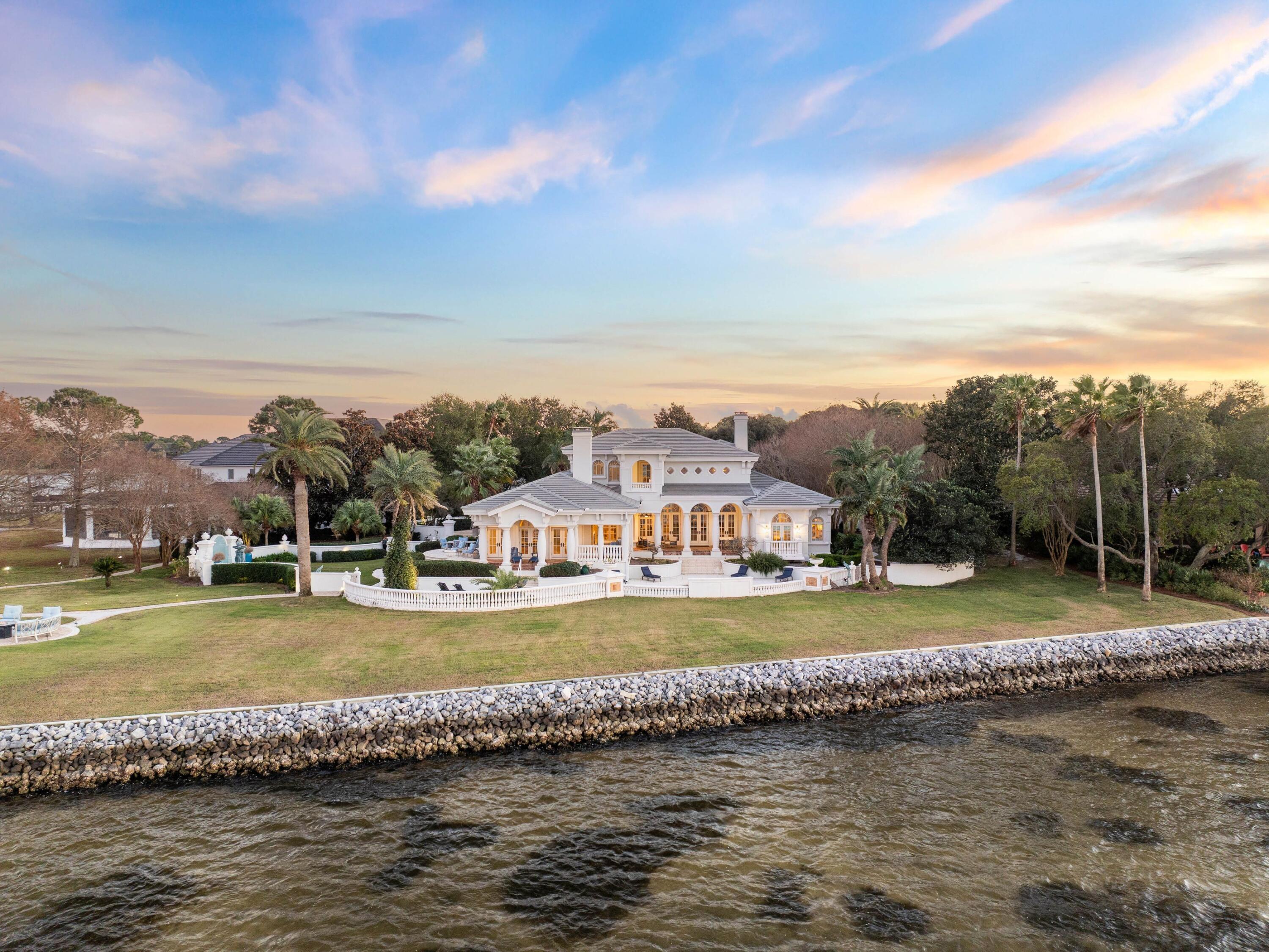Set across nearly an acre and a half with 385 feet of uninterrupted bayfront, this estate feels like its own peninsula of stillness and sky. The grounds sweep outward in all directions, shaped by mature gardens, cypress-lined privacy, and water that curves around the property in a wide, shimmering arc. From this vantage, sunsets arrive in full panorama, casting shifting bands of color across Choctawhatchee Bay and giving the residence an atmosphere both cinematic and serene. Designed by Massey-Ledo Studio Architects, the Mediterranean-inspired home balances classical architecture with modern ease. Arched openings, wrought-iron railings, and interior columns lend a sense of sculpture, while generous windows usher in natural light and frame horizon-to-horizon water views from the main gathering spaces. The floor plan moves with quiet intention, opening to the outdoors at every turn and encouraging a rhythm of living that feels uniquely tied to the bay. Thoughtful amenities, including a wine room, cedar-lined closets, a whole-home water filtration system, a dehumidifier, and integrated sound, complement five bedrooms and five baths. The gourmet kitchen features Thermador appliances, dual ovens, a broad cooktop, granite surfaces, and a dedicated KitchenAid icemaker. A signature sunken bar anchors the family room, positioned to watch the water shift with the tides. On the first floor, a steam room offers spa-style respite.
Outdoors, the estate feels both cultivated and natural, with manicured gardens, a fountain, and a tranquil bayfront pool. Brick pavers define the walkways, drive, and sunset patio, creating a warm textural contrast to the water beyond. The deepwater dock is a true rarity, upgraded with new Tru-Flow decking, a 42-by-17-foot boat slip with lift, two jet-ski lifts, dredged access, and the capacity to accommodate a 38-foot cruiser. Evening brings a transformation as newly enhanced exterior lighting softly illuminates the trees, gardens, and waterfront. Recent improvements include new landscaping, featuring expanded azaleas and mature cypress plantings, an upgraded irrigation system, updated HVAC, a 2021 concrete tile roof, tandem tankless water heaters, a Generac generator, Ring exterior cameras, and enhanced lighting controls.
Meticulously cared for and architecturally significant, 400 Coleman Point stands as one of northwest Florida's most compelling bayfront estates, offering rare privacy, deepwater access, and a horizon of water that feels endlessly its own.
