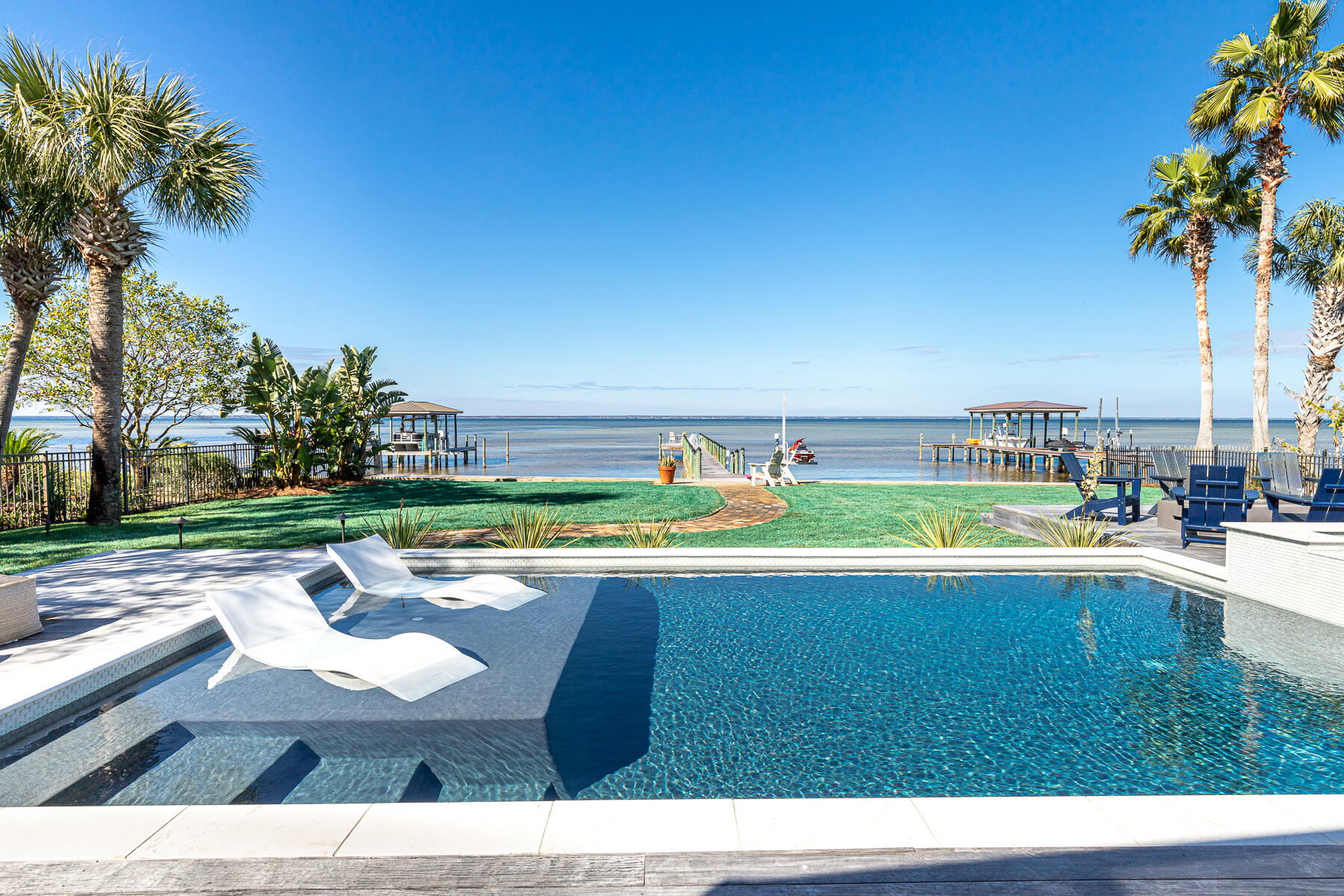 Sophisticated bayfront renovation and no HOA. Single-level living in a compelling floorplan that perfectly mingles privacy and invitations to gather. Curb appeal is unmistakable with a deep winding drive that leads to a pristine white home with a welcoming courtyard entry. Flexible design and a seamless floor plan endue an entertainer's enclave or a relaxed family estate. Sparkling bay views are first captured within the glass-paned front doors and then draw you in through the dramatic living area highlighted by a 12' coffered ceiling. An expanse of glass fully retracts, leading to a newly added screened-in porch and the bay beyond. A sprawling backyard is highlighted by a recently constructed heated pool and spa with a sunken fire pit. Tastefully framed in Epay wood decking, the backyard oasis is professionally landscaped in a minimalist aesthetic. Sunsets seem to linger longer over an extended-length dock complete with sound system. Interiors are memorable, as are the parties. Circa Lighting is tasteful yet edgy. Designer furnishings are colorful and relaxed. Seller is willing to convey some furnishings in a separate sale. The recent full house renovation consists of a custom wet bar, painted dark gray with open shelving and lower cabinetry. The wet bar includes a Sub-Zero, 180 bottle wine fridge, and separate icemaker. The renovated kitchen packs innovative storage into a very workable, modern space with marble counters, a subway tile backsplash, a Wolf 8-burner stovetop, and a double gas oven Liebherr fridge with double freezer drawers, and a KitchenAid dishwasher. New LVT flooring throughout most of the home fades from ash to taupe depending on the light and ensures durability and ease of maintenance for years to come. The master suite includes two spacious closets plus a recently added built-in entertainment cabinet with additional hanging space and a chest of drawers. The comfortable in-house guest bedroom and renovated bath encourage lazy mornings. An office boasts its own water views and eye-catching, functional built-ins. An ultra-private guest casita with bath rests just off the courtyard with its own entry. Situated within close reach of the kitchen, the outdoor grilling station becomes an extension of the kitchen and integral to daily living. A short boat ride guides to dining on the water or a quick drive leads to the beach.