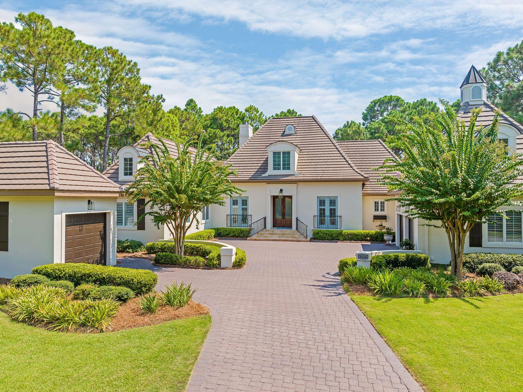 Nestled in mature pine trees and overlooking the Burnt Pine Golf Course, this magnificent estate offers 4,810 square feet of carefully maintained living space along with a three-car garage and a heated pool within a screened lanai. From the sweeping driveway, the French chateau-style architecture delivers jaw-dropping curb appeal. Steep gabled roofs punctuated by dormer windows add to the sense of grandeur. A light and airy foyer welcomes you inside, with three sets of double doors drawing you toward the shimmering waters of the outdoor pool. Pass through the formal dining room with lighted display cabinets and check out the sitting room with a feature fireplace with custom mantel creating a natural focal point. Textured walls, wood floors, Venetian plaster, barrel and beam ceilings and tongue and groove paneling add elements of interest to the tasteful decor. The 44-foot-long Ferrari of kitchens deserves its own fanfare with stunning marble countertops and a feast of high-end appliances. The pitch-sized island includes an ice maker, sink and dining table, while the adjoining family room has its own wine fridge. Located on an oversized lot and buffered by greenery, this secluded home enjoys peaceful views of the lake and 10th fairway. The landscaped yard is laid mainly to turf, with mature trees providing dappled shade. This outdoor haven is fully equipped for lazy days by the pool and spa, entertaining guests easily from the outdoor kitchen. It boasts a built-in wood-fired pizza oven along with a sink and refrigerator. The vast screened-in living space has beautiful stone flooring connecting the outdoor dining area with multiple sitting areas. Hidden Sonance speakers deliver your favorite background music while lighted fountains dance and entertain after dark. Two spacious suites occupy the remainder of the first floor, and a lengthy hallway provides a suitable sense of arrival. The primary suite includes its own fireplace, sitting room and access to the pool. The walk-in closet segues into a dressing area with multiple built-ins providing customized storage. Beautiful tile elevates the master bathroom, which has a twin vanity, oval tub and hexagonal tile flooring in the walk-in shower. The guest suite has its own beautiful bathroom with noteworthy tile features. Two additional guest bedrooms are tucked beneath the hip roofline on the second floor. A separate staircase leads to a final surprise. A bonus room offers views in all directions, making it ideal to furnish as a private office or workout room. Additional features include a Hanish Water whole house purification system, a well water iron removal system, and Control4 home automation with monitored home security. This exclusive home is set behind private gates within the prestigious community of Sandestin. Championship golf, tennis, a marina, shopping, fine dining and live entertainment are all within easy reach by golf cart.