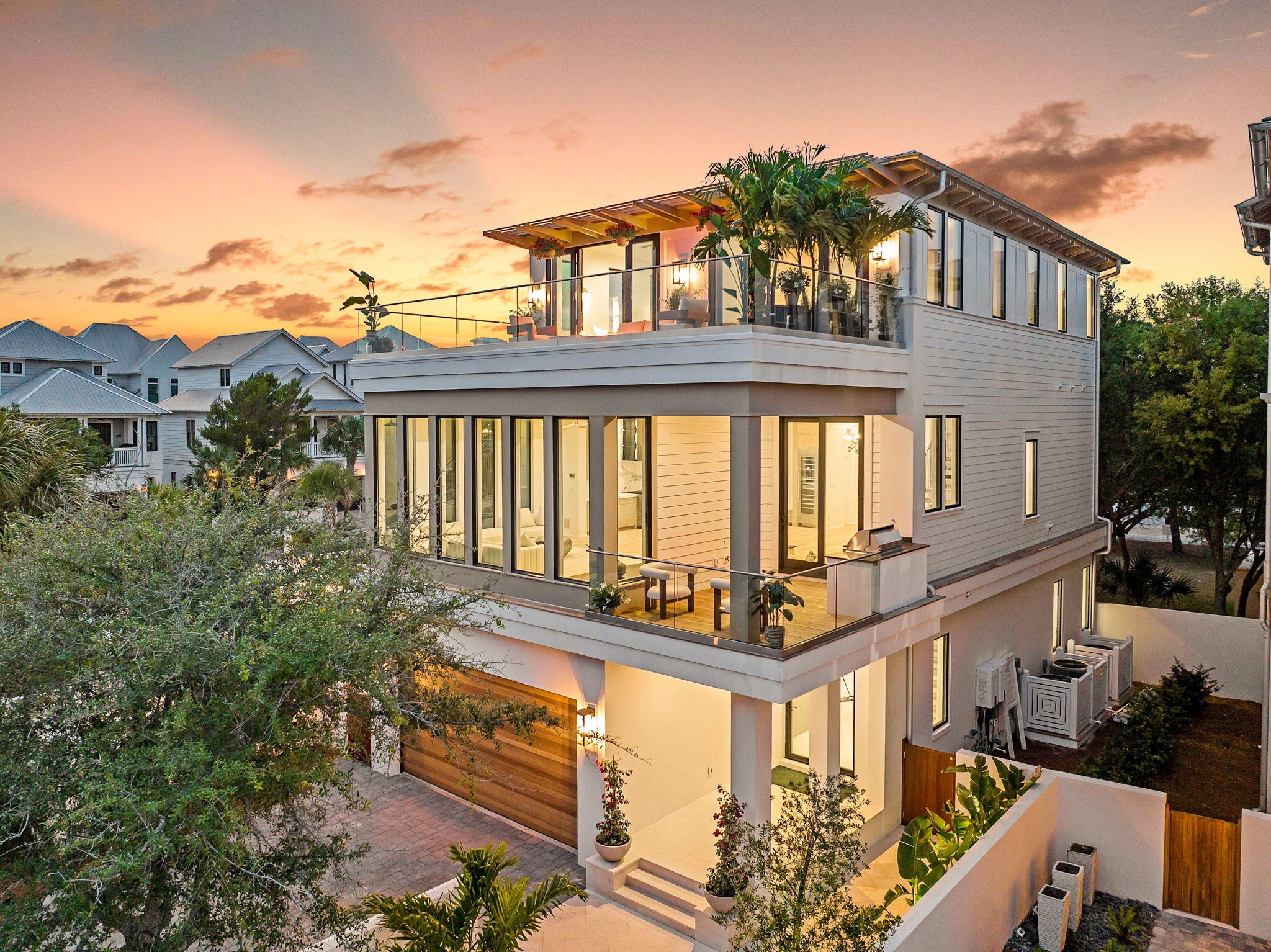 The Glass House is a striking new architectural statement in Seagrove Beach, completed in May 2025 within the private gates of Seanest Village. Designed by Gregory Jazayeri of GDJ Design and Ivana Jazayeri of IVA Design, and built by Lpkk, Petr Kasparek, this 3,967 square foot residence offers a rare balance of timeless craftsmanship and modern innovation, equally suited for refined vacation living or full-time residency. Built with concrete block construction on the first floor, the three-story home features five bedrooms, five and a half baths, and three spacious living areas, including double primary suites thoughtfully designed for flexibility and comfort. Ceiling heights soar with 10 feet on the first and third floors and nearly 12 feet on the main living level, culminating in a large rooftop terrace where Gulf views stretch beyond the treetops.

Inside, a state-of-the-art technology suite complements sleek custom finishes. An 85 inch display anchors the audio-visual system with immersive surround sound, whole-home WiFi, Alexa integration, and exterior security cameras. Custom white oak cabinetry, Thermador and Viking appliances, Kohler fixtures, and smart bidet toilets reflect an uncompromising standard of modern luxury. Offered furnished, the interiors blend clean lines with curated modern pieces, creating a ready-to-enjoy coastal retreat.

The first floor is anchored by a glass pivot door entry, leading to a guest suite, bunkroom with custom queen over twin bunks, two full baths, a lounge with wet bar, and shaded porch opening directly to the Seanest pool and boardwalk.

On the second level, walls of glass frame the shimmering pool while a peninsula fireplace connects the living, dining, and kitchen spaces. Culinary features include a chef's kitchen with Thermador appliances, a 48 inch Viking gas range, hidden oversized butler's pantry, and a 66 bottle glass wine display. A junior primary suite, laundry, powder room, and outdoor grilling porch complete this floor.

The third floor offers Gulf facing vistas from a morning bar and lounge, alongside the primary suite, a serene retreat with a glass display walk-in closet and spa-inspired bath featuring a freestanding tub, dual vanities, and a double shower. A second laundry space and an additional bedroom with bath nestled beneath the live oaks round out the level.

Residents of Seanest Village enjoy two vanishing edge pools, deeded beach access, and direct entry to the neighboring State Forest, all within walking distance of dining, shopping, and the new Greenway Station.