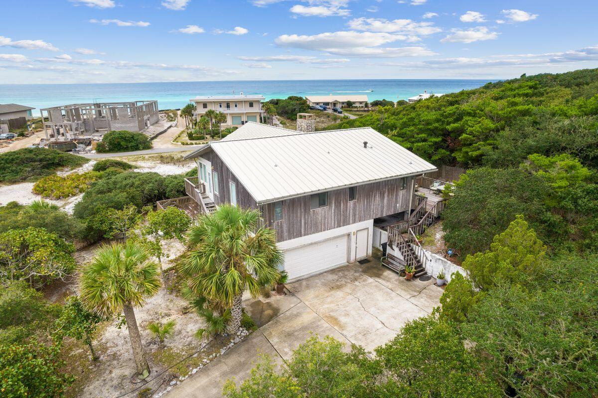 Nestled amongst an unspoiled green oasis with panoramic coastal views, this unique hideaway is located in the secluded community of Four Mile Village. Surrounded by the Coffeen Nature Preserve to the north and the Gulf of Mexico to the south, the serene neighborhood provides an idyllic locale for this commanding sanctuary. Tucked away on an elevated one-acre parcel, one row off the gulf, this home was designed to maximize the stunning views. Grounded with Old Florida charm, the open living space has a cathedral ceiling, soaring picture windows and tile flooring. It spills out onto a wraparound balcony, allowing nature to thrill all the senses. The expansive wooden deck is an elevated space for barbecues and entertaining or just enjoying the sounds of nature. The living room is bathed in natural light, which is ideal for those who enjoy being at one with their surroundings. It flows into a well-planned kitchen with gleaming hardwood flooring. The master bedroom is generously sized and on the main living level, while 2 additional bedrooms occupy the first level. Set in a gated community, this is a place for those who appreciate unspoiled nature. Neighboring Fuller Lake is a rare coastal dune lake offering 42 acres of fishing and tranquility. In contrast, there are plenty of amenities offered just outside the gates with upscale dining and shopping at Grand Boulevard and just a short distance to Scenic Highway 30A.