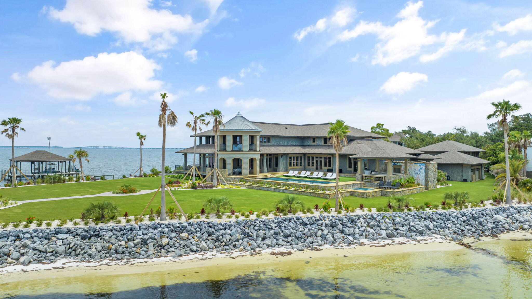 Enjoy the luxury of over 1,000 ft of waterfront on this Gulf Breeze property! Located in the highly sought after gated community of Peakes Point, this lavish and private 10,500 square foot home offers the best there is to offer both indoors and out. From the custom-designed bronze fixtures, to the sycamore and pear wood walls, the interior wow-factor is high! Modern amenities such as the fire suppression system, golf simulator/track room, generator, Control 4 Home Automation System, and hurricane rated impact doors and windows ensure comfort and security. Step outside to enjoy the beautiful views of both Pensacola Bay and Santa Rosa Sound from the yard equipped with an underground mosquito mister, upgraded landscaping, heated pool, hot tub, putting green, 2 jet ski lifts, 2 boat lifts,  and greater than 5,000 square feet of porches. Additionally, the estate boasts a guest house and ample indoor and covered parking. Situated on the western most tip of Gulf Breeze, this property is truly one of a kind and the epitome of coastal living!