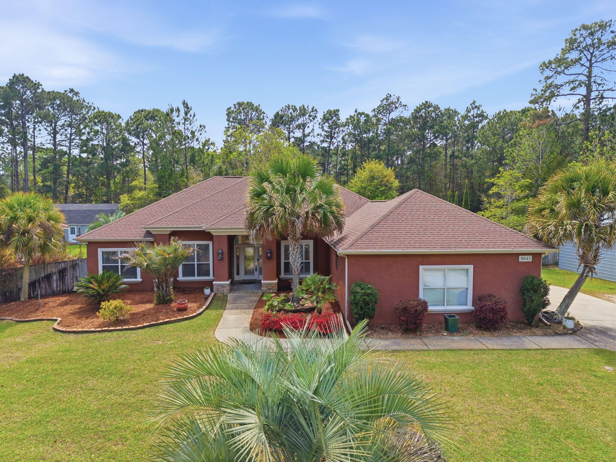 Welcome to this stunning, custom-designed retreat of a home - perfectly situated on 1.27 acres in the Whispering Pines community of Navarre. This 2,216-SqFt home offers a split floor plan with an open concept Main living space with accented wood beamed ceilings and pillars and beautiful, semi-polished travertine stone flooring that flows seamlessly throughout - ensuring a carpet-free, low-maintenance living experience. The heart of the home is a chef's dream kitchen, featuring a massive 3x10 granite island with breakfast bar, stainless steel appliances - including a gas powered stove - a farmhouse sink, and updated cabinetry. The dining room impresses with eleven-foot ceilings and an elegant wood-accented tray ceiling, while the spacious living room centers around a cozy fireplace and triple French doors that lead to your outdoor sanctuary. The primary suite is complete with a lighted, double tray ceiling, a private entrance to the backyard, and a spa-like ensuite bathroom featuring a massive walk-in travertine shower with standalone soaking tub, double vanity, and an oversized closet. Two additional bedrooms provide ample space for family or guests - one with double doors that open to the backyard. There's also a dedicated bonus room with a custom window seat that could serve as an ideal home office or playroom. Step outside to a backyard built for relaxation and entertaining, where a screened lanai overlooks a lush, tropical garden oasis, a semi-inground pool surrounded by a spacious deck, a 512 SqFt climate controlled hobby or workshop, and a custom-designed gazebo. Complete with a side-entry two-car garage and a detached steel carport with plenty of room for an RV or boat, this exceptional property offers the perfect blend of secluded luxury and modern convenience.