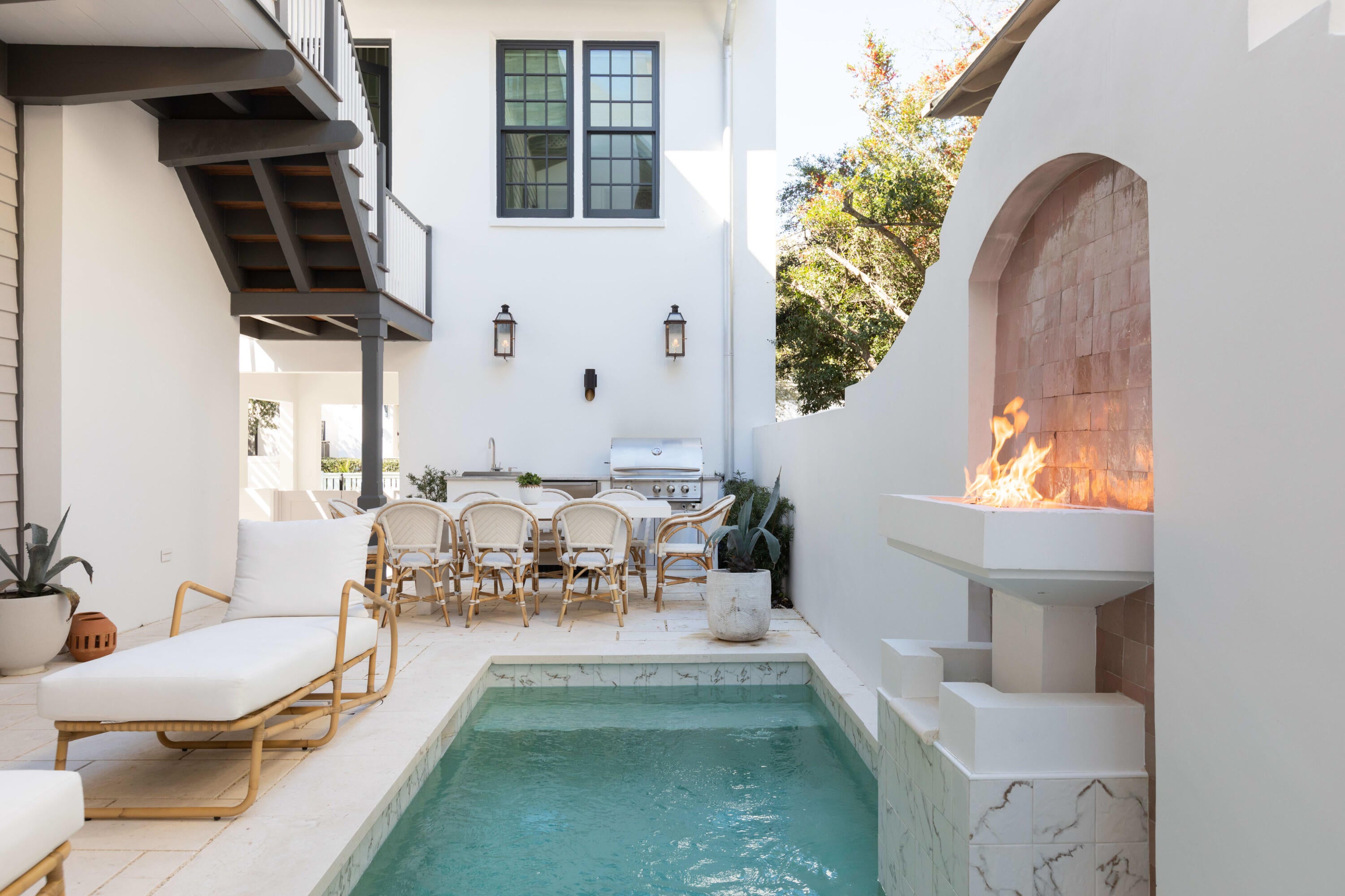 Distinctive architecture and interiors by Kate Marker Interiors define The Salty Rose at 49 Hamilton Lane in Rosemary Beach, Florida. Positioned along a charming pedestrian path near Town Center and the beach, this coastal residence offers four bedrooms, four full baths and one half bath across the main home and carriage house (2022), complemented by a private saltwater pool and summer kitchen.  Building upon the original one-bedroom home, Rosemary Beach's first town architect, Mark Tanney, returned to reimagine the property with an expanded residence, carriage house and garage. Inside, hardwood floors, exposed ceiling beams, gas fireplaces and a soft coastal palette create inviting spaces with thoughtful detail throughout. The main kitchen features a Wolf six-burner gas range and a folding wall that opens to the courtyard, connecting indoor dining with poolside entertaining. An outdoor kitchen and pool fire feature enhance the setting.  The carriage house provides additional living space with its own kitchen, vaulted ceilings, marble countertops, Sub-Zero refrigerator and Wolf range. Connected porch access and a separate exterior staircase offer flexible circulation between the residences comfortably sleeping 12.  Nearby shops, restaurants, beach access, four community pools and the Timpoochee Trail bring Rosemary Beach and Scenic Highway 30A within easy reach. A distinctive blend of architectural character, designer interiors and private outdoor living.