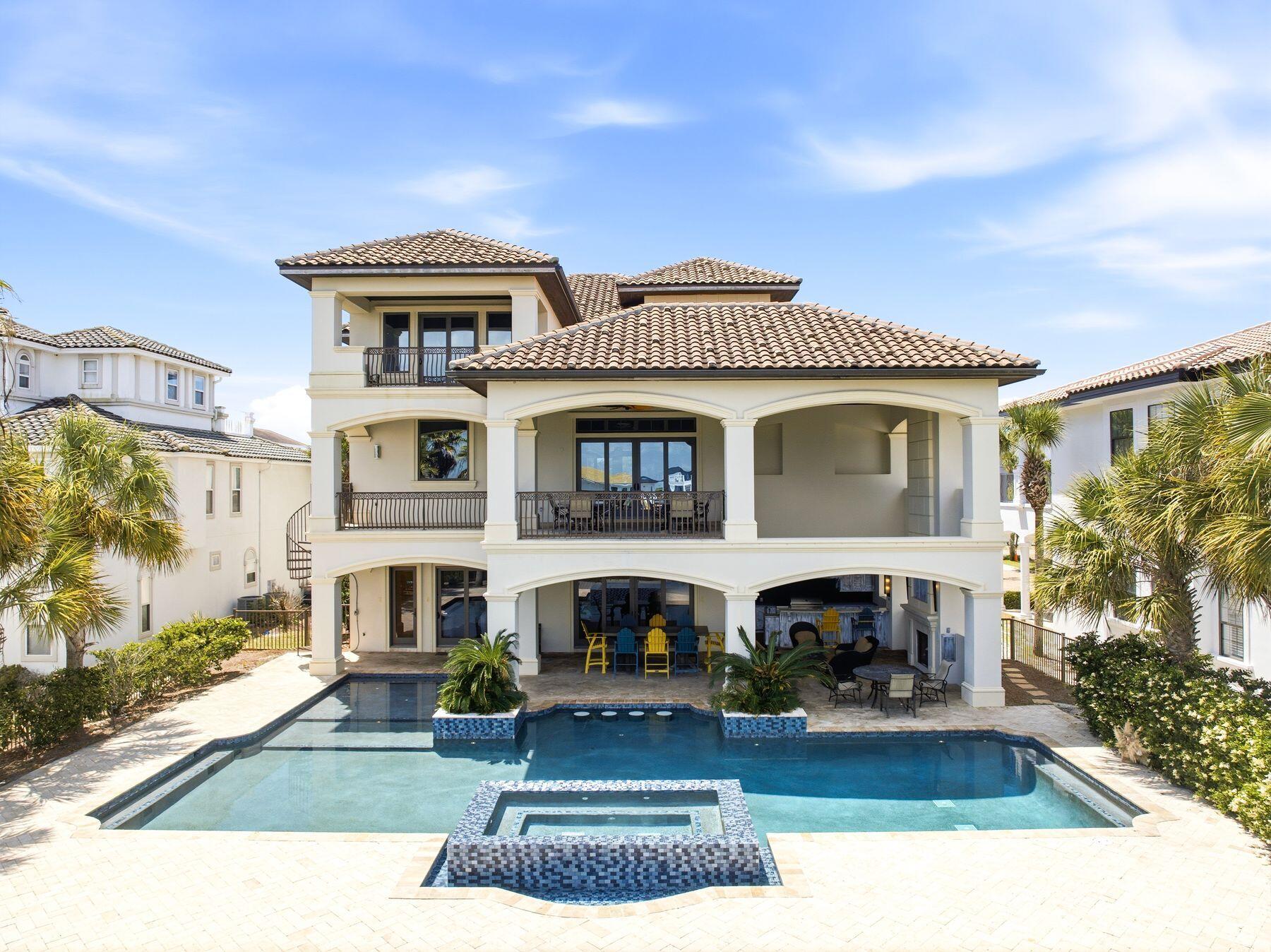 Welcome to an exceptional beachside retreat in the heart of Destin, where coastal luxury meets effortless income potential. Perfectly positioned with 61 feet of lake frontage and sweeping Gulf views, this remarkable residence is just steps from the sugar-white sands of the Gulf of Mexico and a short stroll to a sprawling beach access. The first level is designed for recreation and seamless indoor-outdoor living, featuring a spacious game room complete with a pool table, arcade games, and a convenient kitchenette with full-size refrigerator and ice maker. Multiple guest suites and bunk accommodations offer flexibility for large groups, while direct access leads to a true backyard oasis. The outdoor space lives like a private resort, highlighted by a beautifully designed pool with Baja shelf and spa, expansive sundeck, and tranquil lake views. A covered outdoor living area with a full kitchen, grill, beverage cooler, fireplace, and mounted TV creates the perfect setting for entertaining or unwinding after a day at the beach. A thoughtful feature includes an elevator servicing all three levels. The second level serves as the heart of the home, where an open-concept layout seamlessly connects the kitchen, dining, and living areas. A chef's kitchen anchored by an oversized island and premium appliances flows into a grand dining space accented with vaulted Pecky cypress ceilings and designer lighting, ideal for hosting large gatherings. The living room is filled with natural light and opens to a spacious balcony overlooking the pool and lake with direct access to the pool deck, adding convenience and extending the living space outdoors. Additional guest suites on this level provide comfort and privacy, with select rooms offering private balcony access. The third level offers a more private retreat with an additional living area and multiple well-appointed king suites, each with en suite baths. Select bedrooms feature soaking tubs and private balconies capturing glimpses of the Gulf, while additional bunk accommodations ensure ample space for guests. At the top, a rooftop viewing deck provides a breathtaking vantage point, where sunsets over the Gulf create an unforgettable daily experience. Offered fully furnished and turnkey, this expansive residence comfortably accommodates up to 28 guests and is ideally suited as both a legacy second home and a high-performing short-term rental. This is a rare opportunity to own a property that truly captures the essence of Destin living, blending scale, luxury, and an unbeatable location into one extraordinary offering.