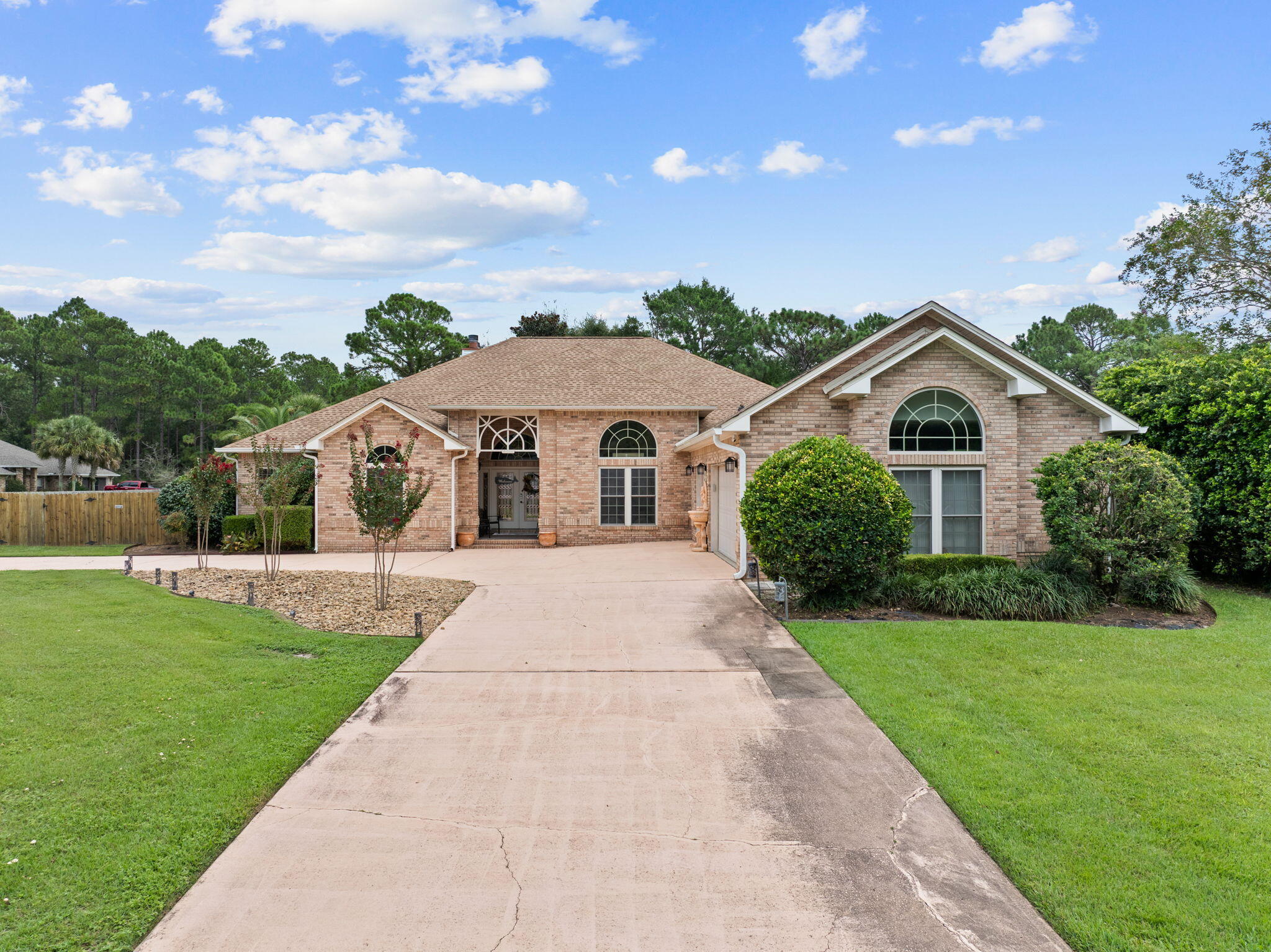 Welcome to this impressive custom home in the desirable Holley by the Sea community! Situated on a landscaped 0.55-acre corner lot, this brick residence offers approximately 3,288 square feet with great entertaining space. With over $200K in upgrades and metal storm shutters, the split floor plan features soaring 13-foot ceilings, crown molding, formal living and dining areas, and multiple fireplaces. French doors lead to a bright sunroom with a wet bar and access to the backyard patio. The kitchen offers upgraded appliances, ample cabinetry, granite countertops, and a large pantry. This 3-bedroom home features two primary-style suites: one with a fireplace, jetted tub, and walk-in shower, the other opening to a window-lined enclosed porch, heated and cooled for year-round use. A separate office adds flexible space for work or play. The oversized 3-car garage includes a climate-controlled section and half bath, and a matching brick outbuilding adds storage. Updates include newer HVAC systems, 2022 roof with transferable warranty, dog run, fans and lights, flooring, fence, garage doors, hybrid tankless water heater, and more. The home also has solar panels and is plumbed for gas, capped for future connection. Ownership includes recreation center membership: pools, clay tennis courts, fitness center, sound-side beach, fishing pier, and boat launch. The Club at Hidden Creek golf course is within the community. Come see all this Navarre home offers!