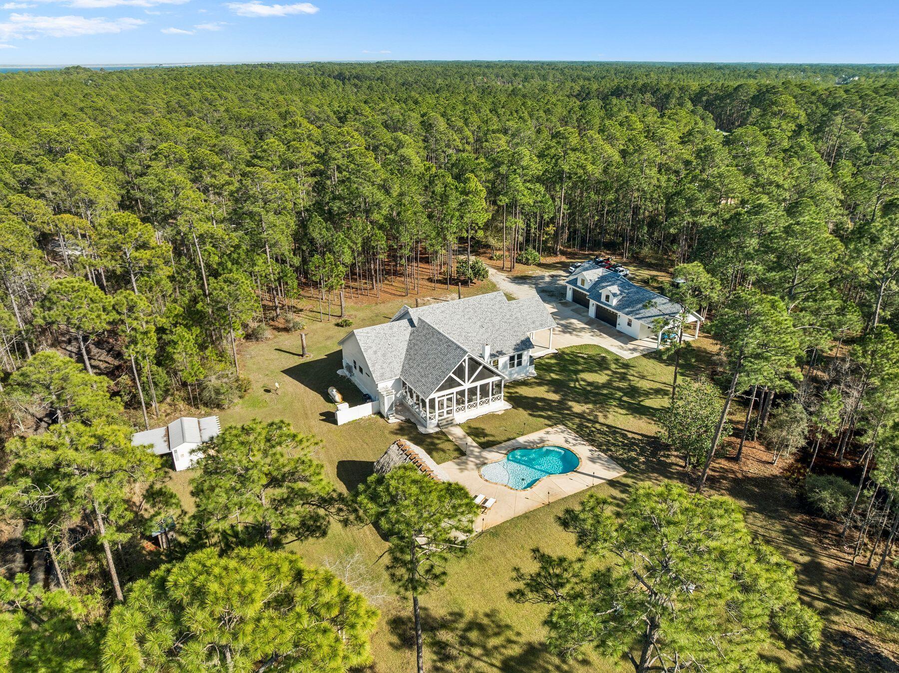 Set behind a gated entrance on ten private acres just north of Scenic Highway 30A, this thoughtfully upgraded coastal home offers a rare opportunity to enjoy expansive estate living just minutes from the beach. Surrounded by lush foliage and abundant wildlife, the property combines refined design, outdoor recreation, and future development potential in a setting that feels worlds away while remaining close to everything Santa Rosa Beach has to offer.

The four-bedroom, three-bathroom residence was designed with both everyday comfort and effortless entertaining in mind. Inside, an open concept floor plan centers on a spacious gourmet kitchen featuring a large standalone island, a wine and coffee bar, an ice maker, and a fully customized walk-in pantry. The living area creates a warm focal point with pine-inlay vaulted ceilings and a stacked-stone fireplace, accented by custom shelving. A dedicated office or flex space sits just off the main living area, offering versatility for work, hobbies, or additional guest accommodations.

Outdoor living is elevated through a vaulted screened-in patio that extends seamlessly from the back of the home. This inviting space features a wood-burning fireplace, lounge seating, and a dining area ideal for gatherings throughout the year. Beyond the patio, the property unfolds into a resort-style outdoor retreat complete with a large in-ground pool, tiki hut and bar, hot tub, and raised garden beds. Whether hosting friends, relaxing under the stars, or tending to the garden, the grounds provide a lifestyle centered on space and fresh air.

Recent upgrades have further enhanced the property, including full interior and exterior paint, updated lighting and fixtures, custom pantry and storage improvements, and refinished porches in durable Extira wood. The detached four-bay garage has been fully renovated with insulation, HVAC, workshop space, and upgraded lighting, creating a highly functional environment for hobbies, creative projects, or content production.

Additional features include a mudroom with extra storage and a dedicated dog washing station, a whole house generator, RV electric hookups, generous boat and trailer parking, a charming garden shed, and an additional outbuilding ideal for tools, equipment, or small livestock.

For those seeking long term flexibility, the property also presents exceptional future potential. Potential to divide the undeveloped rear five acres into two 2.5-acre homesites with existing easement
access allowing up to three additional residences, with an existing easement in place for convenient access.

Despite its peaceful setting, the estate remains close to local amenities. Cessna Landing boat launch is just minutes away for easy access to the bay, while nearby shopping, dining, and the renowned sugar white beaches of 30A are only a short drive away.

Private, spacious, and thoughtfully improved, this one-of-a-kind property offers a rare blend of acreage, luxury, and coastal convenience.

Furniture is negotiable.
