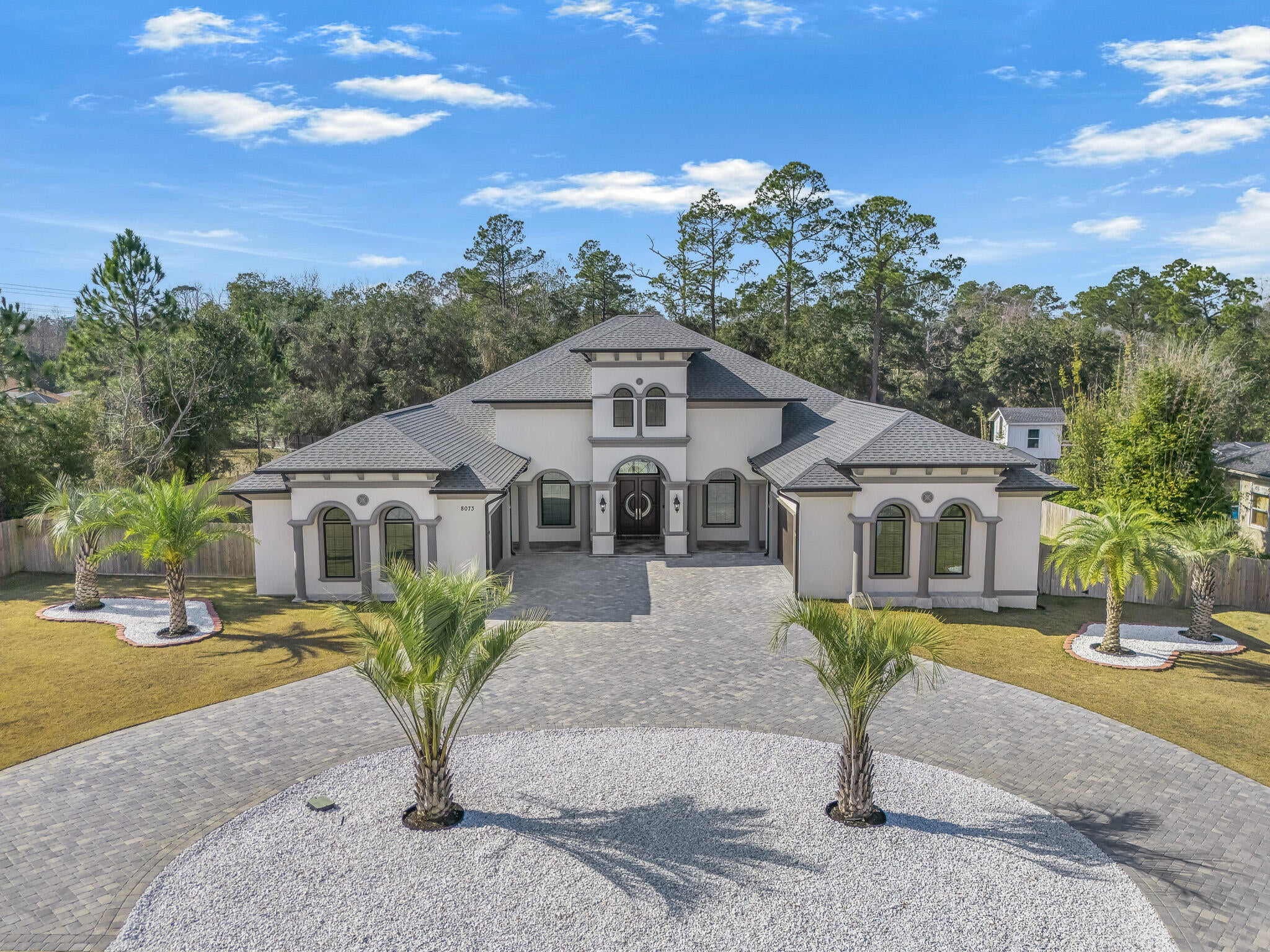 This exceptional, architecturally designed residence blends striking scale, thoughtful craftsmanship, & refined luxury into a home that feels impressive & inviting. Set on a 0.79-acre lot, the property immediately captivates w/its dramatic 24' front porch tower, soaring to a 32' roof peak—a bold statement that sets the tone for what lies beyond. Inside, 5,000 S/F of beautifully curated living space unfolds w/intentional openness and flow. Ceiling heights range from 10 feet to over 16'5'' in the Great Room, where custom ceiling designs, floating architectural walls, & a stunning 6-foot crystal chandelier create a sense of volume & elegance. A 45-foot open span & expansive 16-foot sliding glass doors invite natural light & seamlessly connect indoor living w/the outdoors. This exceptional, architecturally designed residence blends striking scale, thoughtful craftsmanship, & refined luxury into a home that feels impressive & inviting. HOME IS SOLD COMPLETELY FURNISHED!
Set on a 0.79-acre lot, the property immediately captivates w/its dramatic 24' front porch tower, soaring to a 32' roof peak a bold statement that sets the tone for what lies beyond. Inside, 5,000 S/F of beautifully curated living space unfolds w/intentional openness and flow. Ceiling heights range from 10 feet to over 16'5" in the Great Room, where custom ceiling designs, floating architectural walls, & a stunning 6-foot crystal chandelier create a sense of volume & elegance. A 45-foot open span & expansive 16-foot sliding glass doors invite natural light & seamlessly connect indoor living w/the outdoors. Every finish was selected for beauty and longevity. High-grade tile & luxury vinyl plank flooring extend throughout the home, front porch, & covered lanai, while 48-inch wide hallways & 8-foot solid doors enhance the home's grand, custom feel. The kitchen is the heart of the home anchored by a statement 9'5" x 5' Dolomite island, dual glass-front refrigerators, custom cabinetry, & an elegant in-wall wine cabinet, making it equally suited for everyday living & entertaining. Five spa-inspired bathrooms elevate daily routines w/floating vanities, frameless glass showers, smart bidets, touch-free fixtures, & illuminated mirrors, offering a retreat-like experience throughout the home. Outdoors, the property transforms into a private oasis featuring approximately 6,000 S/F of pavers, a circular drive, privacy fencing, & meticulously curated landscaping with mature palm trees, Zoysia grass, & white marble stone accents all supported by a dedicated irrigation system. With integrated security, mobile-controlled systems, and enduring construction throughout, this home is more than a residence, it's a thoughtfully crafted lifestyle, designed to be experienced, enjoyed, and admired for years to come.