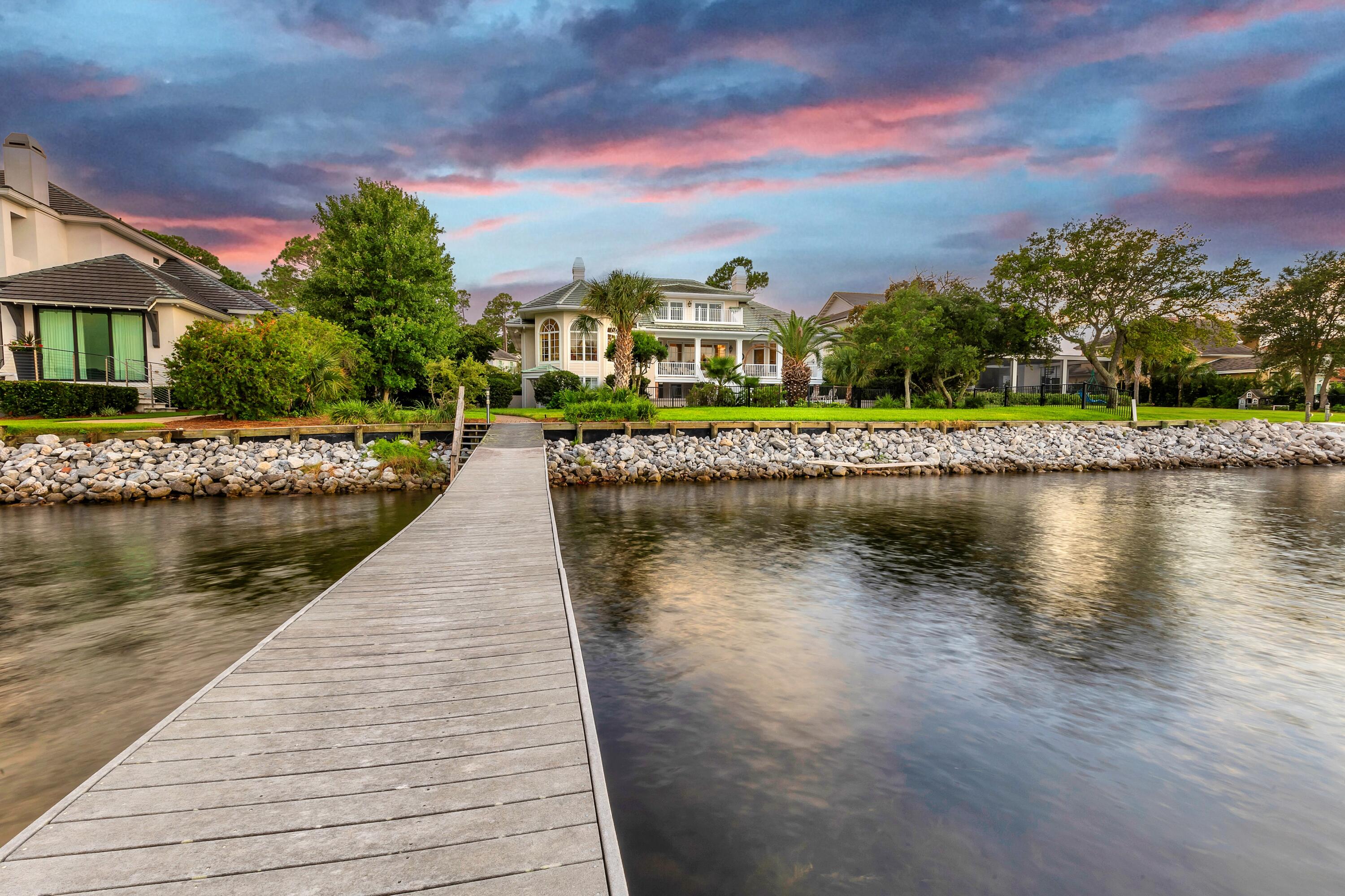 Timeless elegance on the bay behind the gates of prestigious Regatta Bay Golf and Yacht Club. This enchanting sanctuary sits surrounded by lush, mature landscaping, perched over 108' of water frontage with endless bay views. Remarkable in detail with deep porches and graceful design, it exudes a sense of grandeur while embracing impeccable craftsmanship and tranquil comfort. Reminiscent of Louisiana low-country homes, Prescott Architects' raised design highlights water vistas from every vantage point. A rare combination of warmth and space, it measures over 6000 square feet in heated space with over 1000 square feet of porches. Enter a commanding façade to a grand entry which reveals impeccable inlaid marble flooring joined by immaculate hardwoods. Substantial 10" layered crown molding, and 10' high ceilings complete the space. Arched, paned windows frame memorable sunsets and further enhance the remarkable design. Living, dining, and sunlit parlor flow seamlessly and serve as family's central gathering space and an entertainer's delight. The gourmet kitchen with prep island, serving bar, and breakfast area, boasts all white cabinetry, a separate wet-bar, Sub-Zero refrigerator, Viking gas range, and enjoys its own water views. An elevator conveniently services two of the homes floors and is flanked by a private powder room and additional storage. The main floor includes a bay front primary bedroom suite with its own cozy fireplace, dual vanity bath and a free-standing brass accented soaking tub with separate shower. The main floor is completed by a formal dining room and two additional bedrooms with a shared connected bath. Stroll upstairs for fun and games. The recreation room/library leads to its own private balcony through sliding full-wall glass doors. Spacious enough for a pool table and a crowd, it serves as the party spot but is secluded enough for a reading room. A full bath and heated and cooled storage area completes the space. First floor, a highly sought after and secluded guest suite with a kitchenette and private entry provides quiet and comfort for guests or extended family members. A full bath is attached to this suite, which also leads to the pool area. Downstairs is complete with laundry, two additional bedrooms and another full bath. The infinity pool and hot tub are classic in lines and timeless in detail. Recently redecked and measuring 30'X18', it plays a central role in the home's fun and allure. Mature landscaping leads to a seawall and to an extra long 160' dock with covered boat lift. The 3-car garage affords extensive space for vehicles and storage needs. This exceptional estate offers a lifestyle of grandeur in which every detail has been thoughtfully considered to create a haven of comfort and tranquility. Experience the enchantment where refined living meets natural beauty and indulge in an extraordinary retreat. Regatta Bay is a guard gated community boasting the Regatta Bay championship golf course, including the clubhouse and restaurant, tennis and pickle ball courts, and a community pool. A golf cart ride to the Legendary Marina and Yacht Club, Lulu's bayside restaurant, and the area's best beaches, shopping and dining, including Whole Foods and Destin Commons, it is Destin's most convenient location.