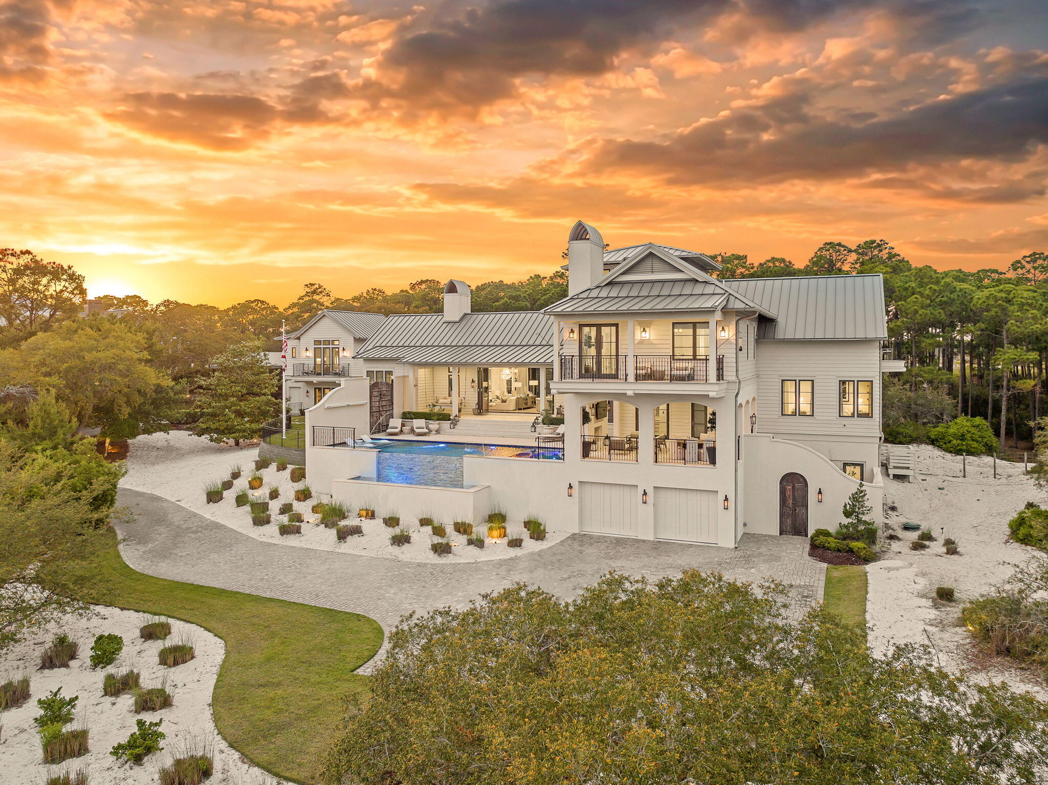 Tucked within the private, gated sanctuary of Four Mile Village, 285 Twisted Pine Trail presents an extraordinary opportunity to experience coastal living at its most serene and refined. Set on nearly three acres and bordered by the unspoiled beauty of Topsail Hill Preserve State Park, this remarkable estate offers a rare sense of privacy, where native wildlife and natural landscapes take center stage. From the moment you arrive, the canopy-lined drive evokes a sense of 'Old Florida,' a peaceful retreat far removed from the pace of everyday life.

One of the property's most exceptional features is its dual frontage, capturing both coastal dune lake and gulf views. Coastal dune lakes are among the rarest natural phenomena in the world, found in only a handful of locations globally... and this home enjoys sweeping vistas of Fuller Lake to the north and the gulf to the south.
Thoughtfully designed by Geoff Chick, the home blends timeless architecture with exceptional craftsmanship. Inside, curated details abound, from handcrafted lighting imported from Murano, Italy, to rich, rough-hewn cypress flooring that grounds the space in warmth and character. The expansive open-concept living and dining area is anchored by soaring vaulted ceilings, exposed beams, and a striking double-sided fireplace, all framed by walls of glass that capture panoramic water views.
The gourmet kitchen is both functional and elegant, featuring an oversized quartzite island, a full suite of Thermador appliances, and additional support spaces including a butler's kitchen, wet bar, and wine cellar, perfect for effortless entertaining. Retractable European doors seamlessly connect the indoors to multiple outdoor living areas, where covered porches, open-air decks, and an infinity-edge pool and spa create a resort-style setting overlooking the dunes and emerald waters beyond.
Each bedroom suite is designed as a private retreat, offering either lake or gulf views and uniquely crafted en-suite baths with custom tilework. The primary suite is a standout, complete with its own fireplace, private balcony, and a spa-inspired bath where both the soaking tub and shower overlook the gulf. Additional features include a third-level bunk room with a morning bar and a private elevator servicing all levels of the home.
A detached carriage house enhances the property with a first-level game room, wet bar, and golf cart garage, while the upper level provides a bright guest space with built-in bunks, a full bath, and sweeping views. Nearly 300 feet of lake frontage and a private dock further elevate the outdoor experience, offering direct access to one of the area's rare coastal dune lakes.
As part of Four Mile Village, residents enjoy access to over 230 acres of preserved coastal woodlands, a 40-acre dune lake, and more than 2,000 feet of private Gulf shoreline. Rich in both natural beauty and history, this one-of-a-kind property captures the essence of Northwest Florida's most treasured coastline, where luxury and untouched landscape exist in perfect harmony.