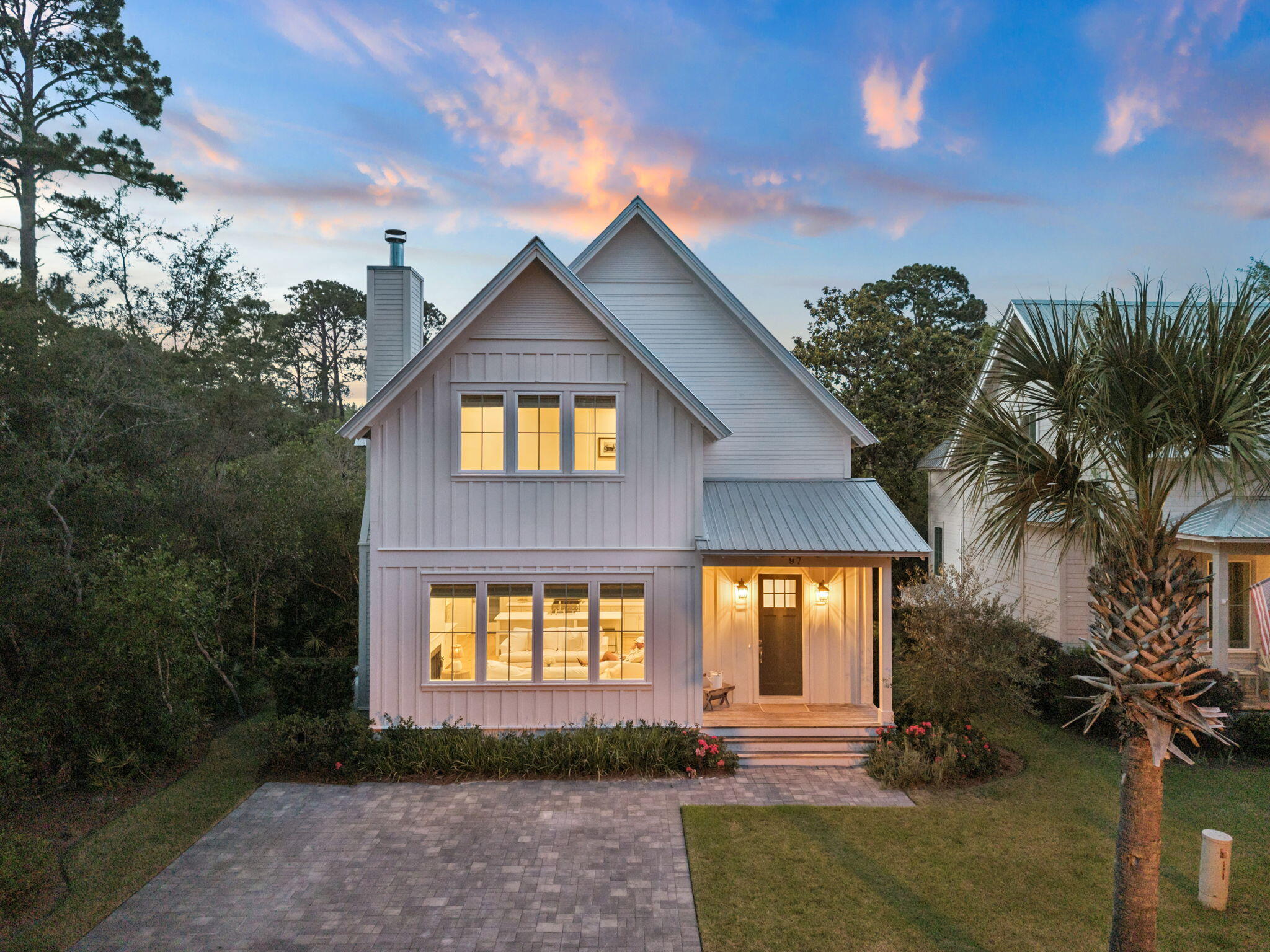 Tucked beneath a canopy of magnolias and longleaf pines just steps from Choctawhatchee Bay, 97 Greenbriar Lane is a coastal farmhouse that delivers the quiet, unhurried character of Old 30A without compromise on finish or function. Set within sought-after Grayton Bayou, this property offers rare proximity to the bay, a community pool and spa, and the natural beauty that makes this stretch of the Emerald Coast so enduringly special.

Crisp white board-and-batten siding, a standing-seam metal roof, and a paver motor court set a clean, timeless tone. Inside, wide-plank white oak floors and paneled walls flow through light-filled living spaces. A shiplap fireplace flanked by built-in shelving anchors the great room, while oversized windows frame the wooded backyard. The chef's kitchen features a large center island with farmhouse sink, quartz counters, a professional range with stainless hood, open shelving, and a secondary prep area with bar sink and beverage refrigerator. A separate dining room with chandelier rounds out the main floor.
A powder bath lacquered in deep charcoal with brass fixtures adds a bold, editorial moment downstairs.
The primary suite offers a spa-inspired bath with a freestanding soaking tub and glass-enclosed subway tile shower. Additional bedrooms with vaulted ceilings offer comfortable accommodations for residents and guests alike. A bonus room with cathedral ceiling provides flexible space for a media room, additional sleeping, or a lounge. A large rear deck overlooks the lush native landscape, and the community's bayfront green space with sweeping bay views is just a short walk away. Residents also enjoy a resort-style pool and spa, all minutes from Grayton Beach State Park, Western Lake, and Historic Grayton Beach.