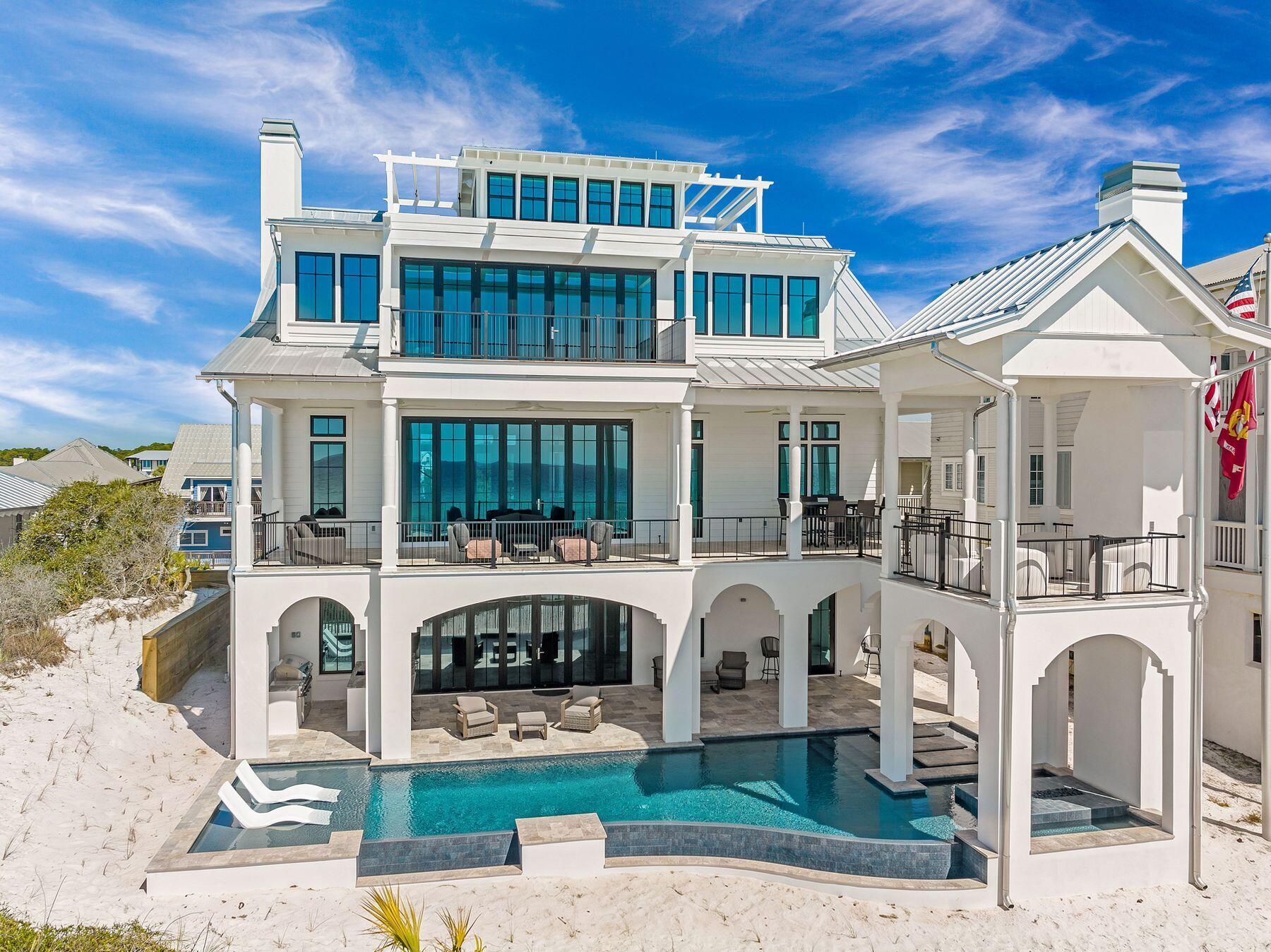 Most homes along this stretch of Grayton Beach play it expected. Whitewashed shiplap, soft coastal palette, the familiar vocabulary of a beach house doing its best impression of the one next door. Sixty-one Auburn does something different. The design intention here was coastal industrial, and builder Chris Burch of Grand Bay Construction and architect Chris Stoyles of Archiscapes committed to it completely. Exposed steel beams run the full height of the home, solid and horizontal on the ground floor, shifting to a triangular pattern on the second for a detail that is structural and sculptural at once. Nearly every wall surface is mitered nickel-gap paneling, and ceiling is tongue-and-groove. The lot itself is an asset before the front door opens. Auburn Drive carries some of Grayton's oldest and most beloved cottages, many raised on pilings with views earned over decades. This new construction, completed in 2026, occupies one of the street's highest natural positions and makes full use of it. The Gulf is visible from the pool deck, the kitchen, the primary balcony, and the watchtower. The state park fills the view to the north. The site works in every direction. The ground floor establishes the register. A marble fireplace anchors the main interior space while an oversized wet bar island in leathered quartzite handles the social load. Flanking Sub-Zero units, one a dedicated wine chiller and one a combination refrigerator with pebble ice and freezer, make the bar a serious operation. Seven-panel nano doors retract to open the entire south wall onto a gulf-front pool with a floating fire pit and sunning shelves. The summer kitchen carries the leathered quartzite through and adds a 52-inch DCS grill with side burner. A first-floor bedroom suite with a multi-head shower, soaking tub, dual vanities and a Moen smart toilet functions as a fully self-contained guest level. A flex room currently configured as a gym converts easily to office, bunk room or whatever else the moment calls for. The main living floor is where the coastal industrial intention reads most clearly. Triangular steel beams run the ceiling of a kitchen outfitted for real cooking: 48-inch Thermador dual-oven range, Bosch dishwashers, quartzite waterfall counters, a prep sink alongside the main, under-cabinet lighting, cabinetry with crown molding and uplighting, ceilings approaching 12 feet. Custom graphite pendants with bronze interiors provide the lighting anchor. A steel and glass door leads to the butler's pantry with GE Cafe convection microwave and oven, enough counter space to run a second line, and storage that actually gets used. Seven-panel nano doors open the south wall to a covered balcony with an outdoor fireplace and multiple configurations for alfresco dining. A north-facing balcony looks out over the state park. An elevator services all three primary floors. Above the garage, a fully self-contained one-bedroom, one-bath apartment with a full kitchen and Juliet balcony, handling extended family with equal ease. The third floor is quieter, more private, and built around the primary suite. An angular roofline pitches toward seven nano panels that open onto a private gulf balcony. A painted brick fireplace sits on the opposite wall. The bath is an exercise in material confidence: a stone countertop running cream into gray into oxidized orange, cement sink basins, a generously sized shower with rain head and multiple body sprayers, shell travertine tile on the walls, a freestanding tub enclosed within the glass shower surround, two casement windows framing the Gulf and a hidden linear drain that eliminates the need for a shower curb entirely. A pocket door leads to the primary closet with full built-ins, a dedicated shoe wall with cubbies, and HVAC service. Two additional guest suites occupy the third floor, both with direct gulf views and full en suites. One features a teak-panel tile shower with rain head and body sprayers. The other offers a slate herringbone shower floor. HVAC runs into every closet on the floor. The watchtower at the top operates on its own HVAC system. A pergola-covered corridor opens to the east. A porch swing faces west into the Gulf. There is a ceiling fan and double-hung windows and nothing else required. It is the kind of space that becomes a habit. Throughout the home: hidden-fastener clip decking with mitered flush-mount edges and water hookups at every balcony level, a view rail stair system with white oak treads and cable-and-steel handrails rising through all four floors, whole-home smart system, and whole-home surround sound. Five bedrooms, six full baths, and one powder bath. Two-car garage with epoxied floor and tiled stairs.