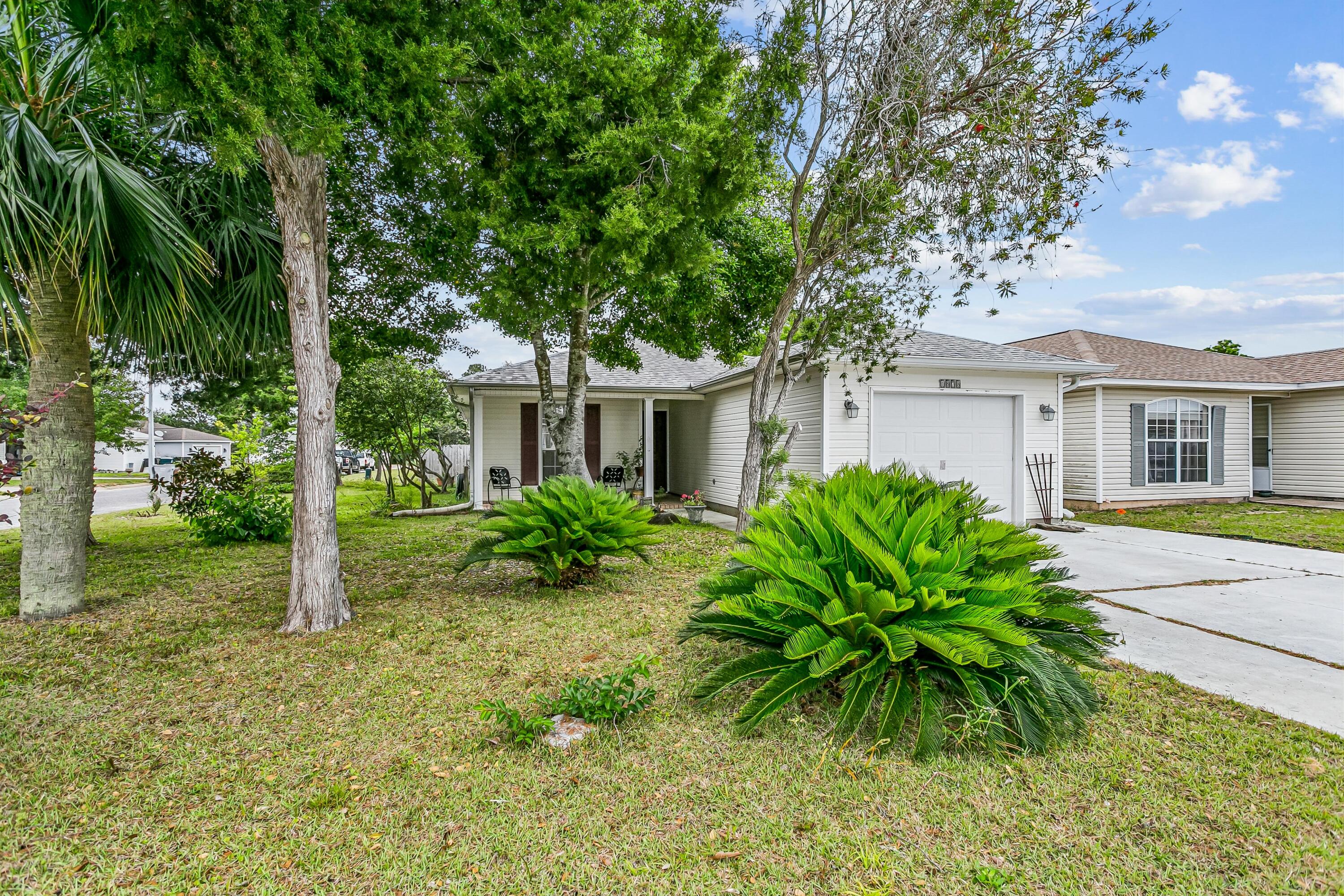 Perched on a corner lot shaded by mature trees, this adorable patio home in The Vineyard sits in one of Navarre's most convenient pockets: close to shopping, golf course, Gorgeous Navarre Beach, Hurlburt Field, and Eglin AFB. The split floor plan makes smart use of the space -- primary suite on one end, secondary bedrooms on the other, and not a square inch of carpet in sight. The living and dining areas are open to the kitchen, keeping the layout connected and social. The primary bedroom has an ensuite bath and a large closet, and the secondary bedrooms tuck neatly on the other side of the home.  The back Florida room is a real bonus -- lots of natural light and a relaxed space that works as a sunroom, hobby room, or just a good place to sit. The backyard is fenced with an open deck, giving you privacy and outdoor space without a lot of upkeep. The 1-car garage and vinyl siding exterior keep maintenance manageable.  Termite maintenance contract in place  ** HVAC permit 2018 ** Hurricane shutters ** Ready for a buyer who sees the value in a well-located property with room to make it their own. Priced right. Located well. Full of potential.