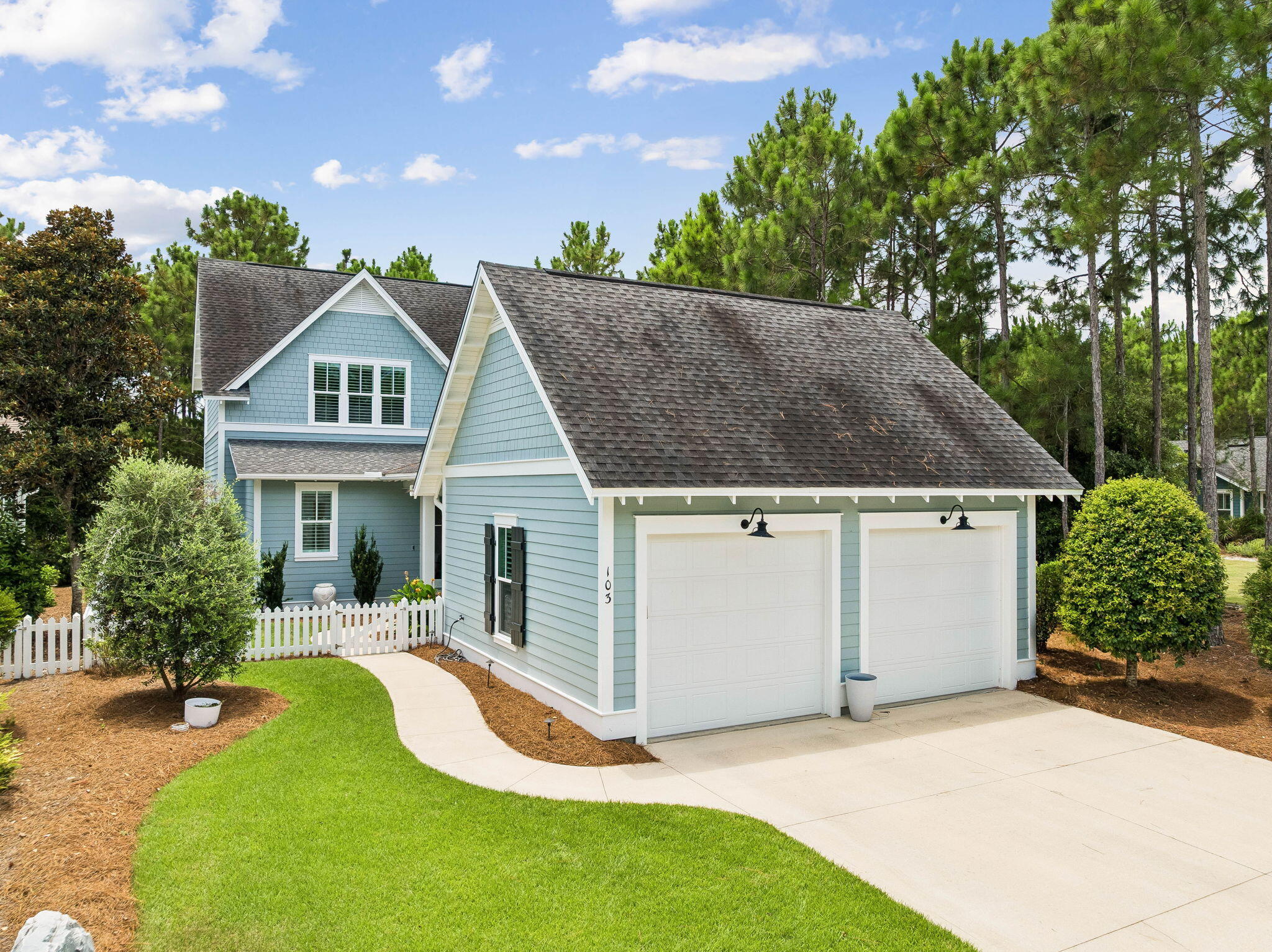 Tucked beneath the pines on a picket-fenced homesite in Watersound Origins, 103 Jack Knife Drive offers easygoing Florida living with timeless charm. This 3-bedroom, 2.5-bath home delivers classic curb appeal along with a detached two-car garage with gooseneck lighting, while inside you'll find a bright, thoughtfully finished interior. Wide-plank hardwood floors, shiplap accent walls, wainscoting, crown molding, and plantation shutters run throughout the main level, where the open living room flows to a dining area anchored by a beaded chandelier and a crisp white kitchen with quartz counters, subway tile, gas range, stainless appliances, oversized island seating, and a lighted glass-front bar/butler's nook. The main-level primary suite features a shiplap feature wall and a spa-style bath with double quartz vanity, soaking tub, and separate tiled shower. Upstairs offers two additional bedrooms plus generous walk-in closets and walk-in attic storage. Outdoor living shines: a screened porch with hanging bed swing and shiplap ceiling opens to an expansive paver patio with fire pit and café lighting, all wrapped by a white picket fence with green space beyond. Residents of Watersound Origins enjoy the Village Commons resort-style pool, fitness center, events lawn, miles of nature trails, Origins golf, and Lake Powell access, all just minutes from 30A's beaches, dining, and the Watersound Town Center.