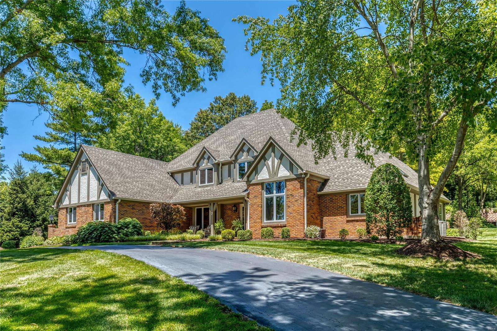 An impressive brick, stucco & cedar elevation highlights the remarkable curb appeal of this spectacular 1.5-sty Tudor. Open floor plan features well-proportioned rooms with soaring ceilings, detailed trim work, plantation shutters & oak hardwoods that extend throughout the main living area. Impressive 2-sty foyer with dramatic flared staircase leads to well-appointed study with 11’ ceiling & French doors, formal dining room & vaulted great room with wet bar & floor-to-ceiling stacked stone fireplace. Designer kitchen with 42” white cabinetry, Viking appliances, 12’ center island & convenient planning center adjoins light-filled breakfast room. Main floor primary bedroom suite with wide bay window & luxury bath with jetted tub offers an appealing retreat. T-staircase accesses 3 additional ensuite bedrooms. Lower Level includes recreation room with wet bar, game room, office, workout room & full bath. Situated on a .85-ac lot with aggregate patio & pool surrounded by landscaped gardens.