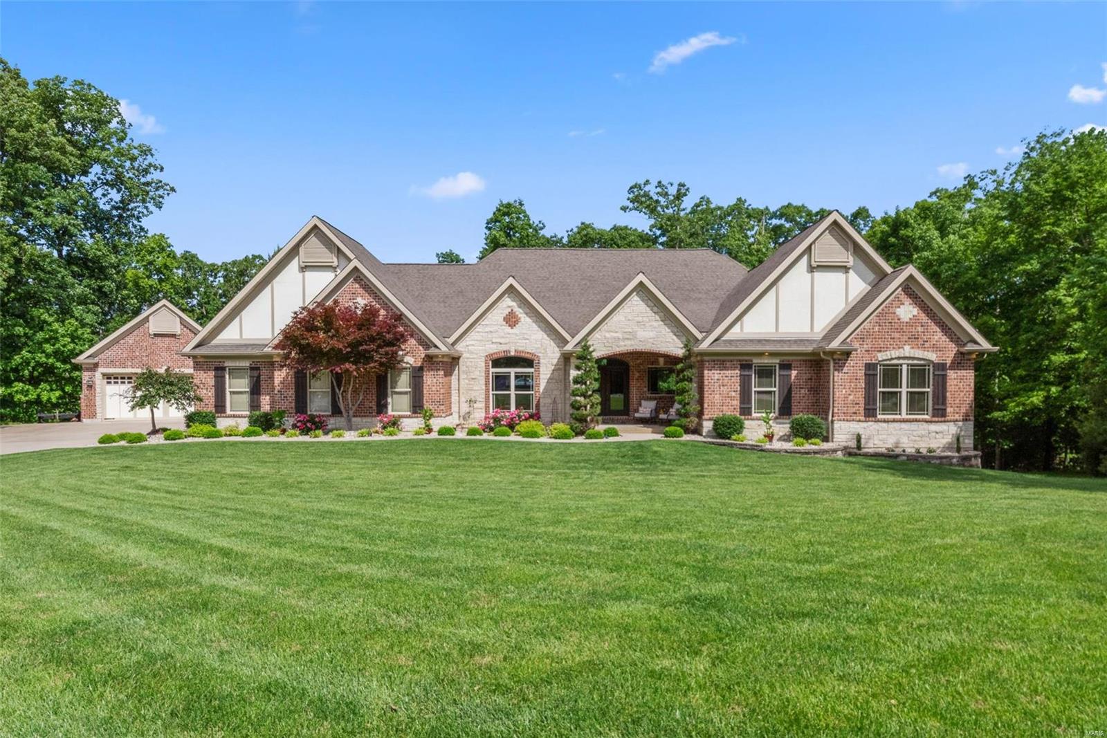 This sprawling ranch w/4+ acres of wooded land in an exclusive neighborhood offers more than 6,200 sq ft of livable luxury. Soaring vaulted ceilings & rich oak hardwood floors in the open main living area, including the great room anchored by a floor-to-ceiling stone fireplace flanked by windows w/stunning wood views. Chef's kitchen has endless custom cherry cabinets, granite counters, huge breakfast bar, & SS appliances, including double wall ovens & built-in fridge. Curl up by the fire in the hearth room. Primary suite w/sculpted ceiling, walk-in closet, & ensuite bath w/jetted tub & oversized seated multi-head shower. Private accessible guest suite w/mini-kitchen, & bath w/step-in/roll-in shower. Enormous finished walk-out LL w/9' pour includes a rec room, media room w/gas fireplace & wet bar, gym, office, playroom, 2 bedrooms, & full bath w/shower. Attached oversized 2-car & detached 2-car garage. Francis Howell Schools. Short drive to I-64/364. What an opportunity! See it today!