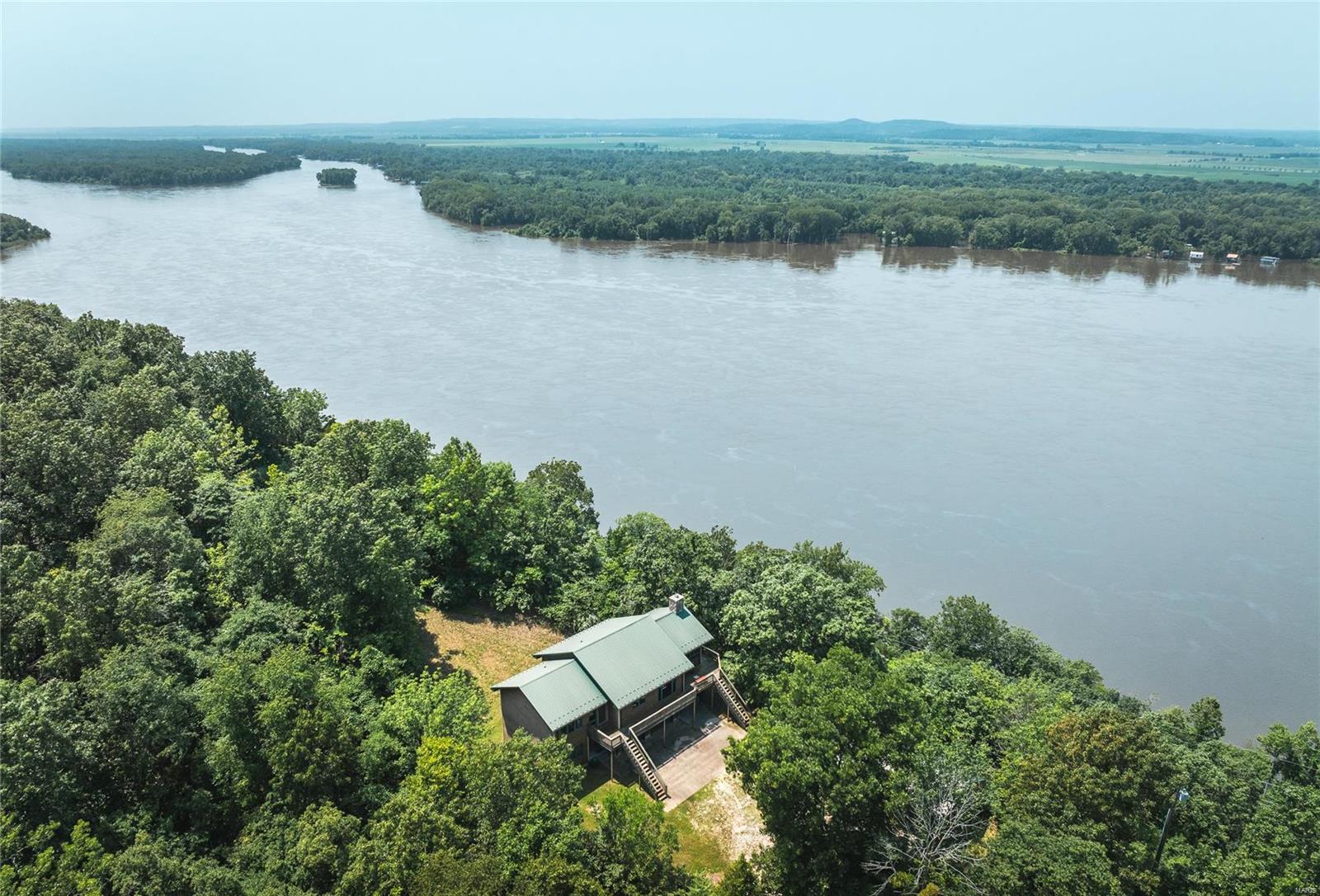 Perched majestically on the bluffs overlooking the Mississippi River, this exceptional 2-story cabin offers a breathtaking sanctuary spread across 154 acres of wilderness. Upon entering, the spacious living area welcomes you with floor-to-ceiling windows that frame panoramic views of the river below. Hardwood floors & knotty pine walls create a warm, inviting atmosphere, complemented by a magnificent wood-burning fireplace that serves as the heart of the home. For outdoor enthusiasts, the expansive property is a paradise. Hunters will appreciate the abundance of wildlife roaming through the mixed timber & open food plots. Nature lovers will revel in the sight of eagles soaring above the river, while fishermen can explore the 2 stocked ponds. Additionally, you will find 3 garages (2 detached, 1 attached) provide ample storage for vehicles, boats, & outdoor gear. Just a short 5-minute drive away lies the boat ramp, offering convenient access to the Mississippi River.