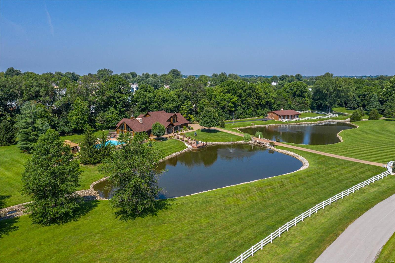 Exceptional gated rustic estate on parklike 7-acre grounds. This stone & cedar 1.5 Sty features soaring ceilings, oak hardwoods & expansive windows that offer continuous vista views throughout the home. Impressive entry foyer leads to private study, formal dining room with wine bar, spectacular great room with cathedral ceiling & stone see-through fireplace and paneled sunroom with fireplace. Designer kitchen with knotty alder cabinetry, granite countertops, KitchenAid appliances & horseshoe center island adjoins vaulted hearth room highlighted by floor-to-ceiling fireplace & adjacent gathering bar. Primary bedroom suite with beautifully appointed bath with shower spa provides an appealing retreat. The 2nd floor extends the living quarters w/3 additional bedrooms & hall full bath. Walk-out Lower Level includes recreation room, game room, family room, office, workout room & full bath. Premium cul-de-sac lot with deck, covered patio, pool & gazebo plus 3-stall barn & 2 stocked ponds. Additional Rooms: Mud Room, Sun Room