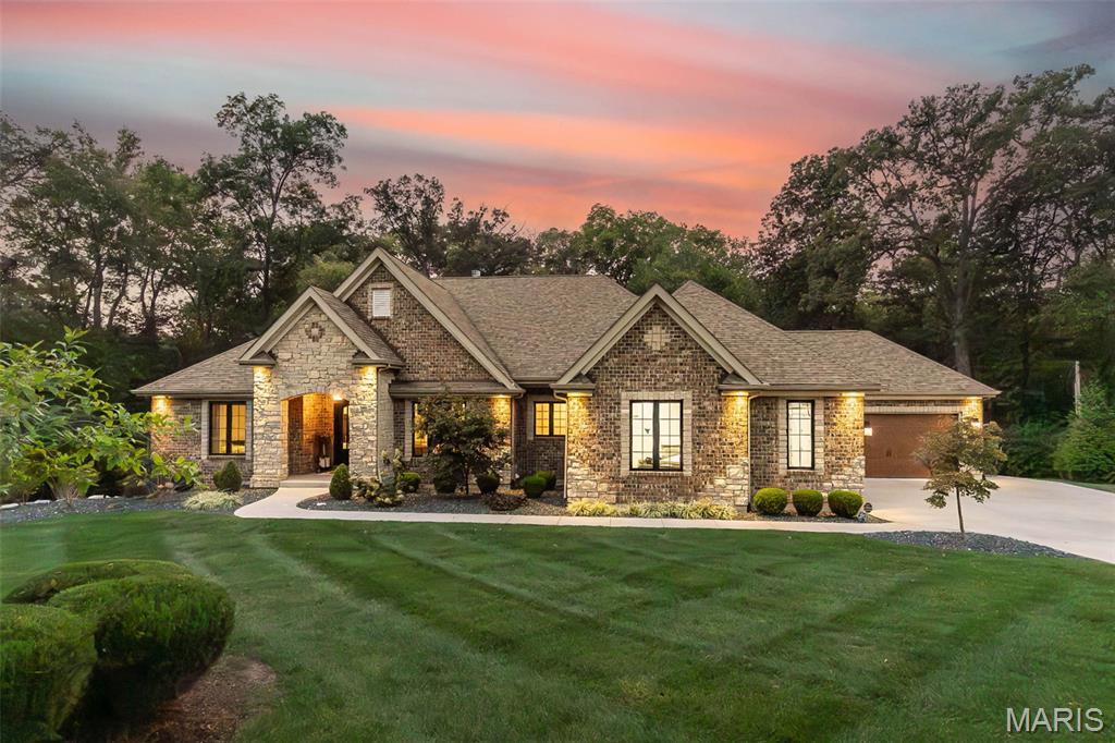You don’t want to miss this showstopper! A stunning sprawling ranch on a private 1.67 acre treelined lot in Lake St. Louis that includes a lot on Fernwood Ter—giving you full access to coveted Lake St. Louis amenities and lifestyle!
This home offers over 5,000 sq ft of luxury living space, featuring 4 bedrooms and 3.5 bathrooms. Car enthusiasts will fall in love with the enormous climate-controlled 4-car auto court featuring polymer flooring, 8-ft insulated doors, and a service door to a patio and sidewalk. 
Inside, you’re greeted by 12-ft ceilings in the great room, 9-ft ceilings throughout, 8ft doors, and French doors opening to a private lounge with a double-sided fireplace. The curb appeal is unmatched with an all-brick & stone exterior, Ebony casement windows, arched Iron&glass dbl entry door, irrigation system, soffit lighting, landscaping, and a timeless hip roof.
The chef’s dream kitchen showcases a gas stove with double ovens, range hood, pot filler, custom tile backsplash, walk-in pantry, and built-ins. A split-bedroom design ensures privacy, while the primary suite stuns with wood floors, spa-like bath with dual vanities + a prep station, oversized walk-in shower, and a custom closet with built-in laundry!
The recently finished lower level (2,400 sq ft) is perfect for entertaining—complete with billiards, media, family, exercise area with custom lighting, 4th bedroom, 3 full bath, and more. Outside, relax on the covered deck with recessed lighting and a fan, overlooking your wooded retreat.
This home truly has it all—style, space, and the exclusive Lake St. Louis lifestyle you’ve been waiting for! Full features list will be attached and available upon request. Truly a gorgeous home, you won't want to miss.