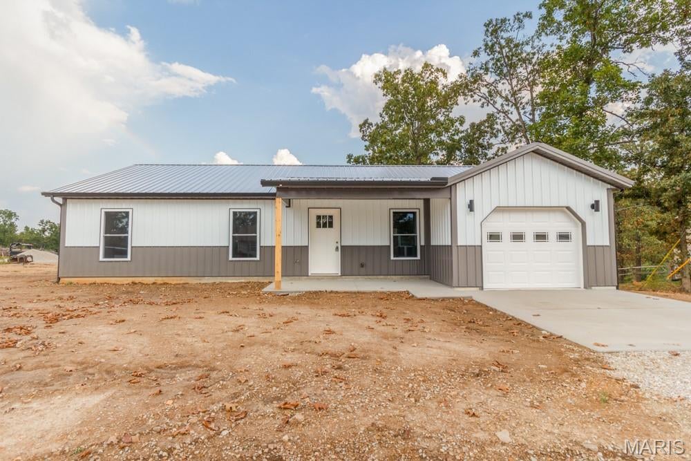 Brand-new construction home with modern style, a well-thought-out design, and energy-efficient features, all located within a 10–15 minute drive of the main gate of Fort Leonard Wood. This 3-bedroom home sits on a 0.29-acre lot with a one-car garage. The exterior features vertically ribbed metal siding and a matching metal roof, providing a durable and low-maintenance exterior.
The home features a very practical floor plan, with attention to detail throughout the interior finishes that include  two-panel shaker-style interior doors, wide-profile baseboard trim, and white woodwork throughout with cased openings around the windows.  Other features include luxury vinyl plank flooring, recessed lighting, white cabinetry, and matte-black fixtures. The kitchen features high-quality cabinetry with soft-close doors and drawers, beautiful butcher block countertops, a pantry, and a suite of LG stainless-steel appliances, including the refrigerator, electric range with ceramic cooktop, microwave hood, and dishwasher. The living room is quite spacious and is open to the kitchen and dining area, creating a comfortable and functional layout. The dining room is generously sized and conveniently located just off the kitchen.
The home also offers several practical storage and organization features, including a small mudroom nook just inside the garage entry.
The primary suite features recessed lighting, two closets—including a semi-walk-in closet with an organizer—and a private bathroom. The primary suite bath offers a stylish vanity, over-the-toilet cabinetry, and a large fiberglass shower. Two additional bedrooms provide comfortable living space, along with a second full bathroom featuring a single vanity, tub/shower combination, and medicine cabinet.
The home is equipped with an efficient heat pump for heating and cooling. The exterior walls are foam insulated, while the attic features blown cellulose insulation.
Outside features include a covered front porch and a nice-sized rear deck with steps leading to the backyard. The backyard provides a good amount of very usable outdoor space for relaxing, entertaining, or enjoying the outdoors.
This home combines the benefits of brand-new construction and modern finishes with durable exterior materials, energy-efficient features, and a convenient location near Fort Leonard Wood. Seller is also offering up to $5,000 in seller concessions at an agreed-upon purchase price and other contract terms.